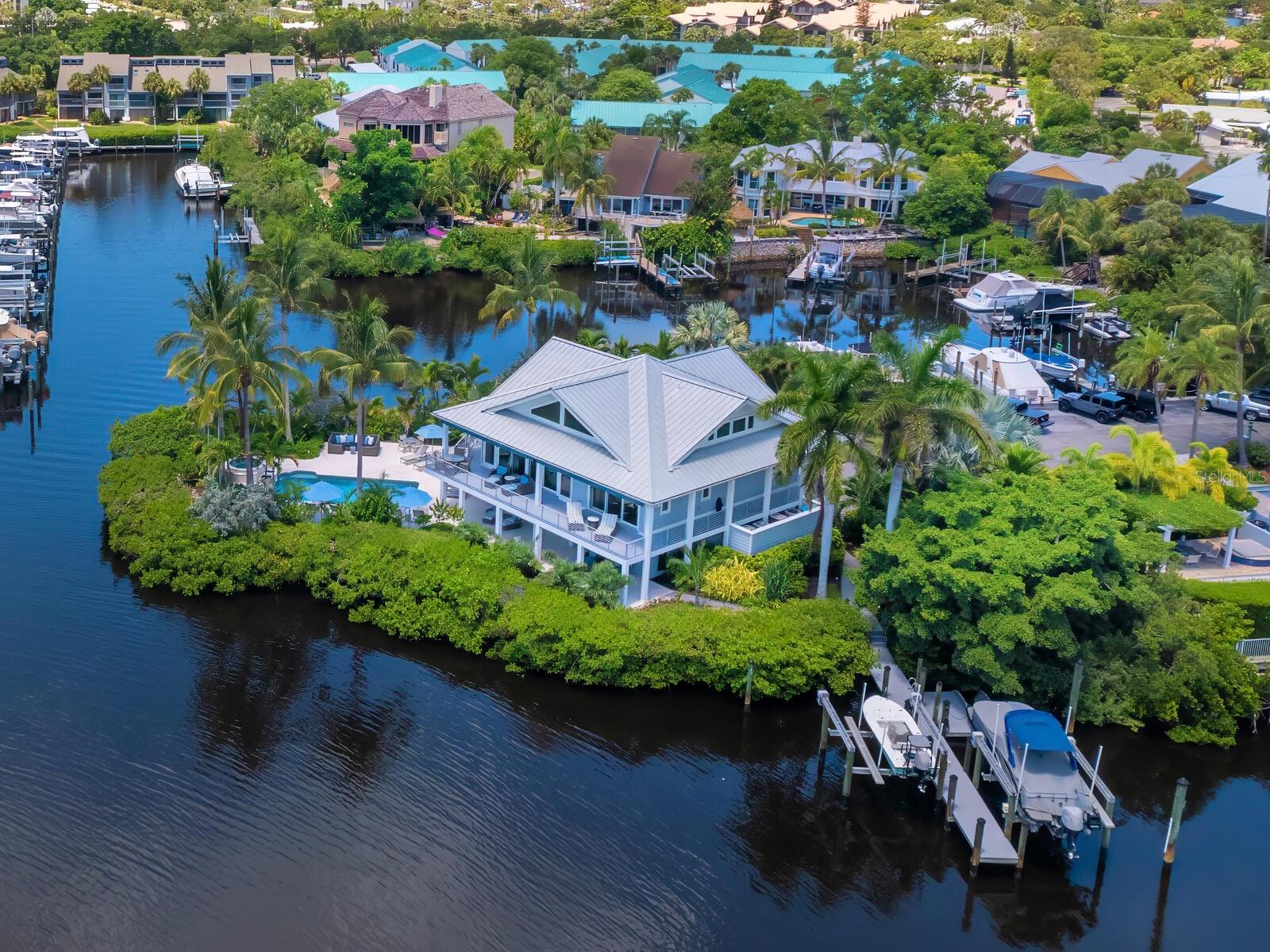 When home feels like a permanent vacation, every day becomes a tropical escape where time slows down, the water is always nearby, and every day begins and ends with a coastal breeze. That’s the essence of 5727 Riegels Point—a casually luxurious, resort-style property where the lifestyle is as effortless as it is extraordinary. Nestled within the gated enclave of Riegels Landing on Siesta Key, an exclusive community with fewer than 30 estate homes, this unique property offers a lifestyle where outdoor living is as exceptional as the interior. Step into your own island sanctuary, surrounded by 357 feet of deep-water shoreline on a private basin with direct Intracoastal access. It’s a true boater’s paradise, complete with two 10,000-lb boat lifts, a floating kayak launch, water and electricity at the dock, and lit pilings perfect for nighttime fishing. The water is deep enough for a large-scale yacht to sit comfortably at your dock. Expansive Shellstone patios wrap around the home, offering countless spaces to relax, dine, and entertain. The saltwater pool and raised spa, framed by fire and water features anchor this private resort experience. Remote smart controls make it easy to unwind in the pool and spa after a sunset cruise. The front entry showcases coastal curb appeal with double frosted glass doors, leading into an interior that blends casual sophistication with the ease of turnkey living. The great room is open and airy, with engineered wood floors and abundant natural light. Large sliders provide seamless access to the outdoor amenities, creating a perfect space for both entertaining and casual relaxation. The chef’s kitchen is designed for both form and function, featuring Wolf cooking appliances, a Sub-Zero refrigerator, a Miele dishwasher, a galley sink, and custom cabinetry throughout. Hidden outlets at the cabinet base and multiple pantries, plus clever storage built into the island, keep everything organized with ease. The primary suite is a serene retreat with engineered hardwood floors, a access to a waterfront terrace with Trex decking that wraps around the entire home, and well-thought-out blind and electrical automation. The luxurious bath features lighted mirrors, dual sinks, a makeup vanity, a free-standing tub, a walk-in shower, and a Toto commode. The suite also includes a spacious walk-in closet with custom built-ins. Upstairs, two generous guest suites share a well-appointed full bathroom. Two loft areas provide the perfect space for reading, working, or relaxing. The lower level offers a multifunctional space, featuring a living space, fitness room, sliders to access the outdoor space, and a wine room with plumbing for a cooler. Additional features include a spacious 2-car garage with custom built-ins, Control4 smart home technology for lighting, AV, security, and more, four HVAC zones for comfort, turnkey furnishings, a whole-house water softener system (salt and carbon filters), a whole house generator and an oversized laundry room with custom organization. At 5727 Riegels Point, enjoy island living with easy access to Sarasota and Siesta Key Village’s dining, shopping, and entertainment. Siesta Key Beach, recently named the No. 1 beach in America by Tripadvisor, is just moments away, offering powdery sand, clear waters, and stunning sunsets. From dockside mornings to poolside evenings, this is coastal living at its best—a full-time escape where your dream lifestyle unfolds.