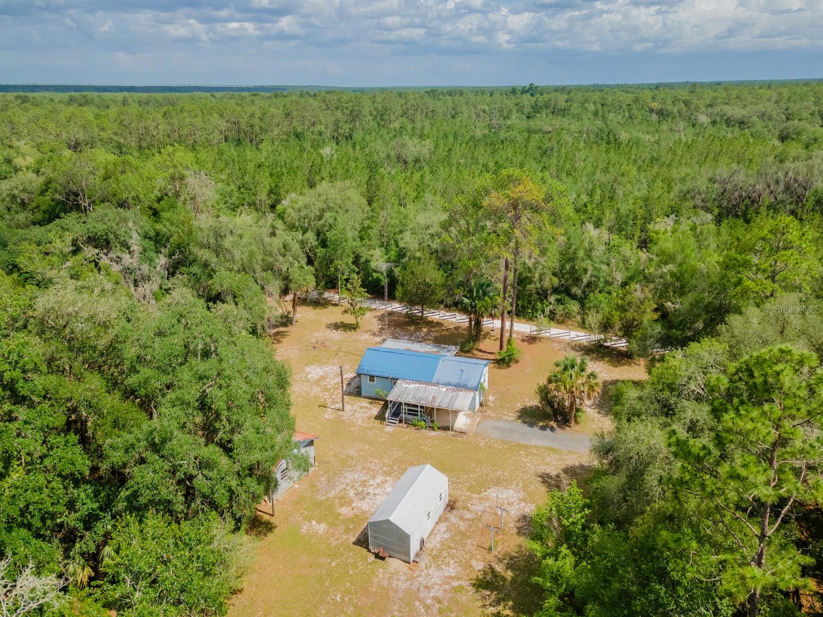 Country Living on 1.63 Private Acres

15265 Country Club Blvd, Fort McCoy, FL 32134
1 Bedroom | 2 Bathroom | 866 Sq Ft | 1.63 Acres | Pole Barn | Workshop

Looking for privacy, room to spread out, and a property with endless possibilities? Welcome to this charming country retreat situated on 1.63 beautifully cleared acres shaded by mature trees and surrounded by the peaceful natural beauty that makes Fort McCoy such a desirable destination.

Originally built in 1967, this well-maintained home offers 866 square feet of living space with an open, inviting floor plan and metal roof(2000). As you approach the home, you'll be welcomed by a spacious 10' x 28' screened porch, the perfect place to enjoy your morning coffee, relax with a good book, or unwind after a day outdoors.

Inside, the living room is surprisingly spacious and filled with natural light from numerous windows(updated in 2006). The flexible layout offers enough room to potentially create an additional bedroom if desired. The kitchen features abundant wood cabinetry, generous countertop space, and includes all appliances, including range, refrigerator, and microwave.

Just beyond the kitchen is a versatile den or office area with built in cabinets and a bathroom with tub/shower and single vanity. Also leads to the main bathroom and primary bedroom suite. The bathroom includes a tiled shower, single-sink vanity, and convenient laundry area. The primary bedroom measures approximately 12' x 18.5', offering plenty of room for larger furniture and featuring a walk-in closet.

Step outside through the rear entrance to find a small wood deck overlooking the backyard and an attached single-vehicle carport. The property continues to impress with numerous outbuildings and improvements. A 20' x 24' metal pole barn includes large double doors, water service, 110/220-volt power, and a dedicated workshop area—ideal for hobbyists, mechanics, or equipment storage. A newer 12' x 24' metal storage building provides even more room for tools, recreational equipment, or seasonal items.

Also included is an older 1-bedroom, 1-bath travel trailer with water and electric already connected, offering potential guest accommodations, storage, or future project opportunities.

Conveniently located just 10 minutes from downtown Fort McCoy, you'll have easy access to grocery stores, restaurants, pharmacy, hardware store, gas stations, and medical services. Silver Springs and Ocala are a short drive away for expanded shopping, dining, and entertainment options, while Gainesville is approximately 50 minutes away.

Outdoor enthusiasts will love being minutes from the Ocklawaha River, Ocala National Forest, and some of Florida's most beautiful natural springs, including Salt Springs, Silver Glen Springs, and Juniper Springs. Fishing, hunting, kayaking, hiking, horseback riding, and off-road adventures are all within easy reach.

Whether you're looking for a full-time residence, weekend getaway, hobby property, or investment opportunity, this unique property offers privacy, versatility, and a fantastic North Central Florida location.

Ready for new owners—schedule your private showing today!