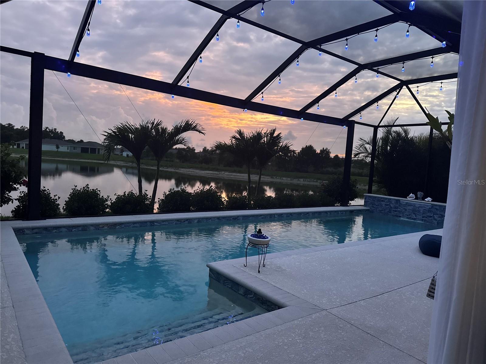 FULLY CUSTOMIZED HOME with WATER VIEW. Amazing CUSTOM-BUILT LAP POOL with TETHER overlooking the water and fountain. Home is surrounded by mature landscaping and professionally placed sod yard. Front entrance is covered and screened so you can leave your shoes at the front door. SPLIT FLOOR PLAN with TWO GUEST BEDROOMS to the immediate left upon entering the home. Guest bathroom is elegant with dual shower curtains from floor to ceiling, no-slip tub, modern fixtures and matching whole house GRANITE vanity. Continue through the extra wide foyer to the OPEN FLOOR PLAN with kitchen, dining and living room combo. Notice the CUSTOM PAINT, HIGH CEILINGS, CROWN MOLDING, PICTURE FRAME WINDOW CASING, DOUBLE PANE THERMAL WINDOWS, WALL SHELVING, FLOOR TO CEILING DRAPERY, large modern CEILING FAN and ELEGANT LIGHTING. Welcoming Chief Kitchen with matching whole house GRANITE COUNTER-TOPS, STAINLESS STEEL APPLANCES, SINGLE-BOWL XL KITCHEN SINK, GARBAGE DISPOSAL, LUXURY FAUCET, and lots of storage and countertop space for cooking and of course the amazing WALK IN PANTRY. Just before entering the primary suite, you will find the laundry room with its custom butcher block countertop and extra storage below and above The PRIMARY SUITE has plenty of room for your KING SIZE BED with DUAL WALK-IN CLOSEST, HIGH CEILINGS, CROWN MOLDING, CUSTOM SLAT WALL, LUXURY LIGHTING and wall to ceiling drapery. The PRIMARY BATH presents with a PROFESSIONALLY PAINTED MURAL, CUSTOM PAINT, DUAL SINKS with matching whole house GRANITE COUNTERTOPS, WALK-IN, SUNKIN SHOWER with sliding glass doors, private WATER CLOSET, CUSTOM WALK-IN CLOSET with all the bells and whistles! Welcome to your happy place by the pool as you walk through the soundproof DOUBLE PANE THERMAL extra-large SLIDING GLASS DOOR into the covered lounge area. The CUSTOM LAP POOL with WATERFALL is simply amazing and provides a TETHER for your swimming athlete. The pool cage is surrounded by classy lights, and multi-colored LED POOL LIGHTS light the water for the pleasure of all. Watch the wildlife around the lake, listen to the fountain or watch the sunset from your private space with mature ARCADIA PALM privacy hedge. WHOLE HOUSE RING SECURITY SYSTEM with MOTION SENSITIVE LIGHTING at the garage and by the pool. Irrigation system, custom gutters, hurricane shutters, large WIRE STORAGE RACKS in the garage for overhead premium storage and LEVEL 2 HARDWIRED EVSE for your ELECTRIC CAR. 
20 minutes to downtown St. Petersburg, 40 minutes to the airport in Clearwater, 30 minutes to the beach. A MUST SEE!!!