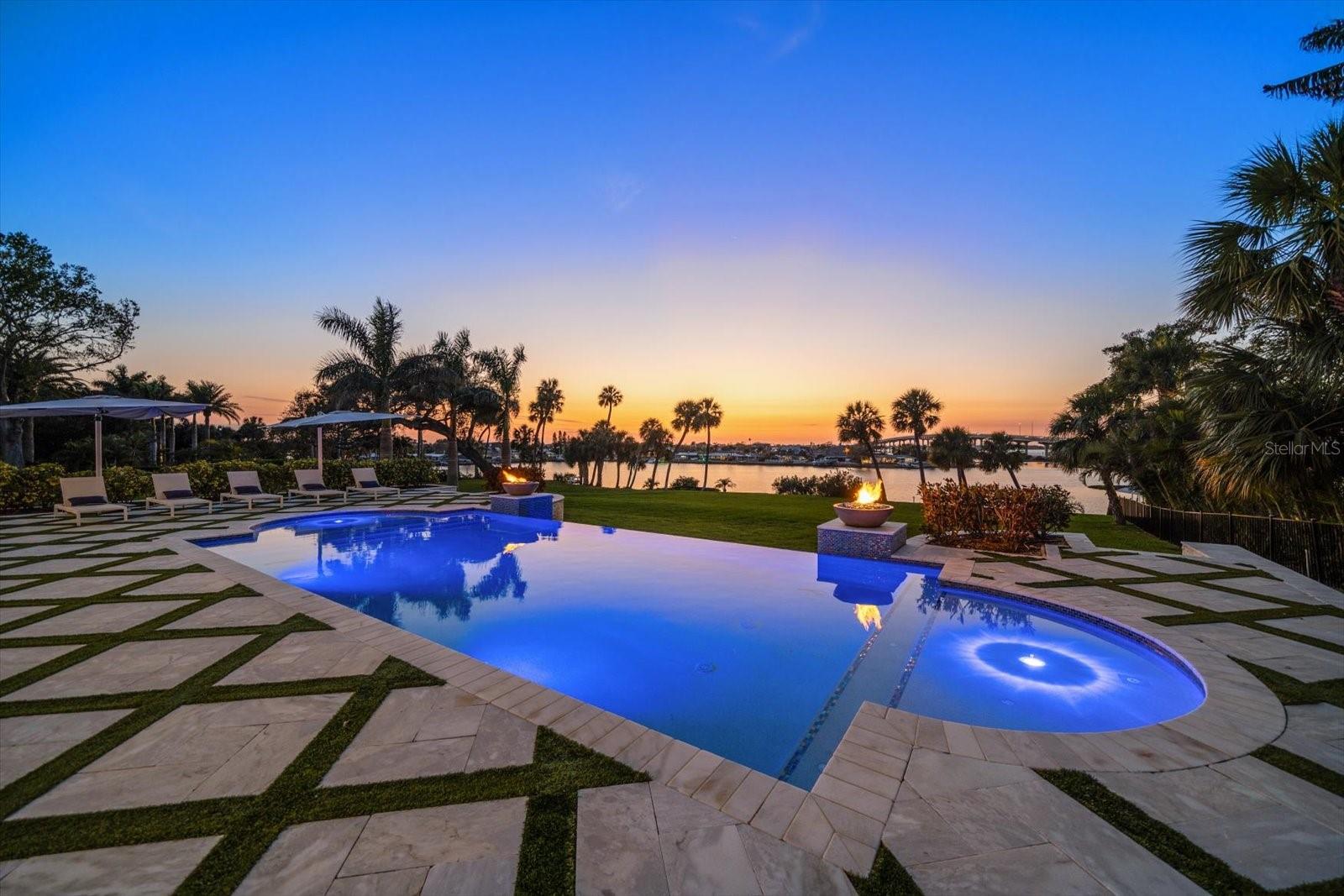 Experience modern luxury in this contemporary estate perched atop a bluff, standing 35+ feet high above base elevation on a sprawling 1+ acre lot with breathtaking views of the intracoastal waterway. Upon entering the grand foyer, you’re greeted by an impressive double staircase and soaring 20+ foot ceilings that seamlessly lead into an expansive living room framed by floor-to-ceiling windows. Elegant pearl marble flooring flows throughout the home, while the bedrooms showcase rich hardwood floors. Expansive glass doors and generous windows capture picture-perfect sunsets year-round. This residence boasts an array of upscale features including professional-grade appliances from Wolf, Sub Zero, and Bosch, two luxurious linear fireplaces, a recessed LED lighting system, and a private elevator. The massive chef's kitchen features onyx countertop, white cabinetry, pot filler, dual dishwasher, gas range and is a great place to entertain. The first floor primary suite offers stunning views, a linear fireplace and dual walk-in closets. The primary bath features a glass enclosed shower, dual floating vanity and soaking tub. The additional bedrooms and loft are up the grand staircase and have high ceilings, custom moldings, walk in closets. Enjoy the convenience of full laundry facilities on both floors and custom outfitted closet systems. Additional highlights include a spacious three-car garage, refined natural stone accents, temperature-controlled wine coolers, a loft, formal living and dining areas, and an outdoor marble terrace. Day or night, relax outside and enjoy stunning views and indulge in a resort-style infinity pool/spa with tiled fire bowls. With over 100 feet of water frontage and a composite boat dock with 15K lb. lift, there is deep water and easy access to the Gulf. This exceptional location, elevated setting, and premium construction makes this one-of-a-kind estate an absolute must-see.