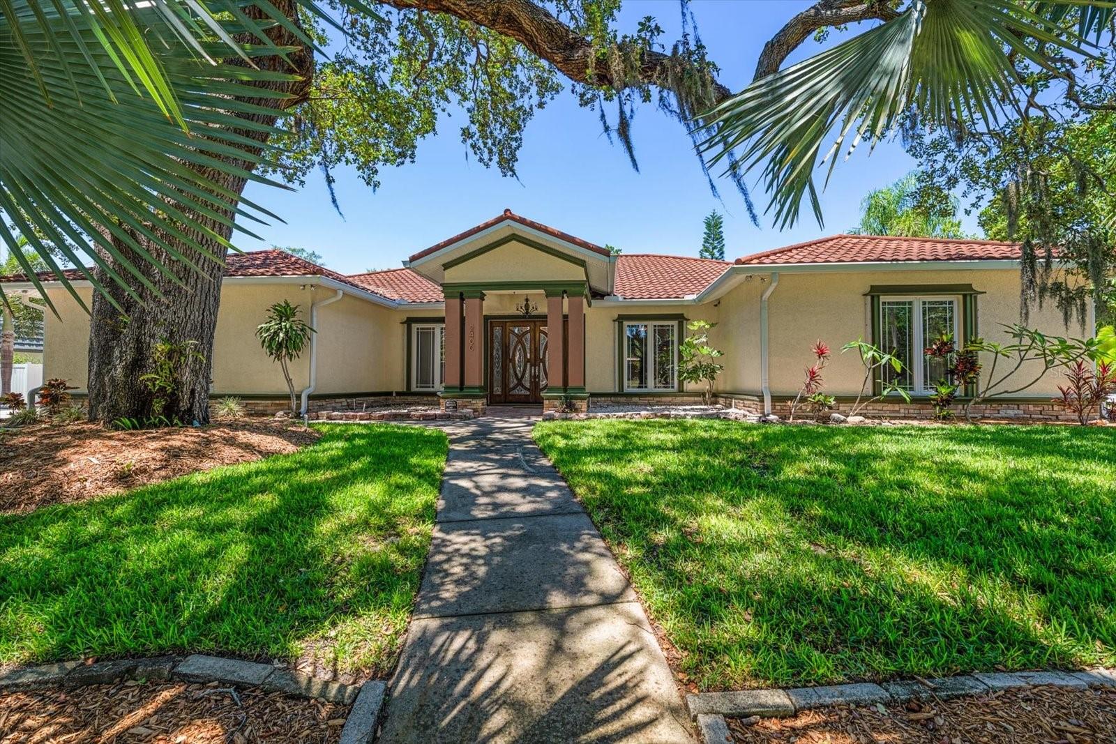 Welcome to this stunning 4 bedroom, 3.5 bath, 3 car garage pool home nestled on a lushly landscaped corner lot in the peaceful and sought-after Sharon Oaks subdivision. Surrounded by towering palms, majestic oak shade trees, frangipani, and fruit bearing mango trees, this property offers a private tropical setting. 
A covered brick paver front porch welcomes you to beautiful double doors. Step inside to soaring vaulted ceilings, skylights, and an abundance of natural light that fills the open-concept design with warmth and elegance. From the moment you enter, the home feels spacious, inviting, and perfectly designed for both everyday living and entertaining.
At the heart of the home is the incredible chef’s kitchen featuring a massive granite island with prep sink, tiered granite breakfast bar with pendant lighting and bar seating, endless cabinetry, granite countertops, and SS appliances. Cooking and entertaining are effortless with double wall ovens, a gas range, and two Bosch dishwashers. A large skylight brightens the space, while a convenient pass-through window connects seamlessly to the backyard pool deck for easy indoor-outdoor entertaining.
Flowing directly from the kitchen is the aptly named great room — an expansive gathering space with soaring vaulted ceilings accented by three skylights. A wall of pocketing sliding glass doors opens effortlessly to the pool deck and outdoor living areas, creating the perfect blend of indoor comfort and outdoor relaxation. The cozy gas fireplace adds warmth and charm, making this space ideal for entertaining or quiet evenings at home.
Perfectly connected to the open living spaces is the formal dining room, while the adjoining library offers a quiet retreat. Designed with a desirable split-bedroom floor plan, the spacious primary suite serves as a private sanctuary with an impressive walk-in closet and luxurious spa-inspired en suite bath. Relax in the Kohler SOK heated jetted tub or enjoy the enormous two-sided walk-in shower. The en suite also features a separate water closet complete with a bidet.
On the opposite side of the home, two additional bedrooms (bedrooms 2 & 3) share a Jack and Jill bathroom, with bedroom 2 featuring French doors that open directly to the backyard pool deck. The fourth bedroom is conveniently located near a separate full hall bath, making the layout ideal for family and guests alike.
Just off the kitchen, a thoughtfully designed hallway includes a half bath, spacious laundry room with pool deck access, and an additional door leading to the garage side of the home.
The side-facing 3 car garage is currently outfitted with 25’x20’ of installed rubber flooring and an additional 10’x20’ of workshop/storage space and is complemented by an extra-long and extra-wide driveway with ample parking space for at least 8 vehicles. One garage door is extra high to accommodate a lift or boat, and the garage features hurricane-rated doors and openers. The extended driveway continues to a double-gated vinyl fence leading into the backyard, perfect for boat trailer storage.
The tropical backyard oasis invites you to relax beside the sparkling screened pool and spa, surrounded by mature landscaping that creates a peaceful retreat right at home.
Located in the desirable Sharon Oaks community, this exceptional property offers the perfect blend of comfort, elegance, and Florida living at its finest. ELEVATION 23’ ABOVE SEA LEVEL.  NOT IN A FLOOD ZONE.