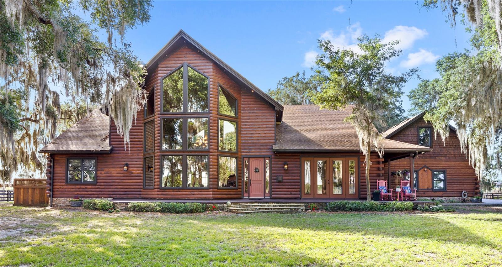 Welcome to The Cedar Island Estate at Arrowtree Reserve, a truly rare offering where the absolute privacy of a secluded “island” setting meets a privately gated equestrian property. Situated at the terminus of a private, dead-end drive, 10925 Arrowtree Boulevard encompasses five high-and-dry acres completely encircled by protected Florida wetlands and ancient cypress, creating a natural sanctuary where your only permanent neighbors are sandhill cranes and the gentle rustle of palms. A 650-foot private driveway, secured by a gated intercom entry and framed by lighted stone columns, winds beneath a shaded canopy of sycamore and 100-year-old oaks, setting the tone for this extraordinary custom builder’s estate. Fully fenced with premium aluminum and four-board fencing, the grounds showcase a picturesque “Florifonia” landscape of rolling hills and lush oak hammocks. Designed with both equestrian and lifestyle versatility in mind, the property features a fully equipped 4–5 stall barn with concrete matted flooring, Nelson automatic waterers, a hot and cold wash rack, private office, tack room, half bathroom, and laundry, alongside a clay-base round pen and three grassed, fenced paddocks, two of which are irrigated. For collectors, hobbyists, or entrepreneurs, a detached, insulated, and air-conditioned oversized two-car workshop provides the perfect climate-controlled environment for a car collection, woodworking, or creative pursuits. High-speed fiber optic connectivity extends throughout the entire property, including the barn. The residence itself is a six-bedroom, three-full bath and one-half bath Western Red Cedar split-log home, blending rustic elegance with grand scale. Inside, soaring 30-foot tongue-and-groove pine ceilings elevate the sunken living room, anchored by a dramatic stacked-stone wood-burning fireplace. The primary suite is a true retreat, complete with its own gas fireplace and an oversized sport shower with dual heads. The gourmet kitchen features granite countertops and flows effortlessly into expansive entertaining spaces, including a game room outfitted with a custom bar and an Olhausen pool table. A private in-law suite positioned over the side-loading 3-car garage is offered with its own entrance and living area. This space is ideal for guests or multi-generational living. Outdoors, a paver patio invites you to fully immerse yourself in the surrounding preserve, where bald eagles, ospreys, and roseate spoonbills are frequently spotted, reinforcing the property’s designation as a true nature sanctuary. Ideally located in the heart of Lake County’s renowned riding and birding country, with nearby access to trails such as the Florida Scrub-Jay Trail, this estate offers a lifestyle that is both peaceful and connected. The Cedar Island Estate is more than a home. It is a private retreat defined by land, craftsmanship, and an unmatched connection to nature. The location is also conveniently located to Downtown Winter Garden and Minneola. The FL-turnpike offers easy access to Orlando and MCO airport. The home is located only minutes to Montverde Academy, as well as other nearby schools. Call today to schedule a private tour.