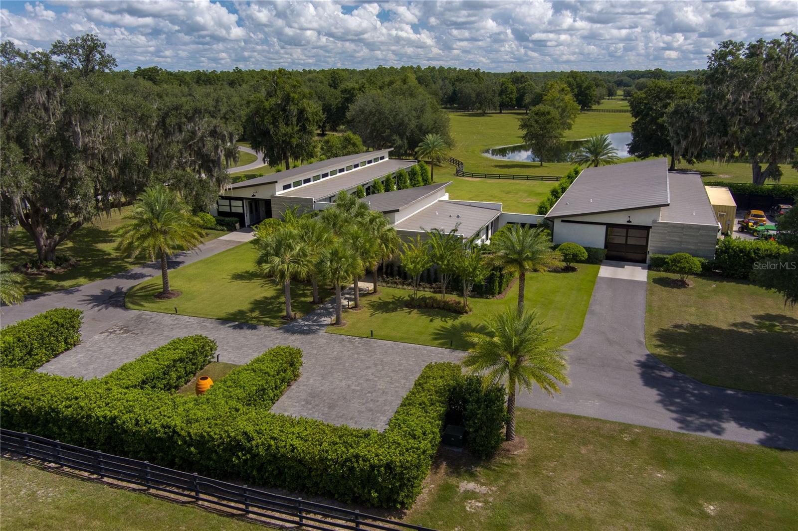 Tucked away on approximately 131 acres and just 10 minutes from HITS and 15 minutes from the World Equestrian Center, this private horse farm offers a refined equestrian setting with thoughtful design and timeless character. Fully fenced and framed by mature oak canopies, the property is enhanced by manicured landscaping, elegant palm trees, rolling green pastures, and a small pond, all introduced by a striking gated entrance that sets the tone upon arrival. The residence sits at the heart of the farm, flanked by barns on either side, creating a balanced and functional layout. A European-style barn includes 12 stalls, a tack room, and a wash bay, while the second barn serves as an equipment barn and features a feed room, dedicated office space, kitchenette, full bathroom, and laundry area, providing excellent support for daily farm operations. Surrounding paddocks are thoughtfully arranged and fully fenced, equipped with run-in sheds, offering comfort and convenience for horses throughout the property. Inside the home, the living room flows seamlessly into a wine and bar area, enhancing the home’s natural flow and social spaces. The open kitchen offers updated appliances and abundant cabinetry, while the two-bedroom, two-bathroom layout includes walk-in closets and sliding glass doors in each room, allowing natural light to pour in and creating a seamless connection between the indoors and the surrounding landscape. A distinctive open back porch with a seating area provides the perfect vantage point to unwind and take in the peaceful farm views, making this property a rare opportunity to own a serene equestrian retreat.