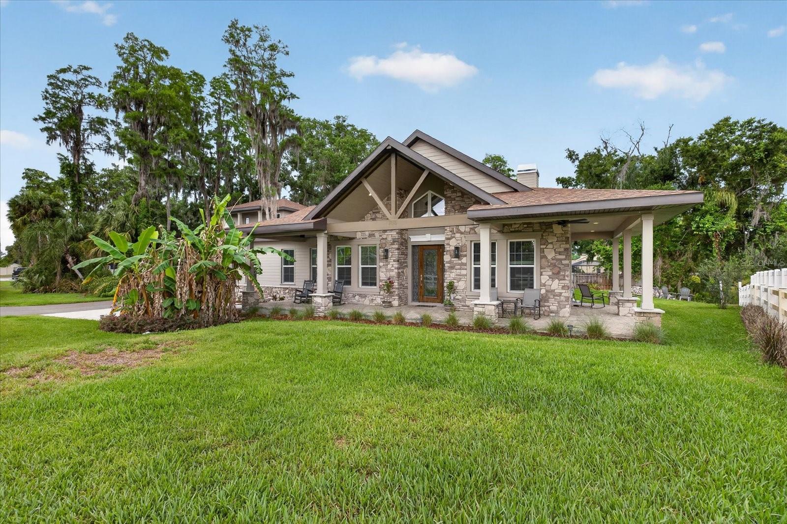 There's a rare kind of home that stops you the moment you step inside — one that feels like it was lifted from the misty ridges of the Georgia mountains and set beside the shimmering waters of Florida. That home is 1208 Sunset Lane, Lutz.
From the stacked stone exterior and sweeping wraparound brick paver porch to the soaring vaulted ceilings and hand-hewn exposed wood beams within, 1208 Sunset Lane is a masterfully crafted new construction estate where mountain lodge romance meets Florida living.
The main home offers 2,926 sq ft under air  of thoughtfully designed living space with 3 bedrooms and 2.5 baths. A stunning floor-to-ceiling stacked stone fireplace anchors the great room, flanked by expansive glass doors that dissolve the line between indoors and out. Dramatic beamed ceilings, rich architectural detailing, and natural light flooding through impact-rated windows create an atmosphere that is simultaneously grand and deeply warm.
A true chef's kitchen built for those who entertain with intention. Solid wood 42" shaker cabinetry, quartz countertops, an oversized stacked stone island, gas cooktop, designer vent hood, walk-in pantry, and a dedicated beverage station with wine refrigeration — every detail curated for elevated everyday living.
The primary suite is your personal sanctuary. A freestanding soaking tub, dual-entry rainfall shower, designer tile work, dual quartz vanities, and a built-in office nook compose a retreat worthy of the finest boutique inn.
Above the garage, you will find a a private 675 sq ft suite with a full bath that offers endless flexibility — guest quarters, home office, gym, creative studio, or income-producing rental. Separate, private, and beautifully appointed.
From the great room, you step outside to a resort-inspired screened lanai, heated pool and spa, outdoor kitchen and expansive  entertaining areas — all set against a tranquil backdrop of mature oaks and natural Florida landscape. With direct canal access to 36-acre Sunset Lake, kayaking and fishing are simply part of the lifestyle.
Built Smart with a tankless water heater, smart home technology, blown insulation, private well and septic, and impact-rated PGT windows that deliver energy efficiency alongside luxury-level comfort.
Minutes from Downtown Tampa, Tampa International Airport, I-275, and Veterans Expressway — yet enveloped in the kind of stillness and natural beauty you'd expect to find deep in the Georgia highlands. This is mountain soul meets Florida sunshine. And a lifestyle that cannot be replicated.  The craftsmanship and high-end finishes found throughout this home — from the hand-hewn beams and stacked stone to the designer tilework and custom cabinetry — simply cannot be found in new construction at this price point. This is mountain soul meets Florida sunshine. And a lifestyle that cannot be replicated.