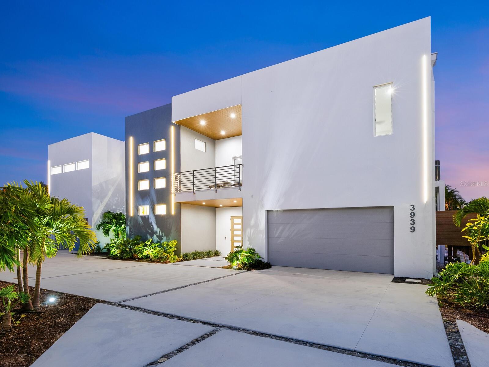 Now Offered At a Refined Price — Modern Siesta Key Living. Set on the north end of Siesta Key, this striking modernist residence offers the rare balance of island serenity and seamless access to the mainland, placing vibrant downtown Sarasota, Southside Village, and the area’s cultural and dining destinations just minutes away—while the azure waters of the Gulf of Mexico and Siesta Key’s world-famous white quartz sand beach are equally close at hand.

Designed with crisp architectural lines and a light-filled, contemporary aesthetic, this nearly 3,800-square-foot, four-bedroom, four-bath home redefines modern coastal living. An open floor plan, 12-foot ceilings, and expansive walls of impact-resistant glass windows and doors create a natural flow throughout the home, blurring the line between indoors and out while capturing the relaxed elegance of island life.

A dramatic natural rosewood floating staircase serves as a sculptural centerpiece, leading to the main living level where modern design and functionality converge. The living area is anchored by a 100-inch electric floating wall and linear fireplace, creating a striking focal point for both everyday living and entertaining. Modern LED lighting, integrated throughout the interior and exterior, enhances the home’s clean architectural lines and evening ambiance.

The open-concept kitchen is sleek and refined, featuring premium appliances, a natural gas cooktop, contemporary cabinetry, and generous prep and gathering space—ideal for entertaining or relaxed daily living. The primary suite is a tranquil retreat, highlighted by a spa-inspired bath with LED anti-fog mirrors, a 74-inch soaking tub, and a walk-in closet, along with direct access to outdoor living. Three additional guest suites are thoughtfully designed to offer comfort, privacy, and flexibility.

One of the home’s most distinctive features is the private balcony with spa-style hot tub, offering views to both the front and rear of the home—perfectly positioned for morning relaxation, evening unwinding, or enjoying coastal breezes after a day at the beach. The property also offers ample room to add a pool, allowing for future customization of the outdoor living experience.

Elevated and thoughtfully constructed in accordance with current building standards, the residence offers peace of mind without compromising design. Beneath the home, an exceptionally expansive garage and storage level accommodates 12 or more vehicles, a rare and highly sought-after feature on Siesta Key. This level also includes a separate flex room with an overhead door that opens directly to the backyard, ideal for a private home gym, wellness studio, hobby space, or additional entertaining area.

Just a short stroll away, a charming neighborhood beach at Big Pass provides a front-row seat to boats gliding through the pass and colorful sunsets each evening—a hidden gem that captures the unique coastal energy of the north end of Siesta Key.

This is a compelling opportunity for buyers seeking a move-in-ready modernist home on Siesta Key’s coveted north end—where convenience, coastal beauty, and architectural sophistication come together, and where the beach, boating, dining, and Sarasota’s vibrant cultural scene are all within easy reach.

A refined blend of modern design, prime location, and lifestyle flexibility, this residence delivers an exceptional Siesta Key experience.