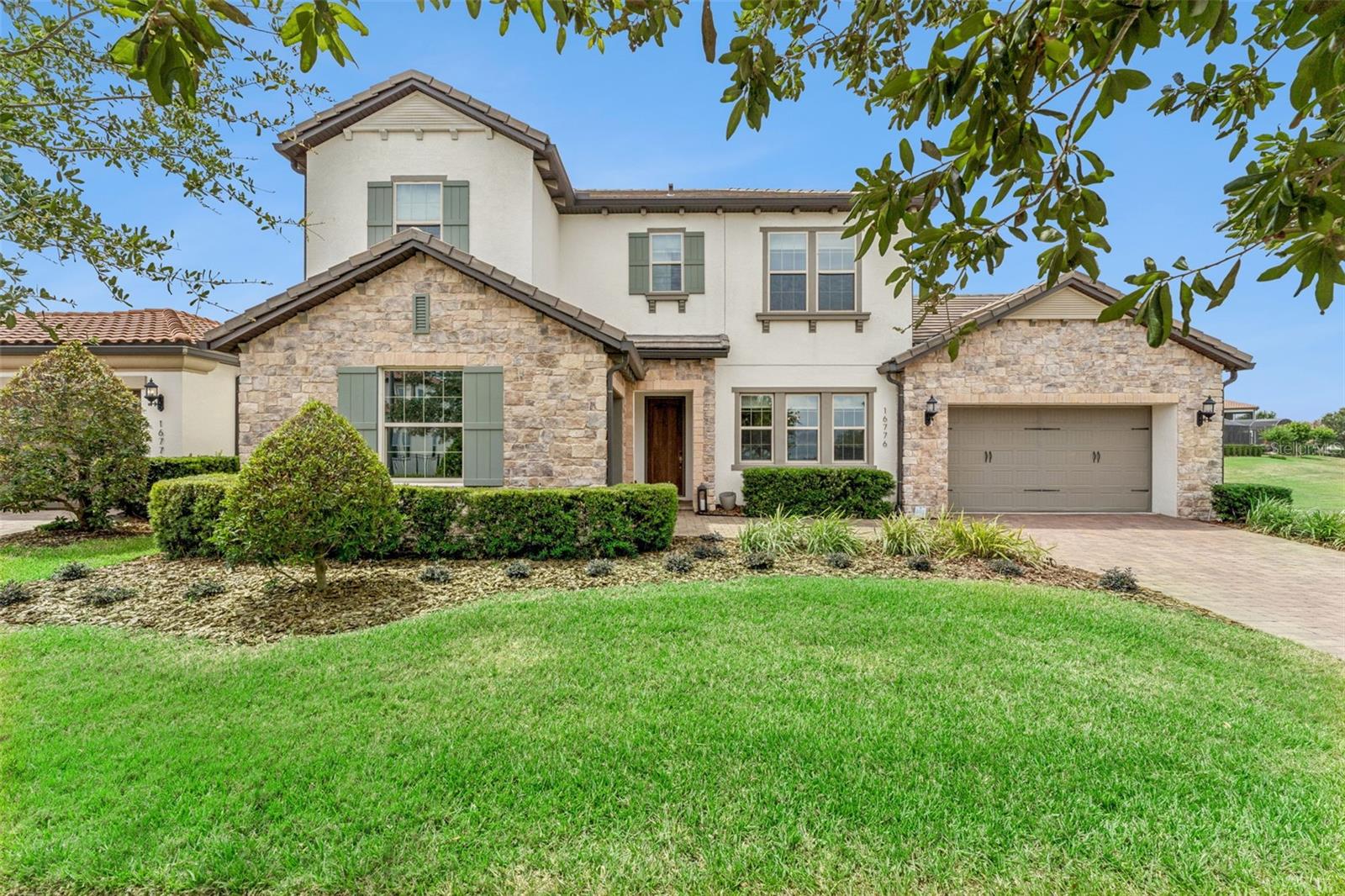 Positioned on a premium homesite with an expansive manicured common area along one side, this property offers added privacy and open space, along with sweeping views of John’s Lake from the front of the home. Inside, the home opens to a formal dining area accented by wood beam ceilings, while custom wall details in the foyer and along the staircase add a refined, designer touch. The main living area features soaring ceilings, abundant natural light, wood beam ceiling accents, and a striking floor-to-ceiling accent wall, creating a dramatic yet inviting focal point that flows seamlessly into the dinette and open kitchen. Designed for both everyday living and entertaining, the kitchen includes a large island with seating, sleek cabinetry, stainless steel appliances, a gas cooktop, built-in oven, and generous pantry space. Just off the pantry, a connecting space between the kitchen and dining room offers the perfect opportunity for a coffee station or butler’s pantry. The main level also offers a spacious primary suite with a well-appointed bath and a custom walk-in closet featuring built-in drawers, cabinetry, and shelving, along with a secondary bedroom and full bath, ideal for guests or multigenerational living. Upstairs, you will find three additional bedrooms, including one with a private bath, while the remaining two share a full bath, plus a generous loft overlooking the living area that provides flexible space for a secondary living area, home office, or play space. The outdoor living space is designed for true Florida living, featuring a saltwater pool and spa added in 2021 with full automation, expansive Travertine tile decking, and a lanai with a motorized screen that extends your living space year-round. The patio is also pre-plumbed for a future outdoor kitchen, offering even more potential for entertaining. Additional highlights include a split three car garage configuration with a separate side entry one car bay and a 2 car garage equipped with an EV charging outlet. Waterside on John’s Landing offers a clubhouse, fitness center, resort-style pool, playground, covered dock, and pavilion on John’s Lake, all conveniently located near Horizon West, Hamlin, shopping, dining, and major roadways.
