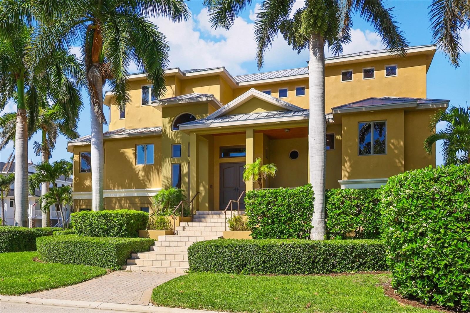 Experience refined waterfront living in the exclusive gated enclave of Hawks Harbor. This custom-built 2013 estate offers 106 feet of canal frontage and over 8,500 total square feet, seamlessly blending architectural elegance with effortless coastal luxury. A private elevator connects all levels—from the expansive six plus-car garage to a stunning main living area defined by soaring 20’ coffered and tray ceilings, crown molding, and abundant natural light through Anderson impact-rated windows and doors. A striking gas fireplace and built in cabinetry anchors the space, while French doors open to 40’ x 11’ covered outdoor living designed for year-round entertaining. The gourmet kitchen is both functional and sophisticated, featuring stone countertops, upgraded cabinetry, and high-end SubZero and Wolf stainless appliances—ideal for culinary enthusiasts and hosts alike. The primary suite is a true retreat, offering direct access to the covered lanai overlooking the saltwater pool, natural gas tiki torches and lush tropical landscape. The spa-inspired bath includes a soaking jetted tub, multi-head walk-in shower, dual vanities, and an expansive custom walk-in closet. Remote operated Hunter Douglas Nantucket 3” Shades grace all of the main living level windows.  Three additional bedrooms, including a second primary suite, and a loft space upstairs provide exceptional comfort and privacy, while dual laundry rooms on both levels add convenience. Outdoors, a resort-style setting awaits with a private dock and 14,000 lb boat lift, offering direct access to Sarasota Bay and the Gulf waters beyond with endless sunsets. Enjoy effortless boating to the shores of Longboat Key and nearby waterfront dining. Built for durability and efficiency, the home features a standing seam metal roof, tankless gas water heater with booster, natural gas, an oversized garage with room for all of your toys and a separate storage or exercise room with a mini split AC. Ideally located between Bradenton and Sarasota with convenient access to the renowned IMG Academy, Sarasota-Bradenton International Airport and top-rated Gulf Coast beaches. A rare opportunity to own a private, luxurious waterfront estate in one of the area’s most affordable and sought-after boating communities. This is more than a home—it is a statement of lifestyle and luxury.