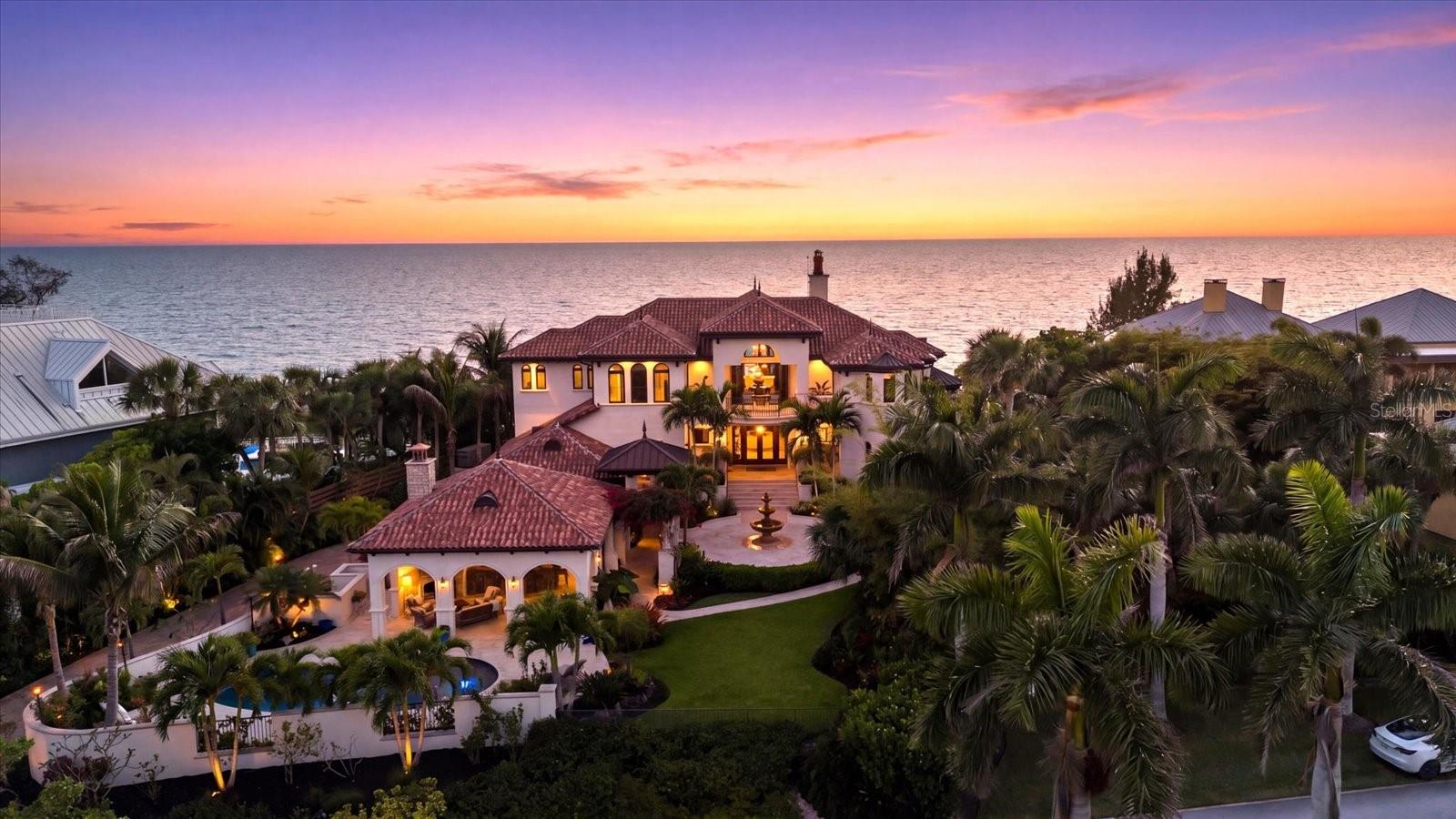 Where the first light of dawn shimmers across the Intracoastal and the glow of sunset melts into the Gulf, this is a once-in-a-generation Gulf-to-Bay estate of uncompromising beauty and distinction. Gracefully positioned on approximately 1.1 acres along the gated north end of Manasota Key, this masterfully curated waterfront compound embodies refined coastal living with private beach access and a bayfront dock and lift. The property offers a balance of serenity and an elevated boating lifestyle. Expertly built by KIMCO and created by Suncoast, the main residence spans 5,839 sf of living space, and the guest house offers 1676 sf. Constructed of concrete at a high elevation with impact-rated windows, with no water intrusion in the main house. Car enthusiasts will appreciate accommodations for 9 vehicles. A tropical, fenced approach leads to an elegant welcome with a private courtyard entry, tranquil fountain, stone steps and bespoke wrought-iron doors. Inside, marble inlays, curated finishes, and sweeping Gulf-to-bay vistas. The great room is a dramatic expression of scale and artistry, crowned by a soaring 35-foot Cypress ceiling, and a two-story curved wall of glass framing panoramic Gulf views. Baccarat chandeliers illuminate the space, anchored by a striking see-through fireplace. The adjacent living salon continues the narrative with a hand-carved marble fireplace, rich mahogany ceiling detail, and bespoke millwork. The culinary suite is both functional and exquisite, showcasing dual islands, exotic stone surfaces, custom cabinetry, paneled Sub-Zero refrigeration, a range hood with brass accents, a Wolf cooktop and double ovens, and a paneled dishwasher, complemented by a butler’s pantry and designer laundry. Formal dining unfolds against sweeping Gulf views. A refined, first-floor guest suite offers exceptional comfort. Two office suites, each with the ability to serve as guest accommodations, offer distinct character:one light-filled with elegant detailing and custom built-ins, the other richly appointed with wood paneling, coffered ceilings, and an onyx-clad full bath. The primary suite is a private sanctuary with a Gulf-front Juliet balcony, intricate cypress ceiling, and a spa-inspired bath featuring Waterford chandeliers, a soaking tub, exquisite marble flooring, and mother-of-pearl adorning the ceiling. An elegant and boutique-style dressing gallery completes the suite. Outdoor living is elevated to an art form with expansive Gulf-front terraces beneath a rotunda-style copper roof, cypress ceilings, and travertine flooring. The pool with LED lighting features a sun shelf, lounging areas, a full bath, and outdoor shower. A fully equipped outdoor kitchen pavilion showcases a custom copper hood, natural stone surfaces, appliances, and a fireplace. The guest house offers unobstructed Intracoastal views, a full kitchen, living room, 2 baths, and a private bedroom, with expansive pocketing doors opening to a scenic balcony. The ground level provides space for vehicles, and a half bath with direct dock access. Boating amenities include approximately 6' of deep water, a 10,000-pound lift, and an updated dock. Modern systems have been meticulously integrated, an elevator, a generator, propane, Starlink internet, intercom, and well for irrigation. Tropical landscaping and a preserved Cuban Laurel enhance the private setting. A rare legacy estate offering architectural excellence, resilience, and an unparalleled Gulf-to-Bay lifestyle.