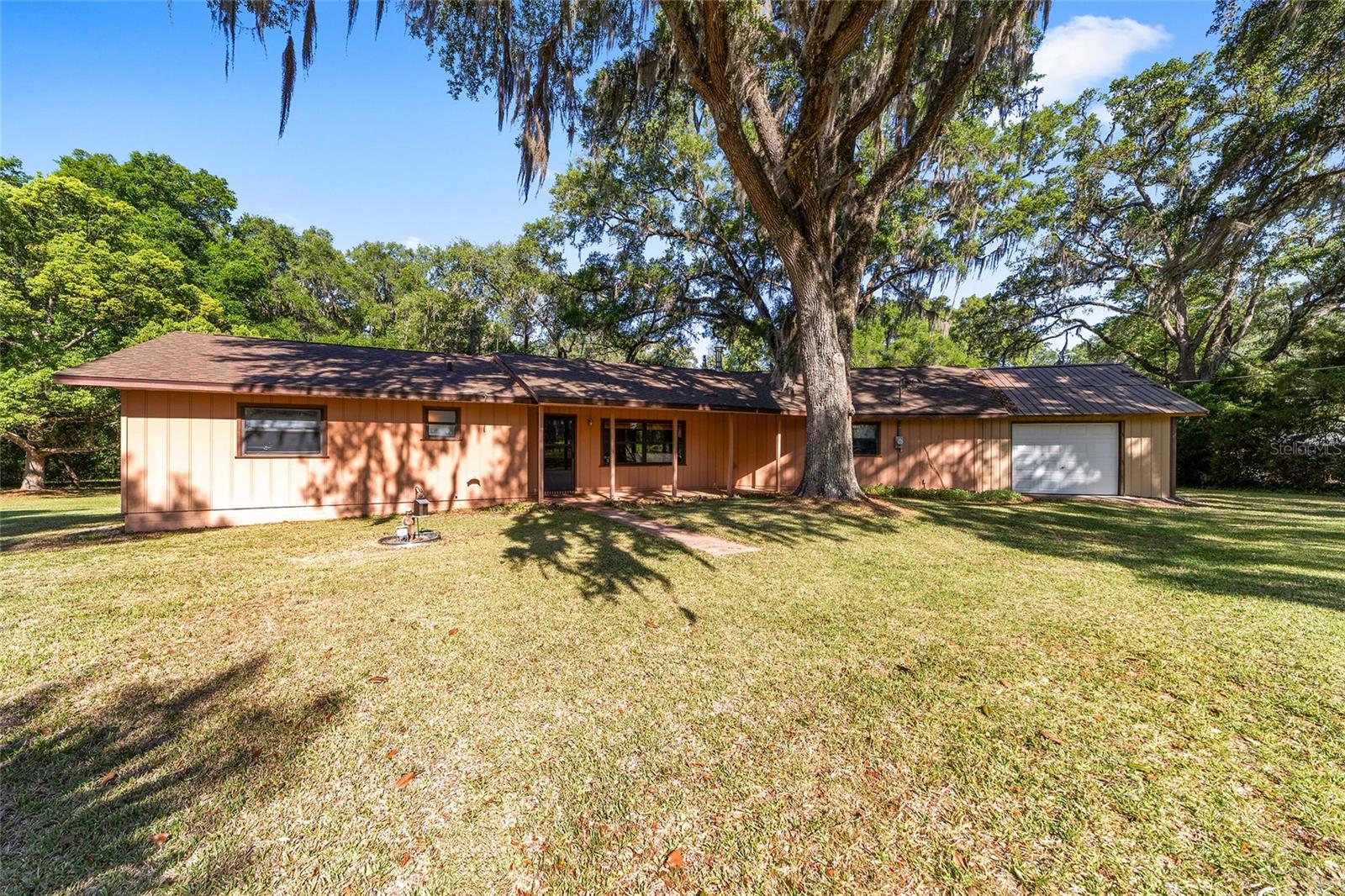 GREAT LOCATION, Tucked beneath a canopy of majestic trees on scenic NW 160th Avenue, this beautifully situated 2-acre property captures the peaceful charm that draws so many buyers to the Ocala countryside. Surrounded by picturesque farms and rolling natural beauty, this inviting 3-bedroom, 1.5-bath home offers the perfect balance of privacy, comfort, and location for those dreaming of the equestrian lifestyle without the expense or upkeep of a large farm. Ideally positioned between Ocala and Williston, with both HITS and the World Equestrian Center just down the road, this property makes an exceptional full-time residence, seasonal retreat, or winter escape.  Inside, the home feels warm, welcoming, and filled with natural light. The spacious living room opens into a separate dining area where sliding glass doors frame breathtaking views of the mature trees and lush landscape beyond. Every window brings in the beauty of the property, creating a calm and grounded atmosphere throughout the home. The kitchen offers generous counter space for cooking and entertaining, along with a large pantry for additional storage, while the nearby back deck invites relaxed outdoor dining under the trees and Florida skies.
The thoughtfully designed split floor plan offers privacy and flexibility, with two comfortable guest bedrooms on each side of the home and the primary bedroom with a walk in closet and bath tucked next to the guest room. Adjacent to the primary suite is a one-car garage with ample space for tools, equipment, golf carts, tack, or weekend adventure gear.  This is an exceptional property for the buyer looking for a little slice of heaven.