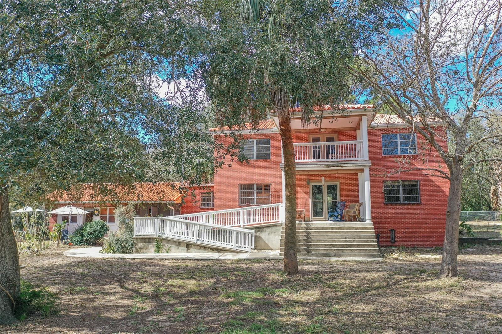 Built to last, this cement block and brick home offers 6 bedrooms and 4 bathrooms, constructed from floor to roof for lasting strength and peace of mind. A classic tile roof crowns the home, while original hardwood floors throughout the main residence add warmth, character, and timeless appeal.

Set on 10 fully fenced acres with three separate pastures, the property is ideal for animals, privacy, or simply enjoying wide-open space. Mature trees provide natural shade and a peaceful setting, and the large front porch is perfect for relaxing and taking in the surroundings. A screened-in in-ground pool is currently covered and not in use, offering future potential for outdoor enjoyment.

The main floor features a spacious great room ideal for gatherings, along with the primary bedroom and en-suite bathroom for convenient single-level living. The second floor includes additional living space, bedrooms, a bathroom, and a kitchenette, plus two separate balconies with water views—perfect for guests or multi-generational living.

The walk-out basement was previously a fully self-contained 2 bedrooms, 1 full bath and shower apartment complete with an open kitchen and living area, two bedrooms, and two bathrooms, providing excellent flexibility for extended family, guest accommodations, or rental income.

Additionally, this home includes a whole home 24k Generac that powers the whole house, guest cottage and barns. 

Additional highlights include a detached guest house with high ceilings and an open-concept layout, as well as a detached barn with water, electricity, two stalls, and ample storage.

While the property does require some TLC, it presents tremendous potential for customization, restoration, or value-add improvements—an exceptional opportunity for those seeking acreage, privacy, and long-term upside.