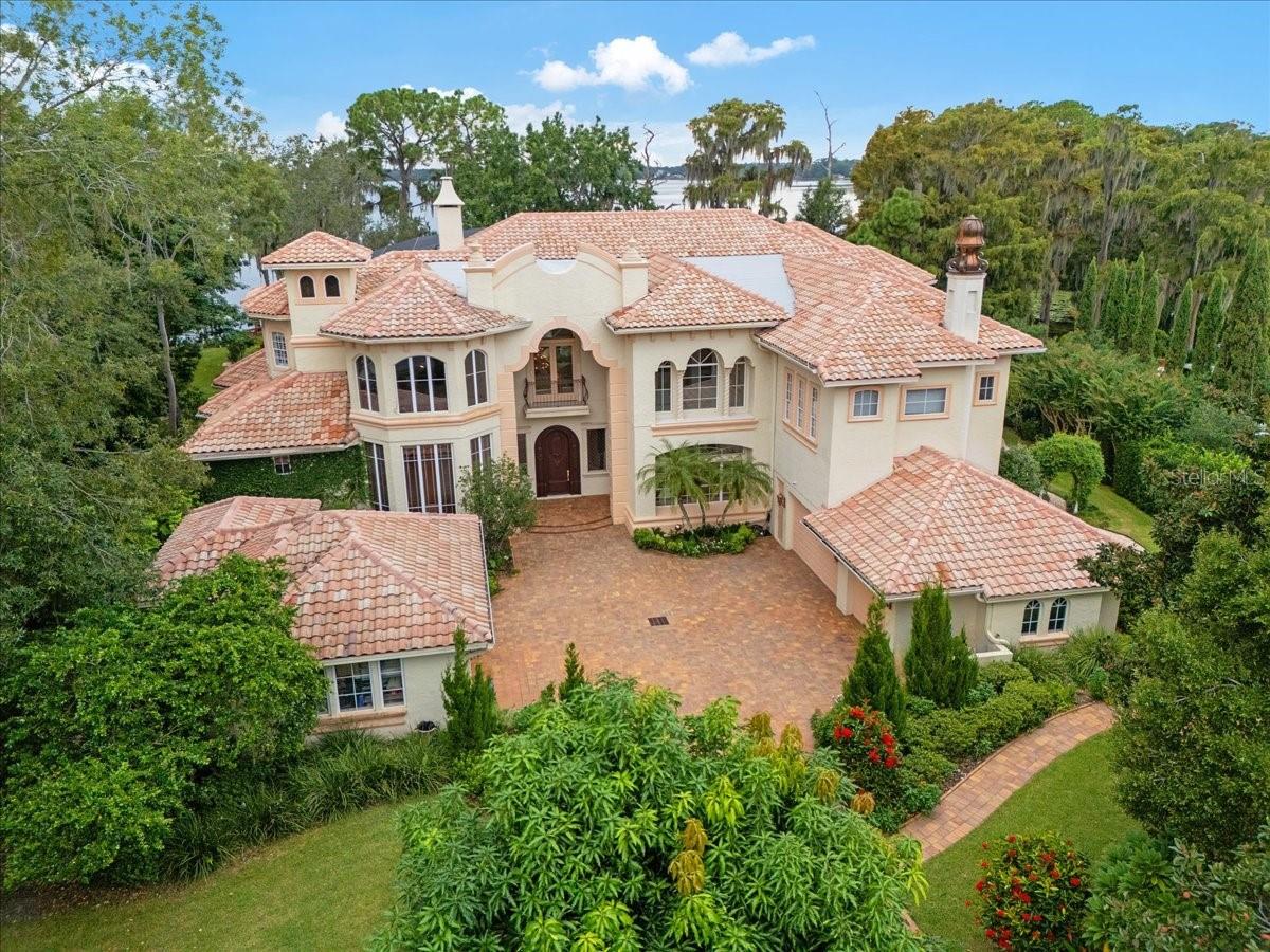 WELCOME TO JARDIN CACHÉ! Built by Rial Jones and designed by the world-renowned architect John Henry, this stunning residence is nestled on the shore of Lake Sheen, boasting over 200 feet of pristine lake frontage on a sprawling 1.02-acre lot. Featuring soaring 30-foot ceilings and a grand spiraling staircase, it makes a striking first impression. The heart of the home is a gourmet kitchen, equipped with solid countertops, custom wood cabinetry, a Subzero refrigerator and freezer, a Wolf electric cooktop, and two dishwashers. An oversized walk-in pantry with custom shelving provides ample storage. The formal dining area showcases volume ceilings and second-tier arched windows, perfect for hosting gatherings. The family room offers 180-degree views of the lake and pool through floor-to-ceiling windows adorned with plantation shutters, creating a serene ambiance. A dual-sided Crema Maya stone fireplace  designed by Barbara Tattersfield with custom built-ins serves as a focal point in both the living room and adjacent  master sitting room which features oversized mirrors with stone surrounds. Retreat to the  main floor primary suite, featuring a custom wooden spiral staircase resembling a double helix leading to a secluded loft. The study, with its floor-to-ceiling custom wood detail and built-in bookcases, is perfect for quiet work or reading. Upstairs, each bedroom has an en-suite bath, walk-in closet, and private balcony, offering both luxury and privacy. The bathrooms are elegantly designed, featuring 7 full baths and 1 half bath throughout the home. Step outside to the stunning outdoor space, complete with a summer kitchen, pool with sun shelf, spa, and water features, all surrounded by lush landscaping. Three Trellises and two water fountains enhance the outdoor experience. Paver walkways meander down both sides of the property, one leading to the dock. The boat dock features a ski boat hoist and pontoon boat hoist. The adjacent floating jet dock can accommodate kayaks or jet skis.  5 elegant rock formations in the back yard, planted with various flowers and planting make the property unique. Additional highlights include a spacious mudroom with built-ins, a 5-car garage & home generator. Don’t miss this rare and extraordinary opportunity to own a piece of lakefront paradise in desirable guard gated community located in the heart of Dr. Phillips minutes from famed Restaurant Row and world class theme parks.