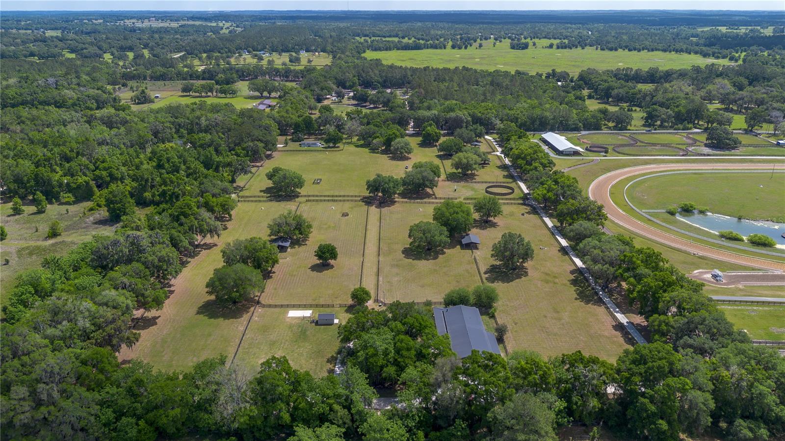 Ideally placed within NW Marion County’s storied horse country, this unique 20+ acre farm is designed with both horse and rider in mind. Enter through one of three gated entrances and follow the full-length concrete drive through a park-like setting shaded by grand oaks and pecan trees. To the south of the farm you can enjoy the sight of thoroughbreds on the training track, with dressage and jumpers alike training across the street—underscoring the property’s appeal for a wide range of equestrian disciplines.  The farm is well-equipped with 7 fenced and cross-fenced paddocks, automatic waterers, and run-in sheds, offering an efficient layout for daily horse care. A 6-stall concrete-block barn with feed room and tack room anchors the equestrian facilities, complemented by a round pen, hot walker, and wide alleyways and riding lanes—ideal for carriage drivers and providing easy access throughout the property. Additional storage buildings, irrigation systems, and established landscaping further enhance the functionality and flexibility of the farm. The primary living space is a well-appointed barndominium-style residence, built in 2005, offering over 2,000 square feet with 3 bedrooms and 2.5 baths in a split-bedroom floor plan. Inside, high ceilings, ceramic tile flooring, and a fireplace create a comfortable and inviting atmosphere. The kitchen is designed for both everyday living and entertaining, featuring abundant cabinetry, granite countertops, an island workspace, and an adjacent dining area. French doors and multiple living spaces open to expansive covered porches, providing seamless indoor-outdoor living and sweeping views of the surrounding pastures.
Directly attached is a comprehensive RV-ready garage with high ceilings and oversized doors, along with a separate 4-car garage with integrated workshop space—ideal for large vehicles, equipment, or hobby use. A well-maintained secondary 1-bedroom, 1-bath guest cottage is also established on the property, offering flexible accommodations for guests, staff, or potential seasonal rental income.
Conveniently located just minutes from Williston and within easy reach of Ocala’s extensive tack and feed options, equine service providers, and world-class veterinary care. HITS is located just 6 miles away, while the World Equestrian Center (WEC) is a scenic 25-minute drive from the farm. This property offers a rare combination of functionality, space, and natural beauty—well-suited for equestrian pursuits or a private country retreat.