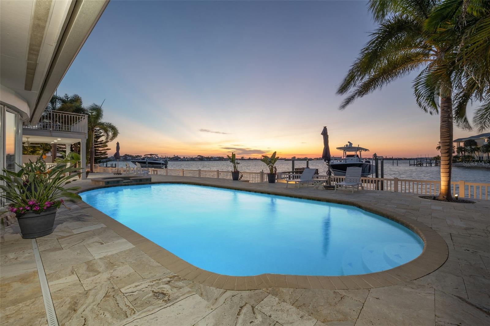 Featuring a privileged setting, this majestic waterfront compound offers spectacular water views and meticulously updated interior features. Exemplifying understated elegance, the timeless design features clean, open spaces that masterfully showcase panoramic water vistas. Featured indoor spaces include an indulgently comfortable formal living room that seamlessly connects to your dining room, a perfect setting for sophisticated gatherings. The open-concept kitchen has stainless appliances, stone countertops, custom cabinetry, and a welcoming breakfast nook, a cherished spot for your morning coffee. At the end of a busy day, make your escape to the master retreat complete with an unrivaled spa-like master bathroom, a large walk-in closet and exceptionally soothing water views. Additionally, the first floor offers a comfortable family room and a private guest suite.  Ascending to the second level, you'll discover a stately bonus room complete with a walk-out balcony. There are three additional bedrooms on this level. Transition out back and relax in your saltwater pool and spa or sit on the stone patio that is perfect for al fresco dining. The dock has a 15,000 pound boat lift and can easily fit a 32 plus foot vessel. When evening arrives, views of splendorous sunsets and colorful skies accompany gentle breezes off the water.  This special property lends itself to entertaining both on and off the water.