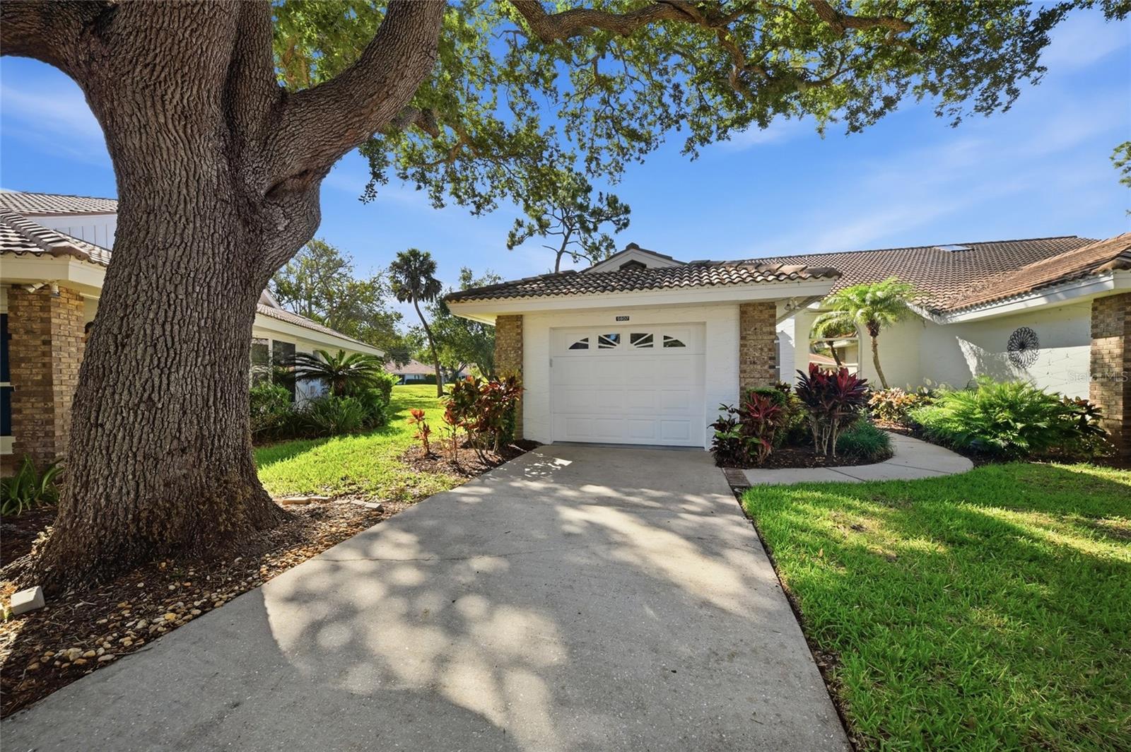 Under contract-accepting backup offers. Welcome to your dream retirement oasis on Lake Natura! This light and bright 2 bed, 2 bath villa sits on a quiet cul-de-sac in the highly sought after 55+ community of Garden Lakes. Perfectly situated near SR 70 and 37th St E, you’re minutes from shopping and dining and less than 15 miles from the coast’s famous white-sand beaches.  Stroll through the perfectly manicured courtyard and enter your very own slice of heaven. A spacious, closet-flanked foyer welcomes you into an airy, open floor plan with vaulted ceilings, where a dramatic wall of windows frames breathtaking, unobstructed lake views.  An entertainer’s dream, this home features a generously sized eat-in kitchen complete with a pantry, abundant cabinetry, a charming bay window, and a large breakfast bar that bridges the kitchen and main living spaces.  Your side patio is the perfect sanctuary to read, entertain or enjoy a quiet cup of coffee by the water. You’ll fall in love with the swaying palms, majestic oaks, and local wildlife that truly capturing that old Florida charm.   Wake up to more sunny lake views in the spacious master suite complete with a sliding glass door that opens directly onto the enclosed lanai. This private retreat boasts both a large reach-in closet and a generous walk-in closet, a dedicated vanity/makeup area, and an en-suite bath featuring a walk-in shower thoughtfully outfitted with safety handrails.  The guest bedroom is bathed in natural light thanks to a large window topped with a beautiful arch window that overlooks the manicured courtyard. The bedroom sits directly adjacent to the guest bath which features a relaxing tub/shower combo with handrails for added safety.  Beautiful plantation shutters outfit nearly every room, with standard mini-blinds completing the guest bedroom. Other features include: Indoor laundry, attic fan in garage, hurricane shutters, ceiling fans in living room and both bedrooms, new washer 2020, new AC 2021 and new water heater 2022. Included appliances: Large Refrigerator, Microwave, Glass Top Stove/Oven, Dishwasher, Garbage Disposal, Washer and Dryer.  Garden Lakes offers a resort-style retirement with a heated pool, tennis/shuffleboard courts, fitness center, library, and a bustling social calendar (from cards to off property outings to monthly potlucks). There’s something going almost every single day. Prefer a quiet afternoon? Stroll the concrete paths under giant oaks or relax on the wooden deck overlooking the lake. This is a place where neighbors are friends and everyone looks after each other.   Can be sold furnished or unfurnished to suit your needs. Don’t let this gem slip away!