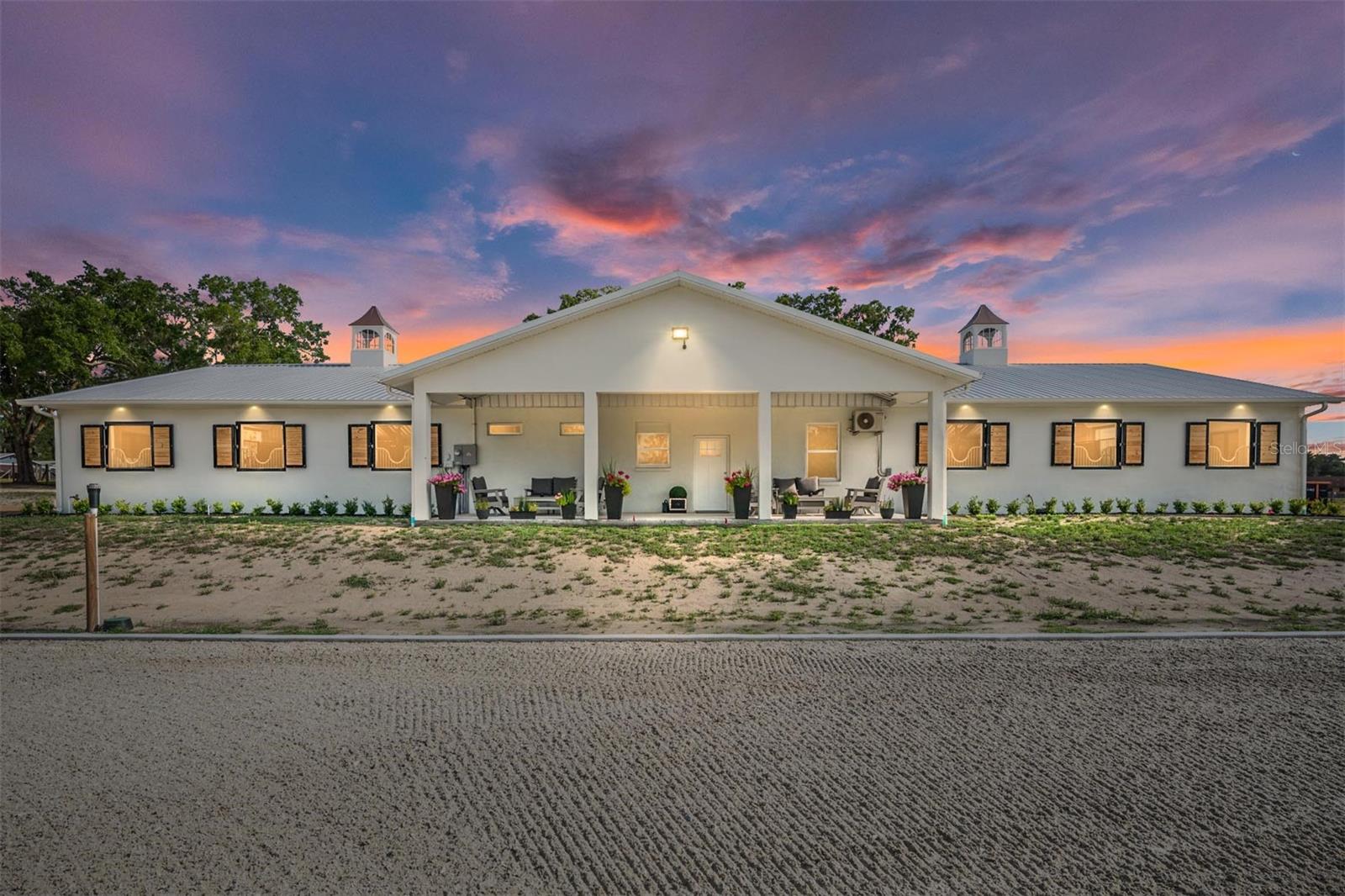 EXCEPTIONAL EQUESTRIAN ESTATE
Positioned directly across from the renowned World Equestrian Center in the heart of Ocala, Florida — the Horse Capital of the World — this extraordinary estate represents a rare opportunity to own a world-class equestrian property at the epicenter of the sport.
Equestrian Facilities
The barn and riding arena were custom built in 2025 by Jim Ballinger of M&W Building Solutions, reflecting the highest standards of craftsmanship and equestrian design. Constructed of solid cinderblock with a double-insulated roof and French drain gutters, the barn is engineered to handle Florida's heavy rainfall while keeping the interior dry and comfortable year-round.
The professional-grade barn features 12 spacious 12' x 14' stalls, each equipped with individual fans, fly spray systems, and automatic waterers. Three cupolas and large industrial overhead fans ensure exceptional airflow throughout. Yoke windows along the aisle and exterior shuttered windows flood the space with natural light while maintaining a classic equestrian aesthetic. Two roll-up end doors and a euro-style slide entrance add everyday convenience for equipment, hay delivery, and vehicle access. The barn is further appointed with two interior wash racks with hot and cold water, a tack room, feed room, laundry room, bathroom, and kitchenette.
Riding Arena & Paddocks
The impressive 150' x 250' all-weather riding arena features a full irrigation system and concrete curb, providing premier footing year-round. Two interconnected water wells — including a dedicated 5 HP well powering arena irrigation — ensure a reliable water supply at all times. Seven irrigated paddocks, freshly reseeded and fully fenced with hot-wired fence boards, offer safe, lush turnout for your entire herd.
Residential Accommodations
The main residence offers 6 bedrooms and 3.5 bathrooms, completely remodeled in 2025 — professionally decorated and furnished by an interior designer with all new appliances — delivering generous spaces for everyday comfort and entertaining. Bedroom views overlooking the barn, arena, and paddocks offer a truly immersive equestrian living experience. Beautifully appointed patio areas extend living space outdoors, perfect for relaxing while taking in the serene surroundings. A newly installed gated entrance and paved parking area offer security and a polished first impression. Multiple dwelling units provide flexibility — ideal for guest quarters, staff housing, multigenerational living, or income-producing opportunities.
Expansion Opportunity
Favorable zoning presents exciting possibilities — including the ability to build an additional residence, plus dedicated structures for hay storage and equipment. Whether expanding the operation or creating a multigenerational compound, the groundwork is already in place.
Location
At the heart of Ocala's premier equestrian corridor, this estate places you steps from the World Equestrian Center — whether you're an active competitor, dedicated breeder, or someone who appreciates the finest in equestrian living, this location puts you at the center of it all.