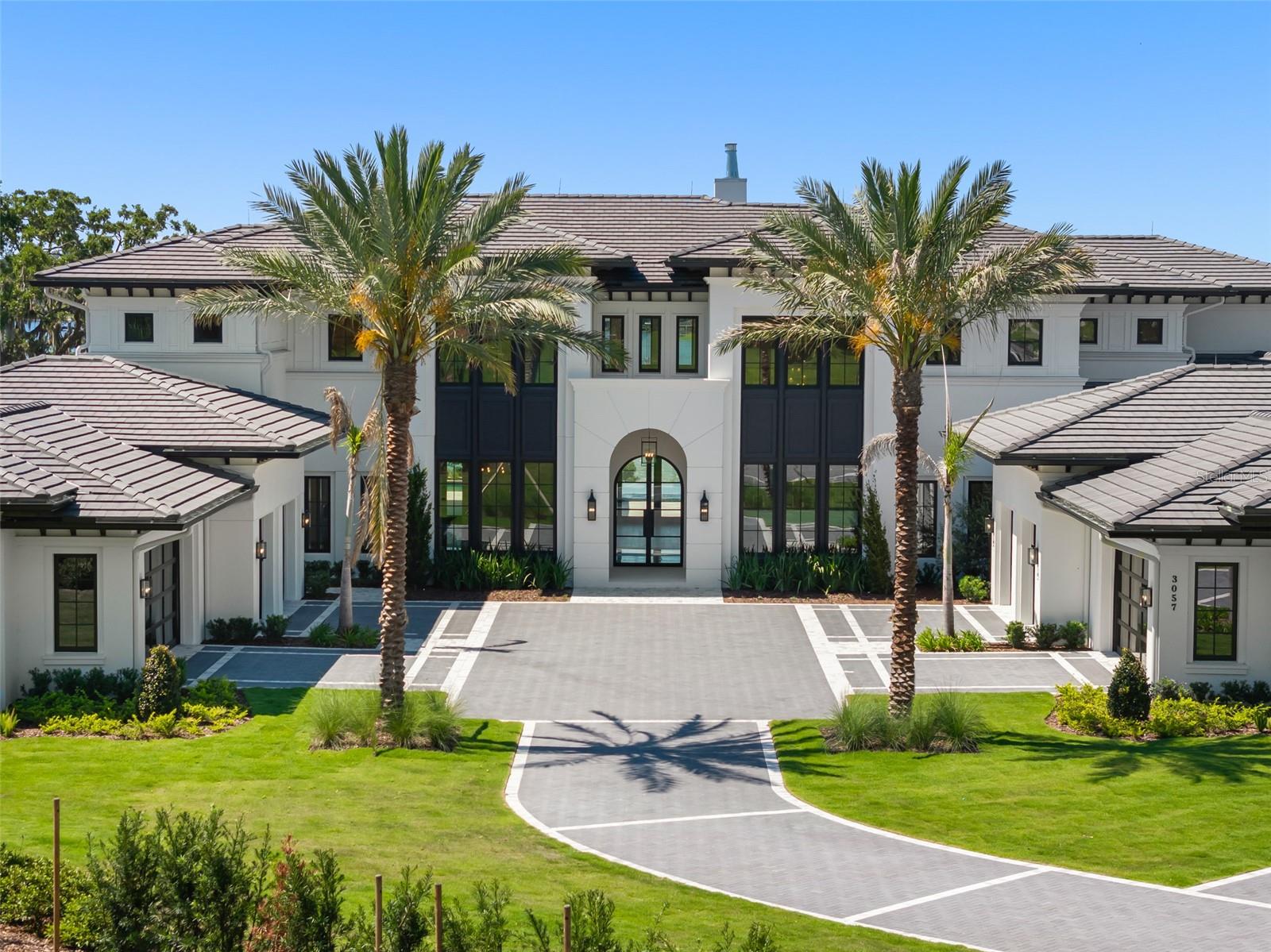 BRAND NEW ESTATE. A truly exceptional one-of-one on the shores of Lake Down, boasting over 12,000SF, 6BR's, 6/5BA's, and unmatched multigenerational flexibility. Designed by Mark Nasrallah and curated by Sorenson Construction, every inch of this estate was crafted with intention and the finest materials.
Two 4-car garages flank either side of the oversized motor court, offering private entry to both the main house and the attached guest house. Off the main foyer, you'll find the formal dining room with Calacatta marble floors, and geometric coffered ceiling. Just beyond the elevator lies a 17x19 laundry room with an expansive island. The east wing is home to the gourmet kitchen, breakfast room, and family room. The chef's kitchen includes a Wolf six-burner gas stove with a built-in range hood, stacked double oven, and Sub-Zero double-wide refrigerator. Two Calacatta Macchia Vecchia marble islands create the ultimate statement. Beyond the main kitchen, behind a hidden door, is the prep/messy kitchen, with a Monogram 4-burner gas stove, Bosch refrigerator, walk-in pantry and butler's pantry. On the opposite side of the kitchen, the spacious breakfast room is bathed in natural light with access to the summer kitchen and pool deck through glass sliding doors. The open-concept layout flows effortlessly to the family room, where a backlit, custom media wall offers endless entertainment options. At the center of the main house is the expansive living room, the heartbeat of the estate. From the backlit coffered ceilings to the handcrafted millwork, and an overwhelming wall of glass, every part of this room feels larger than life. Rich hardwood flooring, built-in bookshelves, and a custom brass fireplace make it feel as charming as it is expansive. For guests, there is a first-floor ensuite bedroom complete with a separate generous lounge room, all overlooking spectacular lake views.
Beyond the custom iron staircase on the first floor is the executive office, with built-in library, wood desk, and beautiful herringbone flooring. Adjacent is a stunning powder bath, followed by the interior guesthouse entry, which opens to a generous living room, a full-size kitchen with a Wolf 6-burner gas stove and a beautiful Arpell Azul mosaic backsplash, its own prep/messy kitchen, and full butler's pantry. The guest house's primary suite is its own oasis, with sweeping lake views, an ensuite bathroom, double vanity, clawfoot tub, and a huge walk-in closet. Two additional ensuite bedrooms — one designed for staff — a full-sized laundry room, and a flex room complete the guest house.
Upstairs, the primary suite spans the entire east wing, with handcrafted coffered and backlit ceilings that are mesmerizing, plus panoramic views of Lake Down from the balcony. The master ensuite bathroom boasts a freestanding massage bath, his-and-hers vanities, and Walden Onyx designer wall coverings. The immersive primary walk-in closet will simply take your breath away, featuring designated his-and-hers areas, a center island, custom-built-in cabinetry, and an adjacent laundry room for the upper level. Directly next to the primary suite lies a spa retreat with a sauna room. A media room and entertainment den complete with its own kitchenette boast a flex room directly across the hall as well as an oversized ensuite guest suite.
Outside, the limestone pool deck & covered summer kitchen, the disappearing-edge pool and spa with retractable screens provide the perfect retreat.
