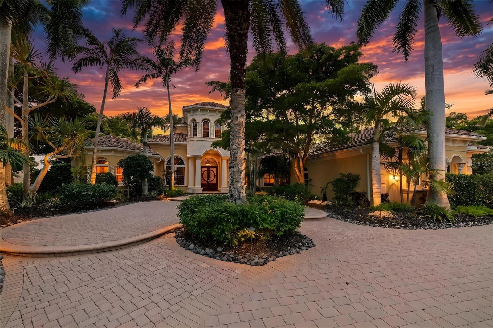 Set on more than half an acre with sweeping golf course views, this extraordinary custom estate by award-winning Pruett Builders is a masterclass in Mediterranean elegance and resort-style living. Tucked within prestigious Lakewood Ranch Country Club, the residence blends architectural artistry, refined craftsmanship, and effortless indoor-outdoor flow.
Mature royal palms and lush landscaping frame a circular paver driveway with a striking compass-rose medallion, leading to a grand columned portico and arched mahogany doors set with beveled leaded glass. Inside, a stunning foyer welcomes you with fluted columns, marble flooring, and a custom mosaic medallion underfoot.
The home's centerpiece reveals itself just steps inside: a breathtaking two-story rotunda anchored by a domed coffered ceiling, crystal chandelier, and soaring arched windows that frame serene views of the lanai and golf course beyond. A dramatic curved wood staircase sweeps to the second level, where a balustraded gallery showcases a custom-built library with floor-to-ceiling bookshelves.
The gourmet kitchen is a chef's sanctuary with custom wood cabinetry, granite countertops, and mosaic tile accents framing a sculptural stone hood. A GE Monogram 6-burner gas range with double ovens, paneled refrigerator and freezer, warming drawer, pot filler, and center island anchor the space, complemented by a walk-in pantry and butler's pantry. The adjoining gathering room flows outdoors through expansive pocketing sliders.
The owner's suite is a private sanctuary with sitting area, plantation shutters, double tray ceiling, and his-and-her walk-in closets with wood built-ins, personal steamer, and ironing center. The spa-inspired bath features a domed ceiling with crystal chandelier, granite vanities, custom maple cabinetry, octagonal marble mosaic floor inlay, walk-through shower, and Jacuzzi tub.
Upstairs, accessible by the curved staircase or private wood-paneled elevator, a spacious game room with wet bar, granite counters, wine cooler, and dishwasher opens to a balcony overlooking the pool and fairways. Additional spaces include a fitness room. guest suite, full bath with steam shower, and dedicated home theater with projector.
Outside awaits a true private resort. A panoramic screened enclosure frames a heated saltwater pool and elevated spa with cascading water feature, all set against graceful Mediterranean arches opening to unobstructed golf course vistas. The veranda and outdoor kitchen feature granite counters, bar seating, refrigerator, grill, sink, and fireplace with cast coral stone surround beneath Cypress wood ceilings; with a spiral staircase to the upper balcony.
Additional luxuries include impact-resistant windows and doors, whole-home surround sound, security system, smart home setup with Control 4, central vacuum, and a 4-car garage with built-ins and epoxy flooring.
More than a residence, 7202 Teal Creek Glen is a statement of refined living, where award-winning craftsmanship and unforgettable indoor-outdoor spaces converge in one of Lakewood Ranch's most coveted enclaves.