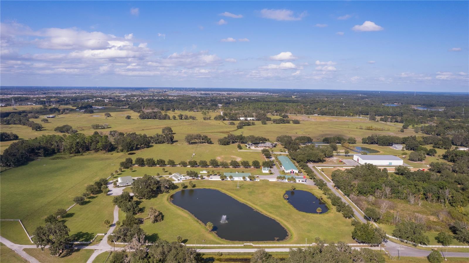 Introducing an Extraordinary 16+ Acre Estate Home: A harmonious blend of upscale living and serene country charm awaits you just a few miles from the vibrant cities of Leesburg, Mount Dora, Clermont, The Villages  and only an hour or so to both Orlando or Tampa. This exclusive property boasts over 30,000 square feet under roof, making it a rare gem in the real estate landscape.

As you enter through the gated and fenced property, you'll be greeted by large winding driveways leading around water features adorned with elegant fountains. The landscape evokes the grandeur of Southfork Ranch, reminiscent of the iconic television show "Dallas." The main home, spanning over 4400 square feet, offers climate-controlled living spaces and features over 2100 square feet of wrap-around porches and lanais.

Upon reaching the entrance, one is compelled to pause, sipping sweet tea or lemonade in rocking chairs while taking in the panoramic views of nature and wildlife. The main living room impresses with soaring ceilings, a floor-to-ceiling fireplace, and sliding glass doors that seamlessly bring in the beauty of the surrounding countryside.

This remarkable property is designed for both entertaining and practicality. The main home comprises 5 full bedrooms and 4 bathrooms, including a spacious 675+ square foot party room with a wrap-around bar. The detached 2000 square foot garage offers versatility, with a loft and space for an in-law suite, ranch hand apartment, or exercise room, complete with separate HVAC.

In addition to the main residence, a guest home spanning two stories and over 2000 square feet provides 3 bedrooms, 2 bathrooms, and 2 kitchens – ideal for long-term rental income or accommodating visiting friends and family.

The estate further includes several purpose-built structures, such as a 5160 square foot steel building (labeled show barn), a 1080 square foot tractor barn, and a substantial 12,500 square foot insulated steel building. For those with a penchant for automotive collections, there's ample space for storage in buildings equipped with bathrooms and large roll-up doors.

Whether you envision hosting events, embracing the tranquility of country living, or enjoying the expansive wildlife, this exclusive property offers a unique blend of elegance, peace, and your very own slice of paradise. Don't miss the opportunity to make this exceptional estate your home.