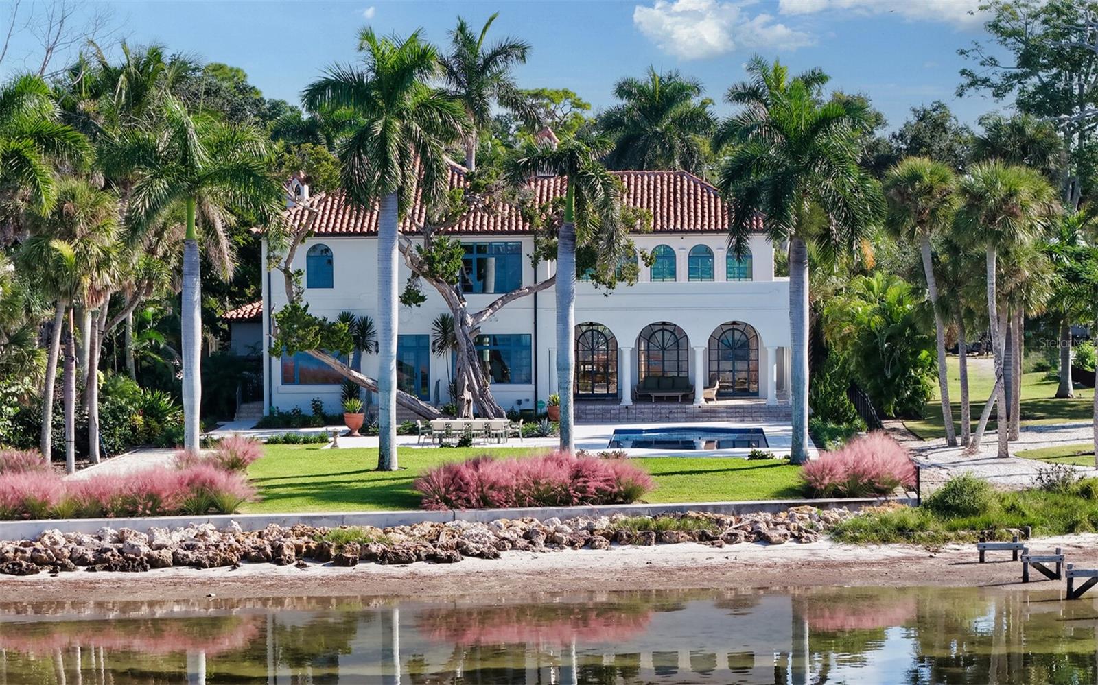 STUNNING BAYFRONT ESTATE at an incredible price.  Located in the Indian Beach–Sapphire Shores neighborhood, this 1925 Mediterranean estate sits on nearly three-quarters of an acre with sweeping views of Sarasota Bay—from the downtown skyline and Ringling Bridge to the northern tip of Longboat Key. Meticulously updated while maintaining its original character, the home blends historic craftsmanship with modern comfort. Behind the gated entry, a koi pond and circular drive with a central fountain lead to a welcoming courtyard featuring four garage spaces. The main living areas are defined by high ceilings, detailed millwork, and generous natural light. The formal living room features a coffered ceiling and marble fireplace, while the adjoining dining room offers bay views, custom built-ins, and a hand-painted recessed ceiling. The newly renovated kitchen includes a Sub-Zero refrigerator, AGA induction range, dolomite countertops, and breakfast area. The den/office overlooks the pool and bay, and the grand salon—with its soaring ceilings, stately fireplace, and 10-foot arched doors—opens to a large covered terrace ideal for entertaining or enjoying the spectacular sunsets. Upstairs are three ensuite bedrooms, each with access to a private terrace. The primary suite, fully redesigned in 2021, includes a spacious walk-in closet, and a luxurious bath with soaking tub, and walk-in shower. Landscape architect Michael Gilkey transformed the grounds into multiple outdoor spaces featuring a lush tropical garden, bocce court, tiled heated pool, and ample patio space. A separate guesthouse offers two rooms, 2 baths, and a kitchenette, easily configured as two ensuite bedrooms. Additional updates include new HVAC systems, air-conditioned garages, new seawall (2022), upgraded electrical and lighting, and impact-rated windows and doors. A rare blend of history, privacy, and waterfront elegance. Book your private showing today.