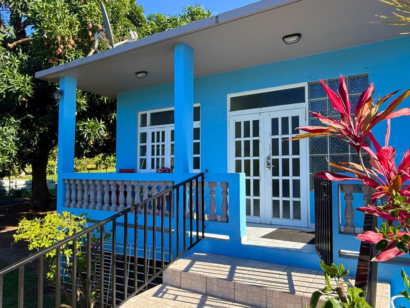 “Mango Paradise” is a titled 3BR/2BA concrete home located in the La PRRA neighborhood of Vieques Island, Puerto Rico. Situated on nearly ¼ acre, this fully fenced property offers tropical character, practical living spaces, and a convenient central-island location between Esperanza and Isabel Segunda.

The property features three mature fruit-bearing mango trees, gated driveway parking for two vehicles, covered front porch, rear patio/bar entertaining area, detached storage building, and former horse stable/corral area. The detached structure offers potential for office, studio, workshop, or guest casita use.

Interior layout includes a shotgun-style flow connecting the living room, dining room, and kitchen. Decorative arches and a wood countertop bar create separation between spaces while maintaining an open feel suitable for entertaining. White tile flooring runs throughout the home. The kitchen includes concrete countertops and shelving, farmhouse sink, dishwasher, oven, gas stove, and compact refrigerator. Laundry room adjacent to kitchen has space for washer, dryer, and additional refrigerator.

Primary bedroom includes ensuite bathroom with walk-in shower. Two additional bedrooms share a rear bathroom. Bedrooms are equipped with mini-split air conditioning units.

Covered rear patio includes outdoor sink suitable for gardening, beach gear rinsing, or entertaining. Front porch faces north and captures trade winds along with a slight ocean view.

Conveniently located near beaches, restaurants, ferry terminal, airport, wildlife refuge, and the world-famous Mosquito Bay BioBay. Suitable for full-time residence, vacation home, or investment property on Vieques Island.