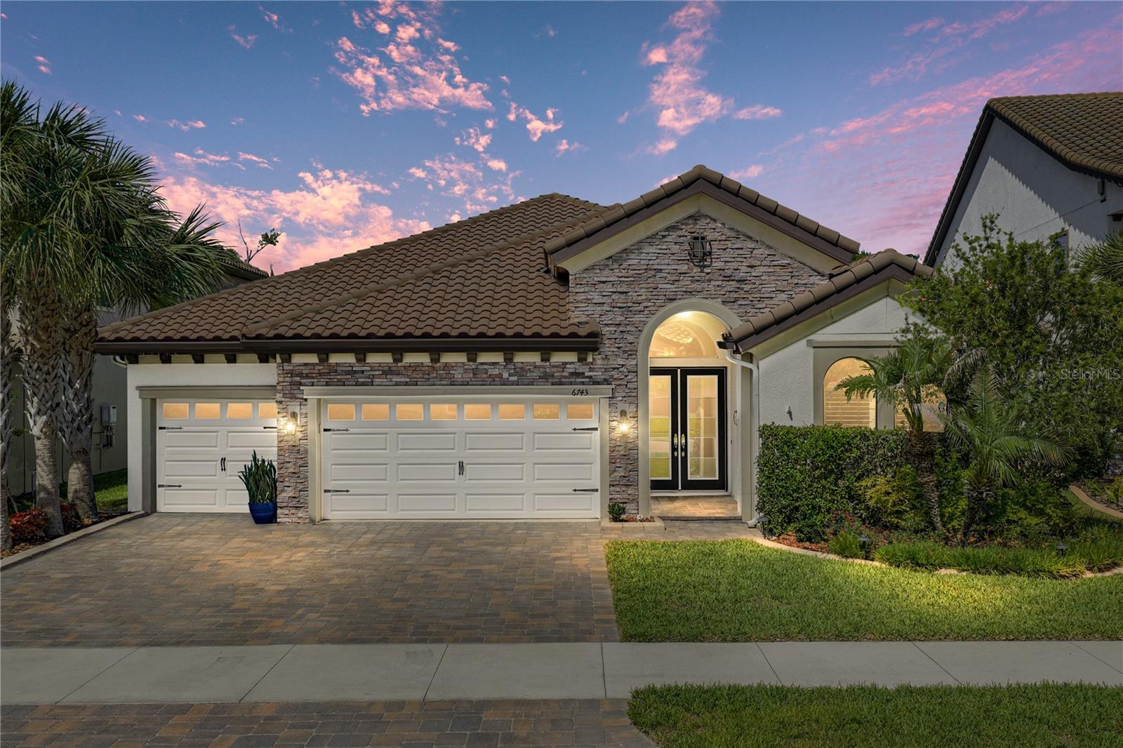 This is the kind of lakefront setting people imagine when they dream about Florida living. Sunset views stretch across the water from the backyard, a private dock waits just beyond the lawn, and every gathering has Curve Lake as the backdrop. Built in 2019 with 3 bedrooms + office, 3 baths, and a 3 car garage, this home brings together a polished interior, a resort worthy outdoor retreat, and a waterfront lifestyle made for boats, jet skis, quiet mornings, and evening entertaining. The arrival feels elegant with sidewalk lined streets, a paver driveway, stone accents, seasonal trim lighting, and lush St. Augustine grass for a manicured finish, with layered landscaping adding privacy, style, and care before you step inside. The open concept main living areas carry a refined, custom feel. Plank tile flooring flows through the space, high ceilings with wood look beams draw the eye upward, and a stone feature wall adds texture. Quadruple sliders pull in natural light and frame views toward the lake, while generous sightlines connect the kitchen, dining, and living room for effortless gatherings. Anchoring the space, the gourmet kitchen is stunning and well appointed with finishes that make the room easy to love and use. Granite countertops cover the large central island that drops down into an extended granite table, creating a memorable spot for meals and conversation. Stainless steel appliances, a gas cooktop, decorative backsplash, walk in pantry, desk nook, and beautiful light fixtures complete the chef’s kitchen. Through modern sliding barn doors, the office/bonus room offers a fluted sound reducing wall to quiet noise transfer, making it a perfect fit for remote work, movie nights, or music practice! The private primary suite has calming water views, back porch access, added insulation in the walls and door for sound control, an oversized walk in closet, and an ensuite with dual sinks, granite topped counters, vanity seating, a private water closet, and a massive walk in shower with bench seating. Bedrooms 2 and 3 are also separated, giving guests or additional occupants their own sense of seclusion. Positioned near the second and third full bathrooms, these rooms welcome overnight company. Beyond the sliders, the property becomes the kind of Florida retreat people try to recreate on vacation. A covered paver patio with retractable screens creates a shaded lounge off the main living area, while the outdoor kitchen and bar include a built in grill, sink, refrigerator, and bar seating. Across the fenced yard, a separate pergola offers a peaceful place to sit facing the water, enjoy a meal, or linger at sunset. The firepit area with cypress benches adds another gathering spot, and lush upgraded St. Augustine grass keeps the backyard soft, green, and usable. A Mosquito Mist system keeps the outdoor experience comfortable throughout the year. The dock deserves its own moment. A dedicated walkway leads to the $40,000 lakefront dock, complete with covered boat parking, electric, and water. This gives the property true lake life function, not just a pretty view. Bring the boat, jet skis, fishing gear, paddleboards, or a quiet chair at the edge of Curve Lake. Set within the gated community of Pristine Lake Preserve, residents enjoy a playground and park in a convenient Land O Lakes location close to schools, shopping, dining, entertainment, and major roadways for an easier commute. Call us today to experience this lakefront oasis for yourself!