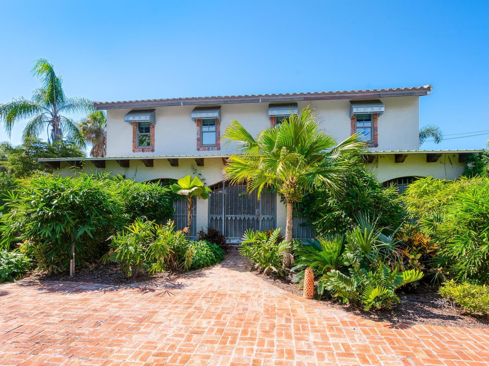 Virtually Staged. Hidden behind lush plantings is this beautifully redesigned and amazingly private two-story home boasting over 3900 sq ft of interior living space all moments away from the shops & cafes of St. Armands Circle, the beaches of Lido Key & downtown Sarasota. As you enter this hideaway of peace and tranquility you are greeted by a fountained courtyard garden through gates of aged iron. From there the interiors will call to the imagination as it evokes the visions of a bastide in Provence or a country home in the hills of Scotland. Imperfection is curated and intentional. Rooms flow easily enhanced by wide plank reclaimed wood floors, white ship lap walls framed with wood accents, reclaimed wood beams artfully placed throughout, thick roughhewn interior doors with patinaed hardware,  an eclectic kitchen design with soap stone counters, side tables and oven backsplash, a double farm sink, a new 10- burner dual fuel  gas range with two ovens, a Sub-Zero fridge with a glass door & four bottom draws to name just a few of the many appealing details.  A grand front room leads to a beautiful staircase of wood and clay tiles with a landing at the center of the house leading you to the primary suite, encompassing the entire second floor. Here we have a library/seating room lined with bookshelves, roughhewn wide plank wood floors, a spacious bedroom with a Julliet balcony, two walk-in closets and bath with a tub, large quartz shower with horizontal subway tiles, dual shower heads & handheld and two vanities with surface mount sinks and quartz counters sitting on retrofitted antique cabinets. There is a loggia spanning the width of the house opening on to an exceptionally large backyard bursting with lush tropical foliage. The nearly 12,000 sq ft lot is 160 ft deep. Intricately laid clay tiles form multiple walkways and an extensive lounging area. Beautifully weathered custom wrought iron gates abound not only on the drive entry but also on the courtyard and on the arched window openings of the loggia. Aged clay tiles surround windows and doors, even the garage door. Custom crafted metal awnings adorn the windows. Exterior custom metal lanterns and sconces echo the same intentional aging. There are two tankless water heaters, a whole house water purifier and a well for the yard. This home will captivate you.