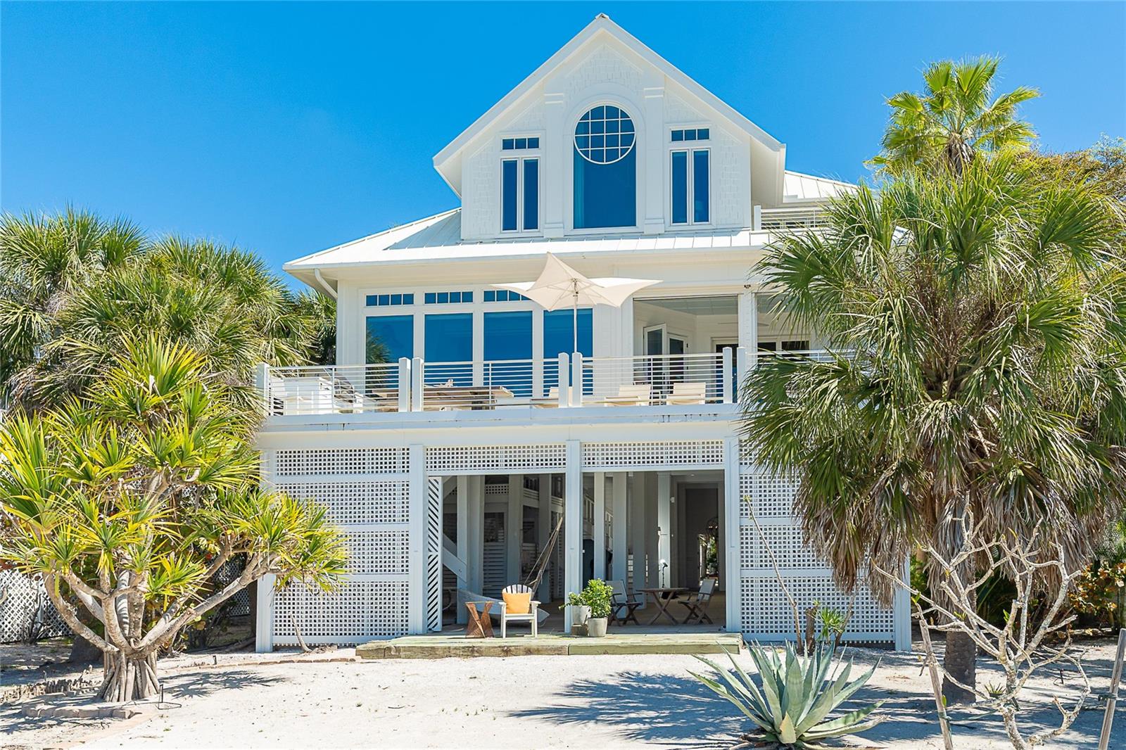 Unparalleled craftsmanship meets coastal elegance in this exceptional Gulf-front residence, ideally located within a premier island resort community on Palm Island, perfectly positioned between Sarasota and Ft. Myers. Accessible only by boat or car ferry, this exclusive barrier island offers over seven miles of pristine, uncrowded beaches and an “away from it all” lifestyle that is increasingly rare along Florida’s Gulf Coast. This property greets you with swaying palms and tropical foliage, then offers a stunning primary suite, two guest bedrooms, a private office/den, four full bathrooms, and one-half bath, this home is designed to capture Gulf views while delivering refined luxury and effortless coastal living. The open-concept kitchen, living, and dining areas are filled with natural light, highlighted by expansive full-length windows that frame endless water views and unforgettable sunsets. The chef’s kitchen is a showpiece, featuring a double Wolf gas range, integrated Sub-Zero refrigerator freezer, a large double island with custom zinc clad surfaces, crisper drawers, and a beverage cooler providing exceptional space for entertaining or preparing a gourmet meal. A butler’s pantry connects to the laundry room and includes a half bath and second dishwasher. A sleek wet bar is built into the kitchen, featuring a small sink, custom cabinetry, and a wine cooler. The adjoining living space is complimented by a gas fireplace. The dining area is elevated by a raised shiplap, cupola-style ceiling and surrounded by sliding windows overlooking the blue water. Anchoring it all is imported Jerusalem gray gold limestone tile. Open the doors to the upper porch and lower the motorized screens to create a shaded retreat. Here integrated hurricane shutters provide an added layer of protection. The lower sun deck spans the width of the home—soak up the sun or enjoy outdoor dining and cooking. The main-floor study offers custom built-in shelving and its own private balcony—perfect for a peaceful retreat. Built for both beauty and durability, the home showcases a full Hardie board exterior, a hidden 4-zone air conditioning system, and exceptional architectural detail throughout. The wide staircase with wrought iron railing is complemented by the convenience of a newer elevator servicing all levels. French doors open to the upper-level private primary suite with sweeping Gulf views and a dedicated sitting area. The spa-inspired primary bath features a walk-in shower with bench and multiple shower heads, marble tile and flooring, and an oversized jetted soaking tub with a Gulf view. The luxury continues with back-to-back vanities, walk-in closets, and a separate dressing space. Equally impressive, one guest suite features a queen-size bed and its own bathroom. The second bedroom includes built-in twin beds and additional freestanding beds to comfortably sleep multiple guests, along with a full bath. The ground level offers painted pilings, weather-treated wood plank flooring, and generous space for relaxing and entertaining. This level also accommodates a golf cart garage, tool storage, and built-in shelving. Situated within a sought-after resort community, including a community pool, fitness center, massage room, and tennis program. Ownership includes first right of refusal on a dock with lift—an opportunity for boating enthusiasts. This is a rare offering combining luxury design, resort-style amenities, and the serenity of Gulf-front living.