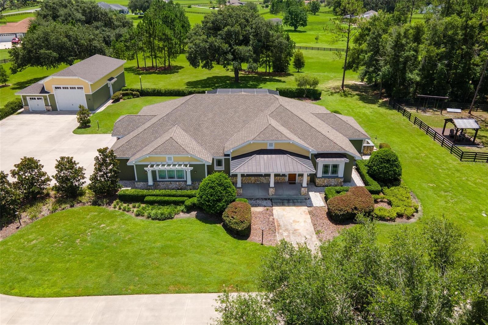 Stunning Sumter Crossing Estate! Welcome to this absolutely incredible custom-built estate in the gated community of Sumter Crossing, located in Oxford, Florida. Privately situated on 6.27 fully fenced acres, this true craftsman-style home showcases solid wood details and expert millwork throughout—offering timeless charm paired with high-end functionality. Designed for comfort, security, and versatility, the home includes an attached three-bay garage with an 11-foot high center door and a Back Yard Buddy 4-post car lift with a 7,000 lb. capacity for serious car enthusiasts or collectors. In addition, a pristine detached RV garage offers two bays, including one with a 14’x16’ overhead door—ideal for RVs, boats, or workshop use. All garage spaces are climate-controlled with mini-split A/C systems, and the RV garage includes its own full bath for added convenience. Built to exceptional standards, this home features hurricane-rated, shatter-resistant windows, solid core and fire-rated interior doors, spray foam insulation, a generator for peace of mind during storms. Inside, you'll find stunning ceilings with wood accents, crown molding, tall baseboards, and meticulous wood-trim details throughout. The thoughtfully designed kitchen is the heart of the home, boasting GE Monogram appliances, an induction cooktop, farmhouse sink, expansive countertops, a center island with vegetable sink, a breakfast bar, custom cabinetry with built-in cookbook shelving, and a fully built-out walk-in pantry. It opens beautifully into the grand living room, where custom built-ins and elegant wood ceilings create a warm and inviting atmosphere. A formal dining area and a spacious Florida room—surrounded by windows and filled with natural light—complete the main living space and provide the perfect place for gatherings. The luxurious primary suite is a private retreat with two custom walk-in closets featuring built-in shelving, drawers, and a secure safe. The en-suite bath includes dual sinks, a separate makeup vanity, a large walk-in shower, a water closet, and built-in shelving. In addition, the master closet was designed as a tornado-safe room, built to withstand high winds for added safety. Outside, enjoy the screen-enclosed pool and spacious lanai, complete with a summer kitchen sink—perfect for entertaining. The circular driveway provides ample guest parking, and the fenced backyard includes a separate fenced area for pets or play, with a charming gazebo for shade. Additional features include a spacious laundry room with ample storage, a whole-home audio closet for media and tech systems, dimmer switches on all lighting, a top-tier security system, engineered hardwood flooring, and board and batten siding with stone accents that complete the estate's craftsman curb appeal. This is more than a home—it's a private, well-crafted retreat where quality and comfort shine through every detail.