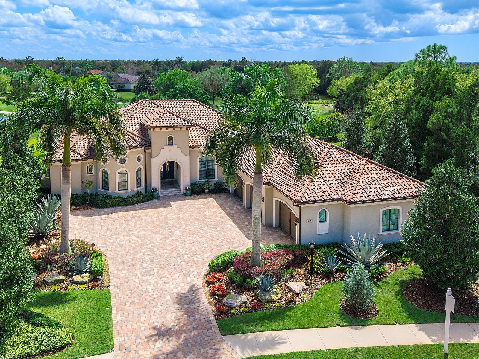 Set within Country Club East, on Royal Lakes' 16th fairway, this highly customized, green-certified residence is distinguished by its architectural details and elevated finishes. Mature landscaping frames the home, complemented by lighting, an expansive side yard, and a paver driveway. Inside, a striking entry with tongue-and-groove ceiling detail and arched iron double doors opens to a cathedral-ceiling foyer, where architectural archways guide the transition into the main living spaces. Throughout the home, upgrades such as solid wood arched doors, crown molding, 7-inch baseboards, Icynene spray foam insulation, and a blend of stone flooring with Dura Shield coating and engineered wood create both visual continuity and performance-driven comfort. The great room is designed with soaring 14-foot ceilings accented by faux wood beams and a recessed media wall with stacked stone detailing. Sliding glass doors open fully to the lanai, drawing in natural light and framing unobstructed views of the pool, lake, and golf course beyond. The kitchen and dining areas strike a balance between functionality and style. Custom cabinetry with glass-front uppers and integrated LED lighting pairs with a full suite of Sub-Zero and Wolf appliances, including a wine cooler and additional refrigeration. A vast floating island with hidden outlets and storage anchors the space, while a walk-in pantry with wood shelving and thoughtful details, such as spice pull-outs and concealed trash storage, enhances everyday usability. Adjacent dining spaces are elevated by layered ceiling treatments, designer lighting, and zero-corner sliders that emphasize the indoor-outdoor lifestyle. A detailed office offers dual workstations, extensive built-ins, a circular tray ceiling with intricate woodwork, and shiplap accent detailing. The primary suite is privately positioned, featuring tray ceilings with cove lighting, a sitting area, lanai access, and dual custom walk-in closets. The spa-like bath includes a Kohler soaking tub with stone surround, two vanities, and a walk-in shower with multiple showerheads, travertine finishes, and architectural window detailing. Three guest suites are equally refined, offering spacious closets, plantation shutters, and access to well-appointed bathrooms featuring custom tilework, granite surfaces, and a shower and/or tub. A standout bonus space, currently configured as a golf simulator room, features a barrel-vaulted ceiling, professional-grade flooring, and direct lanai access. The outdoor living experience is designed as a private resort setting. The lanai features a tongue-and-groove ceiling, recessed lighting, and multiple seating areas overlooking a saltwater pool and spa, complete with iridescent tile and a sun shelf. A fully equipped outdoor kitchen boasts Monogram appliances, marine-grade cabinetry, and granite countertops, all set against tranquil views of the golf course and water. Functionality is further enhanced by a well-equipped laundry room, a thoughtfully designed drop zone and mudroom entry from the garage, and extensive storage throughout. The oversized garage, which holds 6 cars, is equipped with epoxy flooring, built-in cabinetry, overhead storage, a utility sink, and a 7,000lb car lift. Ideally located in Lakewood Ranch, residents are just minutes from Waterside Place, UTC shopping and dining, Nathan Benderson Park, SRQ Airport, downtown Sarasota, and the renowned Gulf beaches.