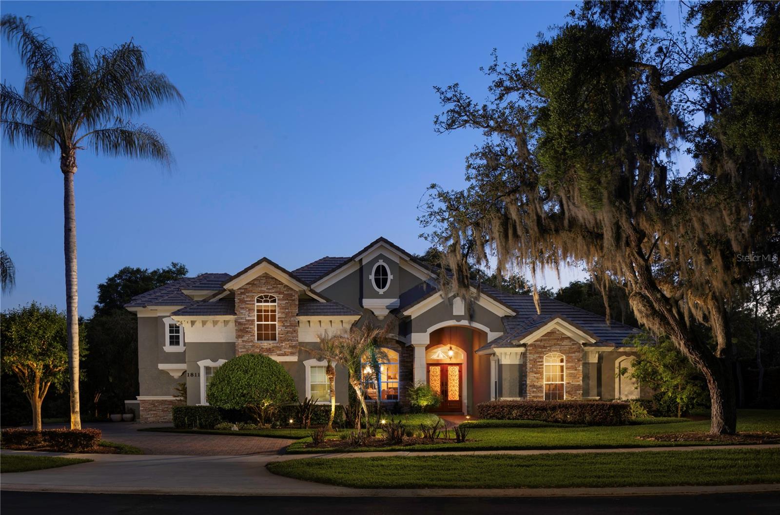 Welcome to Carisbrooke, an exclusive gated enclave of just 43 estates set on sprawling one-acre homesites within the sought-after Markham Woods Corridor. Surrounded by scenic walking trails, community parks and the refined charm of the Lake Mary lifestyle, this exceptional location offers effortless access to major interstates and beltways, placing world-class attractions, pristine beaches and top-tier regional hospitals all within easy reach. From the moment of arrival, a beautifully maintained landscape, fresh designer exterior paint and an elegant circular drive create a striking first impression, leading to grand custom double entry doors. Inside, a dramatic introduction unfolds as floor-to-ceiling windows to frame serene views of the lanai and resort-style pool, while rich travertine flooring and intricate applied moldings elevate the home’s architectural presence. The interior has been lavishly reimagined with uncompromising attention to detail. The chef’s kitchen is a showpiece, appointed with Sub-Zero and Thermador appliances, bespoke cabinetry and exotic granite surfaces. Distinctive design elements, including an Invisacook cooktop and a Waterstone copper faucet set above an impressive 42-inch sink, create both visual intrigue and functional excellence. The adjoining family room, anchored by a custom-built entertainment center, flows seamlessly to the outdoor living spaces. The primary suite is a private retreat, offering rich hardwood flooring and a beautifully renovated spa-inspired bath designed for relaxation and indulgence. The private office enjoys a built-in closet with the versatility of a possible fifth bedroom if desired. Two additional bedrooms are thoughtfully positioned on the main level and share a jack-and-jill bath, while the fourth bedroom and a generously sized bonus room upstairs provide exceptional flexibility for lifestyle, entertainment or leisure. Outdoors, the experience continues with a newly installed limestone paver pool deck overlooking an expansive, meticulously manicured backyard. A striking 10-foot granite fire pit and a custom pergola set the stage for unforgettable evenings under the stars. Completing the residence is an oversized three-car garage with extended driveway parking, along with new mechanical systems, updated designer fixtures and whole-house audio, delivering a turnkey, move-in-ready estate defined by luxury, comfort and incredible Florida lifestyle.