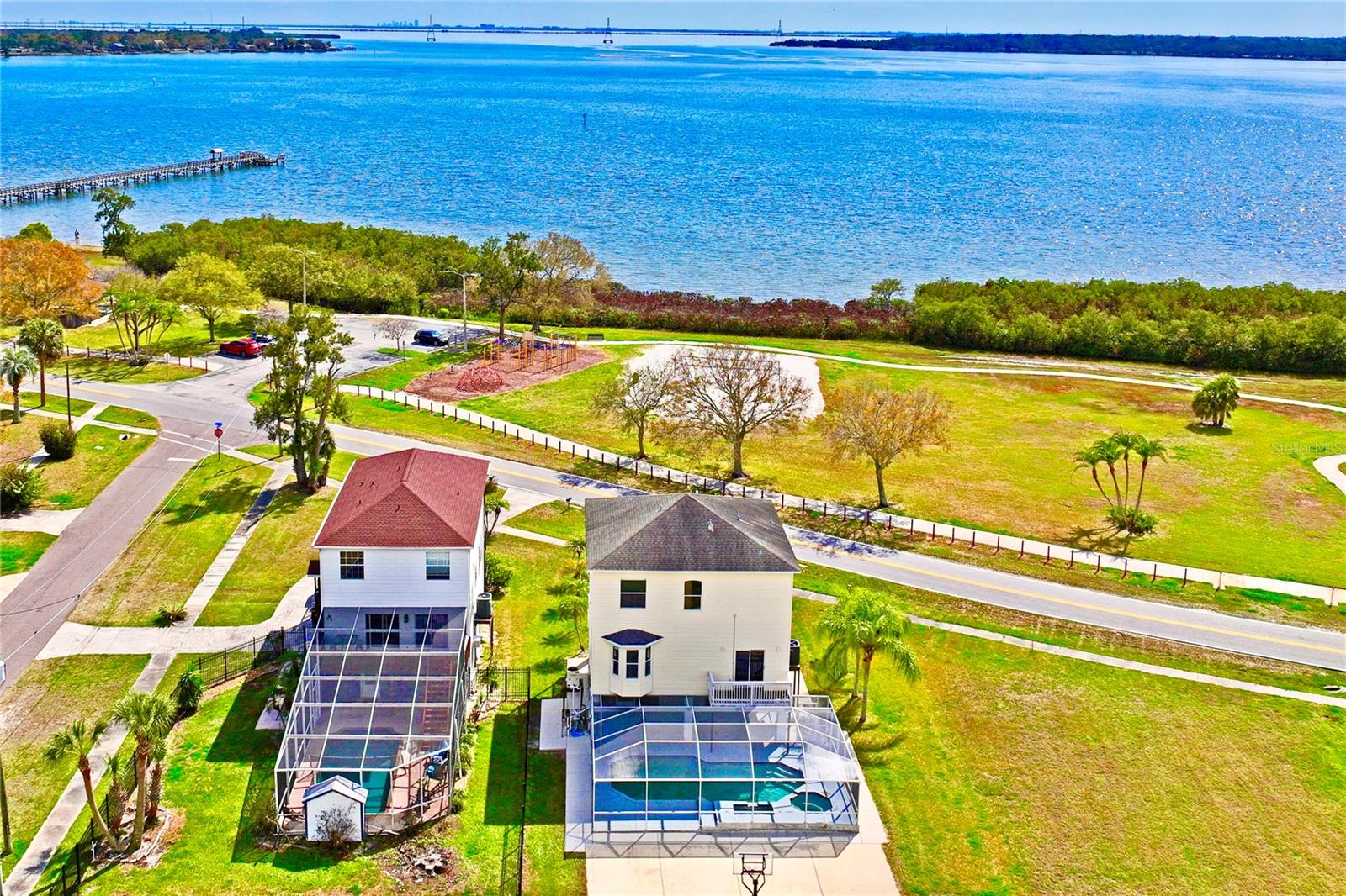 One or more photo(s) has been virtually staged. Gorgeous water views of Old Tampa Bay from this custom-built, original-owner home in a prime Oldsmar location, directly across from popular R.E. Olds Park with its amphitheater, fishing pier, playgrounds, sand volleyball and annual fireworks you can enjoy from your front porch. The resort-style backyard features a large inground pool with spa, kiddie pool, spillover fountain and fiberoptic lighting, all within a screened enclosure with covered area for dining and parties. A spacious concrete pad doubles as a basketball court and offers room to store a boat or add a shed, plus parking for 2 cars under carports and a deep driveway that has accommodated 10+ vehicles, with overflow available at the park. Upstairs, the main living level welcomes you through double hurricane-rated doors to beautiful Brazilian hand-scraped wood floors, abundant windows, and an eat-in kitchen with granite counters and arched opening to the living room, along with a formal dining room. An office or bedroom on this level opens via sliding glass doors to a balcony overlooking the pool, and a convenient half bath completes the floor. The bedroom level begins with a newer washer/dryer closet for easy access to all bedrooms. The primary suite offers stunning water views from sliders, the third-level deck and multiple windows, and its ensuite bath was updated in 2017 with new cabinetry, tile and quartz counters; the second full bath was also updated. Major updates include a 2016 roof and 2023 A/C, making this well-maintained home ideal for both everyday living and large gatherings.