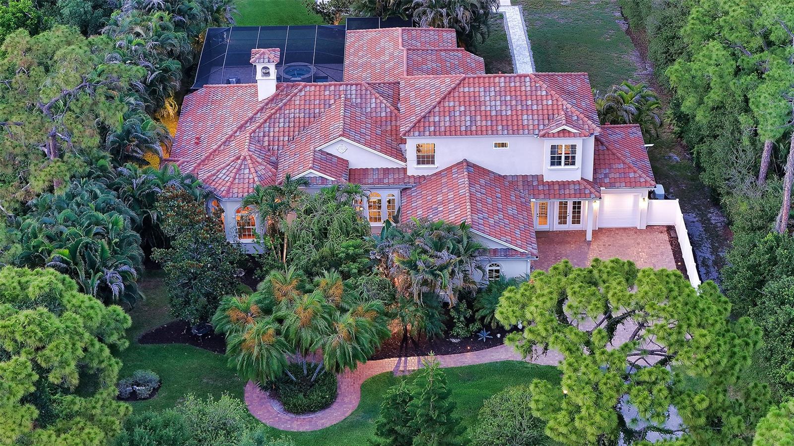 Crafted by renowned luxury builder Todd Johnston, this legacy estate offers over 4,000 sq/ft of thoughtfully designed living space on two private acres within the sought-after community of Foxfire West. Framed by mature tropical landscaping and tranquil lake views, the property offers a timeless blend of elegant architecture, privacy, and resort-style living. A long, winding driveway welcomes you to the residence, where nearly every room enjoys picturesque views of the surrounding grounds. Designed for both everyday living and effortless entertaining, the home's open floor plan is centered around an expansive chef's kitchen- the true heart of the home. Featuring new Wolf and Sub-Zero appliances (2025), solid wood cabinetry, stone countertops and backsplash, a large center island with abundant storage, vaulted ceilings, and seamless connectivity to the surrounding living and dining spaces, the kitchen serves as the natural gathering place for family and friends. A truly exceptional feature rarely found in today's market is the home's private guest residence. Complete with its own living room, kitchenette, private bedroom and bath, attached one-car garage, and covered lanai, it functions as a true second living quarters- ideal for multigenerational living, extended guests, a live-in caregiver, or long-term visitors without sacrificing privacy for either host or guest. One of the home's most distinctive design elements is its seamless connection to the outdoors. The principal living spaces (great room, kitchen, primary suite, and flexible bonus room) all open directly to the screened lanai, allowing the home to wrap gracefully around the heated pool and spa. Complete with an outdoor kitchen and multiple areas for dining, relaxing, and entertaining, the lanai becomes a true extension of the home's interior, embracing Florida's year-round lifestyle. Rich architectural details, including arched windows, travertine flooring, soaring ceilings, and a wood-burning fireplace, create warmth and character throughout the main living areas. Beyond its architectural beauty, the home has been meticulously maintained with significant recent mechanical upgrades, including newer HVAC systems (2024) and a whole-home generator with a propane tank (2023), providing comfort, efficiency, and peace of mind for years to come. The first-floor primary suite offers a tranquil retreat with dual walk-in closets and direct access to the lanai. A handsome library or study offers the perfect work-from-home space, while the oversized flex room with a built-in Murphy bed provides endless possibilities as a media room, fitness studio, or additional guest accommodations. Upstairs, two generously sized bedrooms, each with its own walk-in closet, are connected by a thoughtfully designed Jack-and-Jill bath featuring two private vanity areas joined by a shared shower and water closet, offering both privacy and functionality. A spacious loft and oversized terrace create an inviting secondary gathering space overlooking the beautifully landscaped property. Beyond the heated pool and spa, the estate grounds feature a private pickleball/sports court, batting cage, expansive lawn, and multiple destinations for entertaining, recreation, or quiet relaxation. Combining timeless craftsmanship, an exceptionally versatile floor plan, recent system upgrades, and an extraordinary setting, this is a rare opportunity to own one of Foxfire West's most distinctive legacy estates.