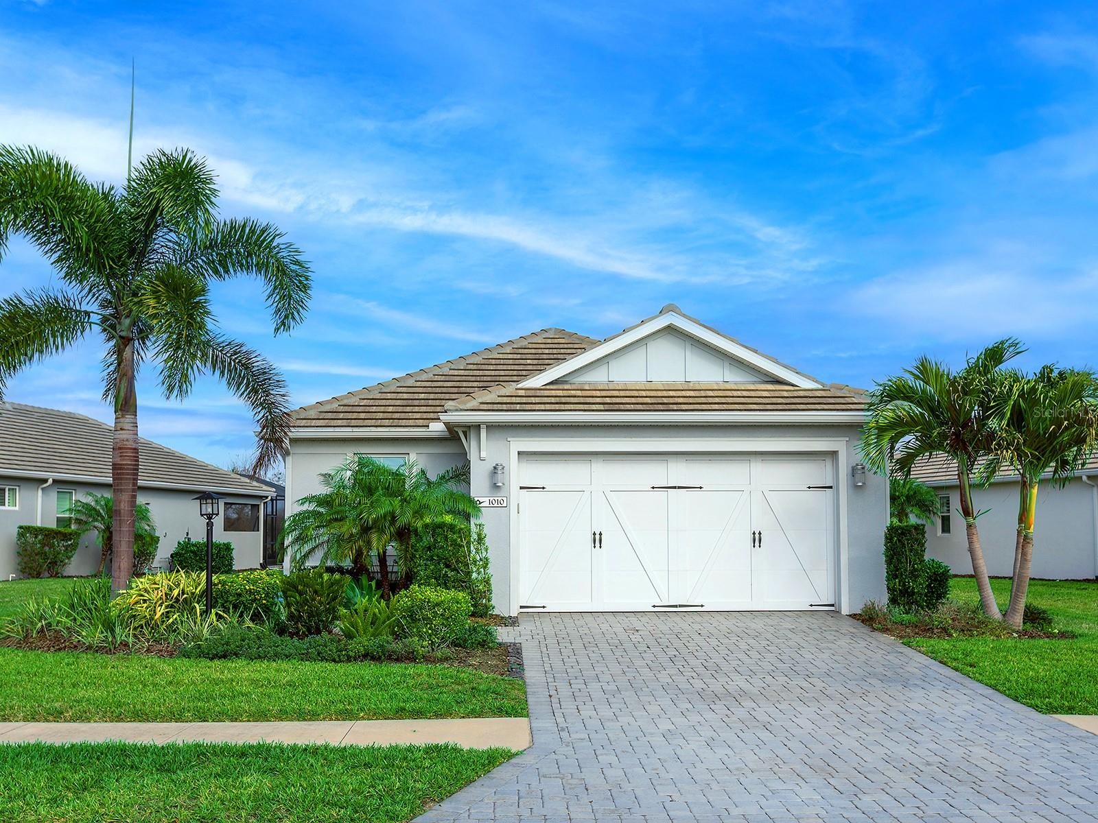 Step inside and discover a residence that effortlessly blends refined comfort with the relaxed elegance of Florida living. 1010 Crosswind, located within Lakehouse Cove at Waterside, offers 2,153 square feet of living space, including three bedrooms, two full bathrooms, and a versatile flex room, complemented by a coastal-inspired front elevation, paver driveway, and a two-car garage with carriage-style doors. Notable enhancements include hurricane impact windows throughout, a whole-house generator, crown molding, window tinting, upgraded light fixtures, recently painted interior walls, a tankless water heater, a water softener, and a reverse osmosis system. The kitchen is bright and contemporary, featuring white shaker cabinetry with crown molding, quartz countertops, a large center island with shiplap detailing and bar seating, stainless steel appliances, a classic subway tile backsplash, and three glass pendant lights that add warmth and style above the workspace. The dining area is defined by a distinctive brick accent wall, statement chandelier, plantation-shuttered window, and seamless connection to the surrounding living spaces. The great room features a tray ceiling with crown molding, a contemporary ceiling fan, abundant natural light, and large sliding glass doors that open to the screened lanai. The primary suite offers a spacious layout with preserve and pool views, tray ceiling with crown molding, ceiling fan, brand-new carpeting, and a custom walk-in closet with built-in organization. The ensuite bath is finished with a dual-sink quartz vanity, oversized walk-in shower with frameless glass, open shelving, modern lighting, and tile flooring. Two guest bedrooms are positioned at the front of the home and include crown molding, ceiling fans, plantation shutters, and plush carpeting, while the shared guest bath features a quartz vanity, a walk-in shower with frameless glass, modern fixtures, display shelving, natural light, and tile flooring. Outdoor living amazes with a paver lanai featuring covered seating with a ceiling fan, a heated saltwater pool with a sun shelf, a motorized retractable awning, and lush tropical landscaping set against private preserve views. The two-car garage is equipped with ceiling-mounted storage racks. Ideally positioned, the home offers convenient access to Waterside Place, Lakewood Ranch Main Street, the UTC corridor, and the new Mote Science Education Aquarium, while Sarasota’s renowned Gulf beaches remain just a short drive away. Life in Lakehouse Cove extends well beyond the residence itself, offering a thoughtfully designed lifestyle centered around recreation and connection. Residents enjoy six pickleball courts, a resort-style pool and spa overlooking Lake Kingfisher, a state-of-the-art fitness center, a boathouse with a kayak launch, two dog parks, a community clubhouse, and a fire pit gathering space. A short stroll leads directly to Waterside Place, where shopping, dining, a weekly farmers market, and year-round community events create a vibrant and highly walkable setting.