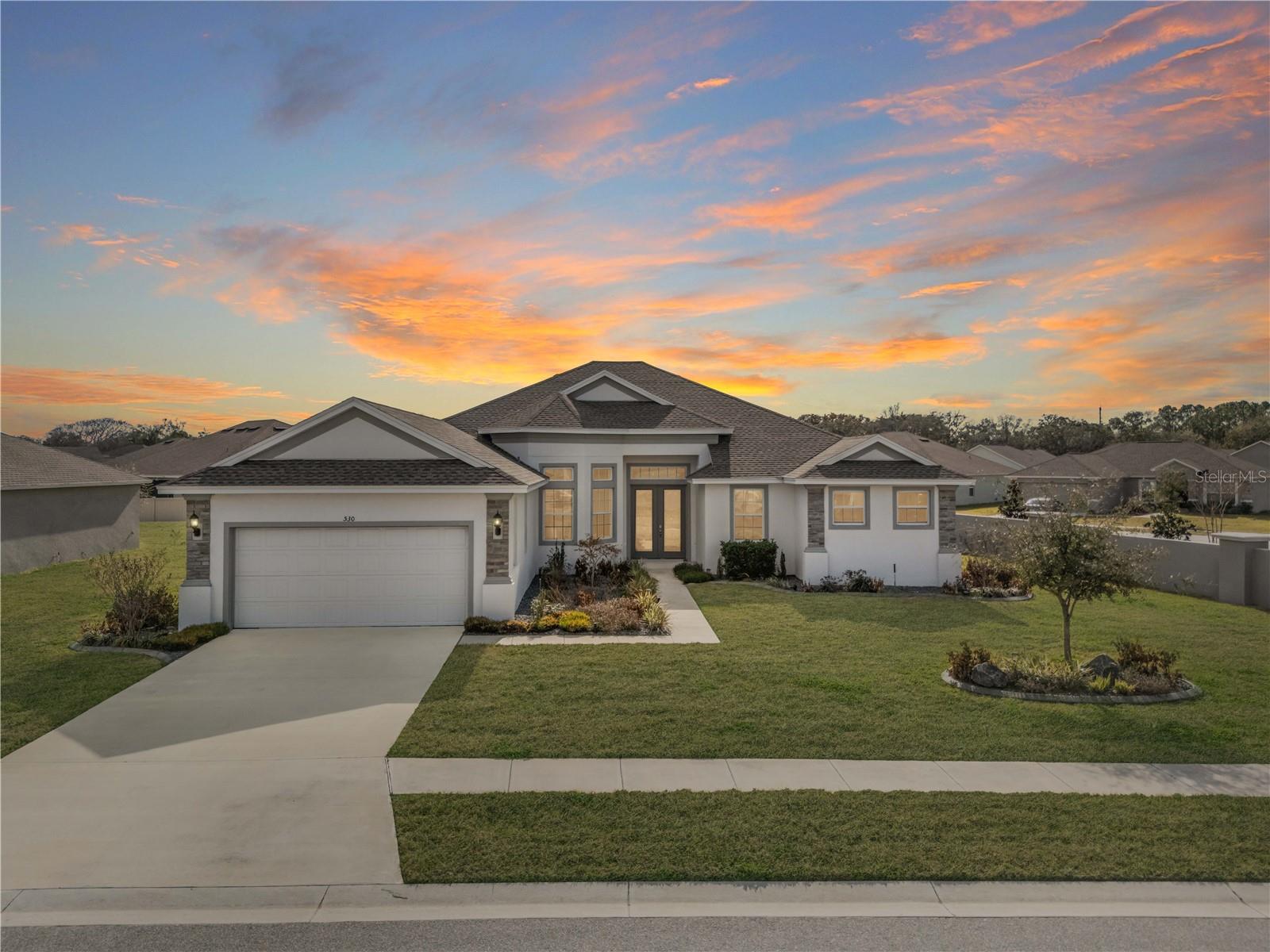 Welcome to this exceptional custom-built 2023 luxury residence located within the gated community of Sanctuary by the Lake, where modern elegance, thoughtful design, & everyday comfort come together seamlessly. Perfectly positioned on a spacious corner lot directly across from the lake, this stunning home immediately impresses with its commanding presence & refined architectural detail.
Step through the beautiful double front doors & experience an immediate sense of openness, highlighted by soaring ceilings, abundant natural light, & expansive living spaces designed to feel both grand & inviting. With over 3,600 square feet of living space, the thoughtfully designed open layout effortlessly connects formal & casual living areas, creating an ideal setting for both entertaining & relaxed daily living.
At the heart of the home lies a beautifully appointed chef’s kitchen, featuring granite countertops, upgraded Stainless Steel appliances, a breakfast bar, walk-in pantry, and generous prep space, perfect for hosting gatherings or enjoying quiet mornings at home. The kitchen flows naturally into the impressive great room and dining areas, enhancing the home’s seamless indoor living experience.
One of the standout features is the oversized covered and enclosed Florida room, custom added by the owners to extend the living space year-round. Whether hosting celebrations, entertaining guests, or simply unwinding while enjoying peaceful surroundings, this space truly elevates the lifestyle this home offers.
Designed with privacy in mind, the desirable triple split floor plan includes 4 spacious bedrooms, 3 full bathrooms, and a dedicated private office, ideal for remote work or flexible living needs. The luxurious primary suite serves as a private retreat, complete with dual vanities, a garden tub, separate walk-in shower, makeup vanity, and a very generous walk-in closet.
Beautiful luxury vinyl plank flooring flows throughout the main living areas, complemented by tasteful finishes and quality craftsmanship that reflect the home’s custom construction. A well-equipped laundry room with cabinetry, countertop workspace, and sink adds everyday convenience. A 50 amp generator port was added for peace of mind.
Beyond the home itself, the location offers the best of Central Florida living. Just minutes from downtown Winter Haven, residents enjoy award-winning restaurants, local boutiques, parks, and year-round entertainment, while nearby access to Lakeland & I-4 provides an easy commute to both Tampa and Orlando. Florida’s Atlantic and Gulf beaches are approximately 90 minutes away, making weekend coastal escapes effortlessly accessible. This is more than a home, it is a refined living experience combining space, luxury, and lifestyle within one of Winter Haven’s most desirable gated communities.