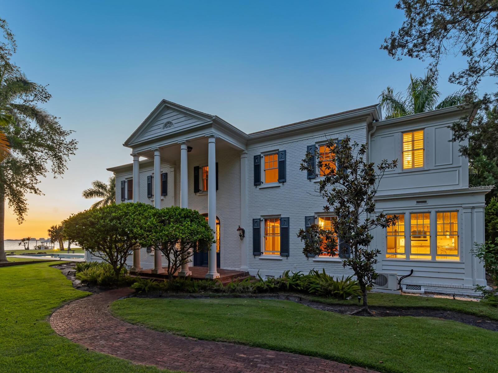 This storied waterfront estate occupies a 1.24-acre lot within the largest contiguous parcel on the Gulf Coast, a magnificent private park with a majestic landscape and vistas on par with Selby Gardens and the grounds of the nearby Ringling Museum. Renowned for its historical significance and stately Southern Colonial architecture, the Earle House presents a rare restoration opportunity to customize modern luxury with the provenance and style of old-world elegance. Encompassing both a two-story primary home and separate garage and guest house, the estate offers spacious accommodations for enjoyment as a seasonal retreat or year-round residence. Priced with consideration for renovations, this property is both comfortably livable and poised for thorough personalization. 
Distinguished by a double-height colonnade and beautiful brick exterior, the 4-bedroom, 4.5-bathroom home boasts original classical features throughout, including wood paneling and crown moulding, hardwood floors, fluted balusters, gas fireplaces, large chandeliers, stained glass transom, double-hung windows, and French doors. Built in 1927 and renovated to modern standards in the 90s with additional projects in following years, the home’s upgrades include a waterfront saltwater pool, elevator, walk-in showers, and top-line appliances.
Flanked by leaded glass window panels, the south-facing main entry opens to a grand foyer that leads on one side to the dining room and on the other to the waterfront great room and adjoining solarium. Awash in natural light from both south- and north-facing windows, the great room is anchored by a large central fireplace with granite hearth and an ornately carved mantle, with access at one end to a private wood-clad den with powder bath. Subtly partitioned from the great room by a coffered beam, the adjacent solarium seamlessly extends the main living space and spectacular vistas with a surround of oversized windows and double doors that open to the pool terrace and waterfront lawn. On the east side of the main floor, the foyer opens to the spacious dining room with two original arched door corner cupboards and a well-appointed wet bar that adds ample storage as well as additional under-counter refrigeration and dedicated beverage cooler. Beyond the dining room, a breakfast nook opens to the roomy kitchen.
Upstairs, a spacious landing leads to three large bedrooms, each with incredible views. To the right, a private alcove with elevator access leads to the western-facing primary suite with a massive brightly lit bedroom, walk-in closet with custom built-in wardrobe system, and a marble-clad bathroom with oversized vanity and walk-in shower. On the other side of the landing, two additional bedrooms offer generous layouts.
The history of the Earle House is integral to Sarasota’s early 20th-century development, dating to the formation of the Indian Beach community with the sale of magnificent waterfront homes to affluent families from across the United States. This remarkable estate, enviably near the Ringling Museum and Asolo Theatre, stands on an indescribable piece of land with more than 130 feet of private waterfront, winding paths, and a palm grove complementing the lush tropical landscape. With adjacent parcels available by separate offer, this is an opportunity to acquire the largest acreage on the Gulf Coast, rich in architectural history and unmatched in natural beauty.