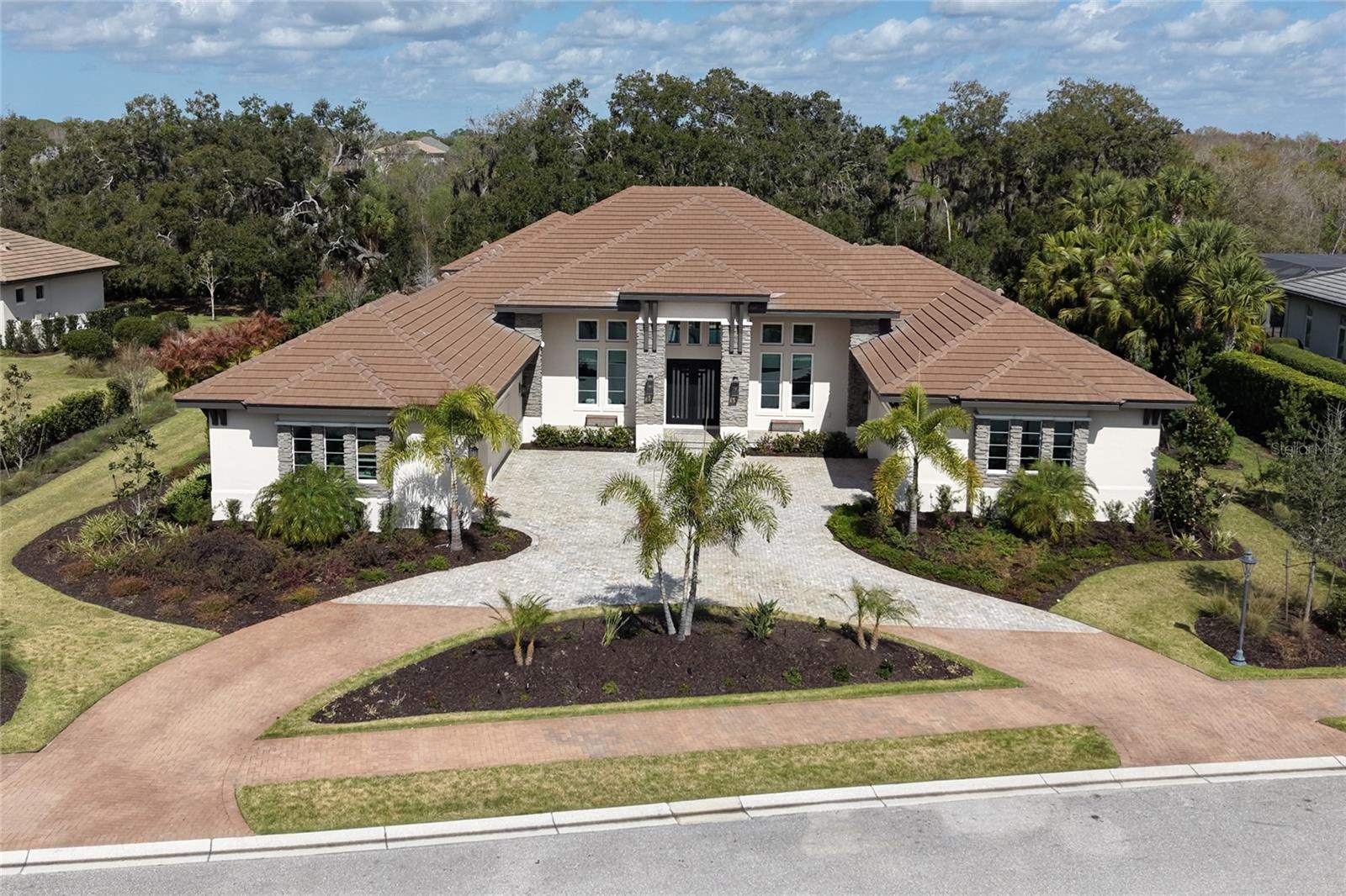 RARE 5-CAR GARAGE IN THE FOUNDERS CLUB.This newly constructed custom home is a true masterpiece. Perfectly positioned on a private estate lot of over half an acre, this exceptional residence offers 4,862 square feet of meticulously designed living space, framed by majestic 100-year-old oak trees and tranquil lake views. Designed with warm West Indies architectural influences, the home’s soft stacked stone façade and inviting front porch create a welcoming first impression. Iron and glass entry doors open to a dramatic Great Room highlighted by stained open truss beams, vaulted ceilings, a gas fireplace, and expansive 10-foot sliding glass doors that seamlessly connect indoor and outdoor living. Neutral wood flooring enhances the home’s refined yet relaxed ambiance.The thoughtfully designed layout includes three spacious bedrooms and four-and-a-half bathrooms, along with a private den that can easily serve as a fourth bedroom. Additional living spaces include a formal dining room with a striking tray ceiling featuring rich wood planks and exposed beams, a lounge/office with a custom sophisticated wet bar designed as both a statement feature and intimate gathering space.The breakfast kitchen is both beautiful and functional, featuring custom built-ins, an oversized island with seating, and a picture window overlooking the Chef’s Kitchen. Designed for culinary enthusiasts, the Chef’s Kitchen is equipped with a professional-grade gas range, wall ovens, paneled refrigerator, elegant quartz countertops, a generous walk-in pantry, and abundant natural light from skylights and large windows.The primary suite is a private sanctuary with separate his-and-her full bath retreats, each complemented by fully outfitted walk-in closets. A cozy sitting area offers a serene space to unwind while enjoying views of the oak hammock beyond.The bonus room’s disappearing glass corner doors open to a beautifully appointed outdoor living area featuring a summer kitchen with professional grill, dual cooling drawers, dedicated ice maker, and luxury finishes throughout. The resort-style pool with infinity-edge spa is protected by a clear-view screen, offering peaceful views of the lake and mature oaks. Built with exceptional quality and attention to detail, this residence includes a whole-house generator, foam insulation, impact-resistant Low-E windows and doors, and integrated Sonos audio. Furniture is available for purchase on separate bill of sale. The Founders Club offers an unparalleled lifestyle surrounded by 700 acres of natural Florida beauty. With just 262 homesites, this low-density enclave is designed for privacy and serenity. Residents enjoy access to a recreation center offering yoga and pilates classes, as well as Har-Tru tennis courts, pickleball, basketball, sand volleyball, and a kid's playground. Membership at the Founders Golf Club is optional offering both golf and social memberships. The renowned Robert Trent Jones Jr. golf course offers members easy tee times and is one of the only walkable courses in the region. Members enjoy a a grand Southern-style clubhouse, fine dining, a year-round social calendar, and a 24/7 fitness facility. It’s more than a home, it’s a lifestyle curated for those who appreciate understated luxury and quiet prestige. All just minutes from exquisite dining, shopping, and the vibrant art scene of downtown Sarasota, as well as Sarasota's incredible beaches.