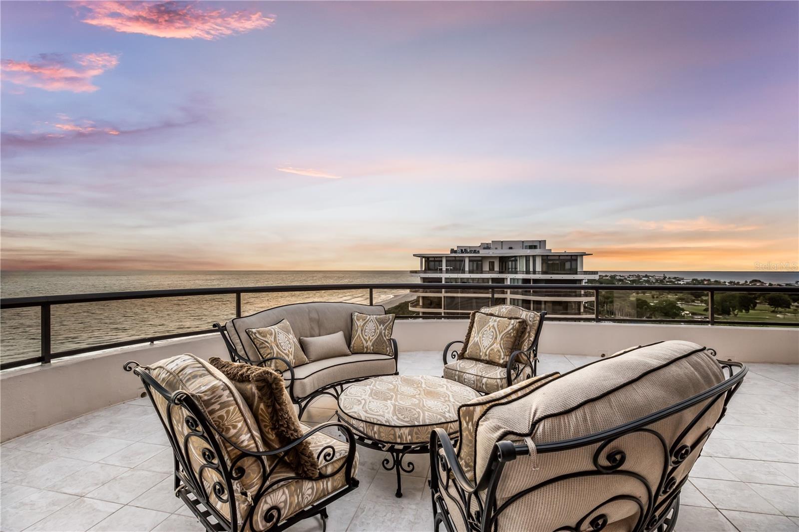 Perched atop the coveted South Building at L’Ambiance behind the gates of the Longboat Key Club, this extraordinary beach-to-bay penthouse redefines luxury coastal living. Encompassing nearly 5,000 square feet of refined interior space and complemented by more than 3,600 square feet of wraparound terraces, this rare residence offers the scale and privacy of a waterfront estate paired with the convenience and security of one of Longboat Key’s most prestigious condominium communities. From sunrise over Sarasota Bay to spectacular sunsets melting into the Gulf of Mexico, panoramic water views create a breathtaking backdrop from nearly every room. Arrive via a private elevator that opens directly into your own grand foyer, where ornate wrought-iron double doors reveal a residence defined by architectural elegance and meticulous craftsmanship. Cathedral coffered ceilings, intricate millwork, crown molding, custom built-ins, designer lighting, and expansive walls of newer impact glass create a dramatic yet inviting atmosphere throughout. Travertine flooring flows seamlessly from room to room, while floor-to-ceiling glass sliders open to expansive terraces, blending indoor and outdoor living on an unprecedented scale. At the heart of the residence, the impressive 34-by-41-foot living room is framed by Gulf views and surrounded by multiple entertaining spaces, including formal and informal dining areas designed for both intimate gatherings and grand-scale events. The gourmet chef’s kitchen is beautifully appointed with custom designer cabinetry, stone countertops, decorative appliance panels, a Wolf induction cooktop, oversized island, walk-in pantry, and generous workspace for effortless entertaining. Occupying its own private wing, the primary suite is a sanctuary. A private vestibule leads to a spacious lounge area, dual walk-in closets, and spa-inspired his-and-her bathrooms featuring custom vanities, stone finishes, soaking tub, separate shower, and abundant storage. Floor-to-ceiling glass opens directly to the terrace, where sweeping Gulf views create an ever-changing panorama. Two additional guest suites offer en-suite baths and walk-in closets, while a fourth bedroom—currently configured as a charming bunkroom—provides flexibility for family and guests. A spacious study can easily serve as a fifth sleeping area or executive home office. The outdoor living experience is simply unmatched. Expansive terraces wrap around the residence, creating multiple venues for dining, entertaining, and relaxation while capturing unobstructed views stretching from the Gulf shoreline across Sarasota Bay, the Longboat Key Club golf courses, and the downtown Sarasota skyline. L’Ambiance is widely regarded as one of Longboat Key’s premier beachfront addresses, offering residents exceptional amenities including 24-hour gated security, concierge services, on-site management, a recently renovated lobby and clubhouse, social rooms, fitness center, tennis courts, resort-style heated swimming pool and spa, private beach access, and a picturesque boardwalk leading directly to the Gulf of Mexico. Ideally positioned within the Longboat Key Club community, residents enjoy proximity to championship golf, tennis, marina facilities, waterfront dining, and miles of pristine Gulf beaches. This remarkable penthouse represents a rare opportunity to own one of the largest and most impressive beachfront residences on Florida’s Gulf Coast.
