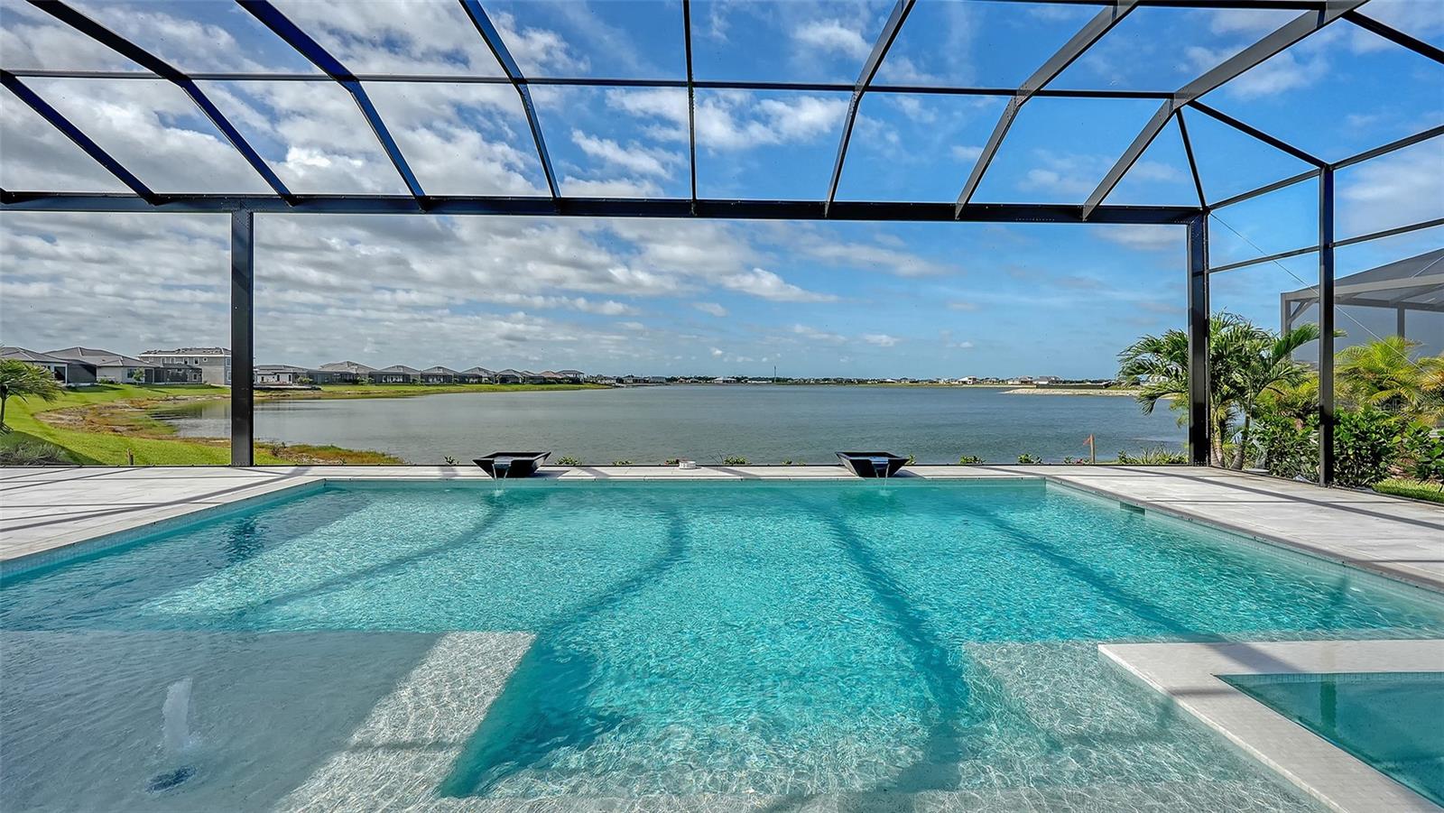 Seize this opportunity to own a brand new, never-lived-in Sterling IV in one of Lakewood Ranch's most sought-after communities, Wild Blue, available now, and without the wait! Set on an oversized homesite with sweeping lake views & southern exposure over your pool & spa, this 2026-built home delivers over 3,700 sq ft of luxury where no upgrade was left behind.
Arrive to impressive curb appeal: manicured landscaping frames a paver driveway leading to a modern entry with iron & glass impact doors, greeting you and your guests with a sweeping lake view visible from nearly every room.
The open-concept floor plan features soaring volume ceilings with dropped soffits & trayed ceilings, large format tile, 12" baseboards, designer lighting, & abundant natural light. Impact pocket sliders connect seamlessly to the resort-style lanai & lakefront beyond.
The gourmet kitchen stuns with custom cabinetry in Summit Bronze bases & island contrasted by Summit Glacial uppers. Cambria Berkshire Brass Smooth countertops wrap the oversized island with a 12" overhang & waterfall leg. IWT Vetri 24x24 Bronzo tile backsplash anchors the cooktop. Appliances include a JennAir 36" six-burner gas rangetop, 1,200 CFM Torino hood, paneled GE Monogram refrigerator & freezer columns, JennAir paneled dishwasher, & under-counter refrigerator drawers. The wet bar features a Nio black & gold faucet with instant hot dispenser.
The primary suite offers direct lake views & a spa-inspired bath with freestanding soaking tub, oversized walk-in shower, split dual-sink vanity, & private water closet. Three guest bedrooms feature walk-in closets, two with en-suite baths, and one doubling as a pool bath. A study, lakeside bonus room, beautifully finished laundry room, & mudroom complete the interior.
The covered lanai features a linear fireplace, ceiling fan, & plumbing for grill, exhaust & sink. The heated saltwater pool includes a raised spa, sun shelf, water fountains, water bowl features, & panoramic screen enclosure framing long lake views.
Wild Blue at Waterside offers walking trails, yoga lawn, putting green, dog park, playground, basketball court, dock & kayak launch, & the Midway Sports Complex with eight pickleball & six tennis courts. The waterfront clubhouse with restaurant, fitness studio, golf simulator, theater, billiards & dual resort pools is on track for fall 2026. Minutes from Waterside Place, UTC, & Lakewood Ranch Main Street, 1046 Blue Shell Loop at Wild Blue is the pinnacle of luxury living.