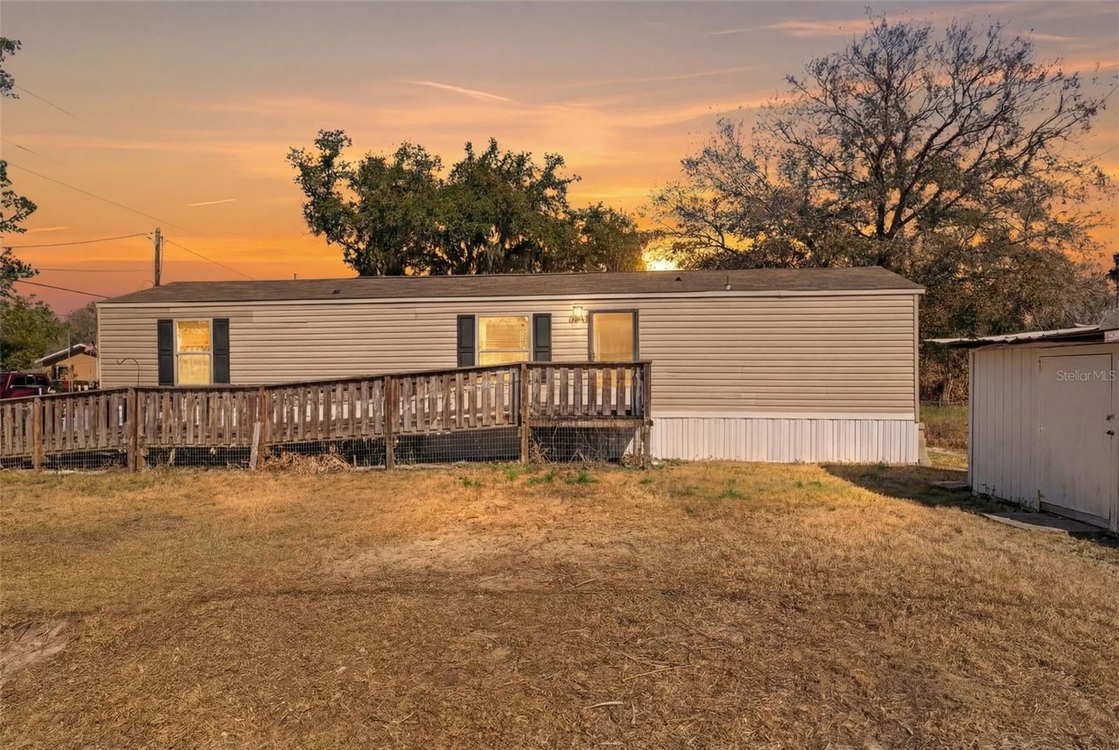 Situated on a .15-acre lot with peaceful tree-lined views, this 2-bedroom, 2-bath single-wide mobile home offers comfortable living with thoughtful updates and an inviting open layout. A wooden ramp provides easy access to the front entrance, leading you into a bright open-concept living room, kitchen, and dining area enhanced by vaulted ceilings, durable luxury vinyl flooring throughout, and a wood-burning fireplace that adds warmth and character to the main living space. The kitchen features a large breakfast bar perfect for casual dining, a stainless steel stove, and a white refrigerator, all flowing seamlessly into the main living area for effortless everyday living and entertaining. The primary bedroom includes a window for natural light and a convenient attached laundry area, while the ensuite bathroom offers a single vanity and step-in shower. The second bedroom also features a window and easy access to the second bathroom, which includes an extended single vanity for additional counter space and a shower/tub combination with grab bars. At the rear of the home, exterior stairs lead down to the backyard where you’ll find a storage shed for tools and equipment, all within a chain-link fenced yard that provides both openness and definition of space. With the roof and hot water heater approximately three years old, this property offers added peace of mind. Located in Inverness, you’ll enjoy close proximity to Fort Cooper State Park for scenic trails and lakefront recreation, the waters of Lake Henderson for boating and fishing, and the charming downtown area of Inverness with its local shops and dining, along with access to the Withlacoochee State Trail, offering miles of paved paths for biking and walking, making everyday living here feel both peaceful and connected.