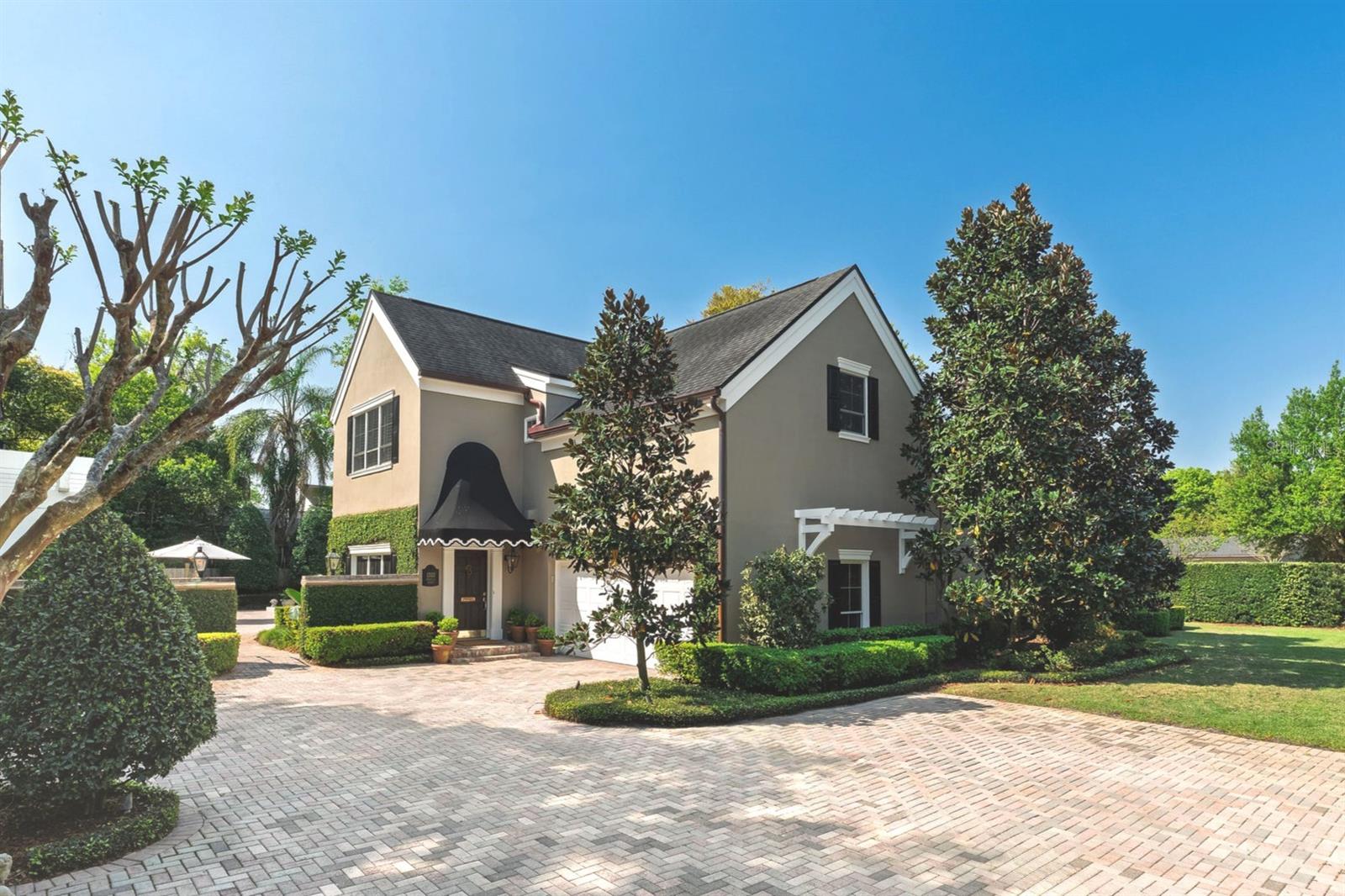 Tucked behind towering hedges on a coveted brick-lined street, this estate sits on an approximately ½-acre corner lot, providing modern functionality, Old World charm, and an unmatched lifestyle. The main residence spans over 3,600+ SF with 4 bedrooms, 4 bathrooms, and an attached 2-car garage. Across the brick driveway is a detached, fully-equipped 700+ SF studio apartment (5th bedroom suite) located above an additional 2-car garage, and an air-conditioned outdoor bar. With two dwellings, a 4-car garage, and an expansive outdoor entertaining space on a ½ acre lot, this home is a true private compound. Notable updates include newer HVAC systems (2020 & 2025), a new tankless gas water heater (2024), a fully renovated laundry room with new LG stackable washer/dryer, newer kitchen appliances, new copper gutters and downspouts, fresh exterior paint (2025), a newly designed primary bathroom, and much more... Ask for the $400K list of improvements! Enter the main residence to a family room that stretches 30 feet wide, with 12-foot ceilings, a gas fireplace, and multiple French doors lining the rear wall to showcase the brick-paver pool deck and lush, fenced-in backyard oasis, and southern exposure that invites natural light all morning and afternoon. The expansive family room is open to the kitchen, making this home ideal for entertaining. The kitchen perfectly balances charm and function, with a NEW Sub-Zero refrigerator, natural gas Wolf range, 2 Miele dishwashers, a copper-topped island that offers room for prep, serving, or seating, and a spacious dinette area with pool views. Behind the kitchen sits a dining room and adjacent den (currently used as a library/office) for more living/dining flexibility. A side entrance opens to a covered side porch overlooking a generous side yard framed by tall Podocarpus hedges... ideal for pets, a fabulous garden, or future expanded parking. A 1st floor rear bedroom wing presents 3 bedrooms & 3 full baths. Privately positioned upstairs, the expansive primary suite offers a quiet retreat, highlighted by a recent luxury bathroom renovation with elegant custom finishes including a large glass shower with 3 showerheads, 2 separate vanities, a Toto washlet, and tons of cabinetry for linen storage. French doors from both the bedroom and bath open to a covered balcony overlooking the backyard and pool, while 3 custom walk-in closets create a true dressing room experience, or the perfect opportunity to turn excess space into an office or special hobby room. Designed for entertaining, the outdoor living is equally impressive, with a sprawling lawn surrounding the large saltwater pool and an expansive paver patio for lounging and dining. A covered, air-conditioned bar is designed with custom cabinetry, exquisite lighting, a copper sink, dishwasher, wine fridge, and beverage fridge...all secured by an electronic storm shutter. The extended bar seamlessly serves the adjacent tent-covered lounge area, complete with a natural gas grill, pool bath, and outdoor shower. Above the detached 2-car garage is the studio apartment with a private entry, along with a full kitchen and bath, making it ideal for extended stays or flexible living arrangements. Located just minutes from the vibrant Park Avenue, this distinctive Winter Park compound is a one-of-a-kind property!