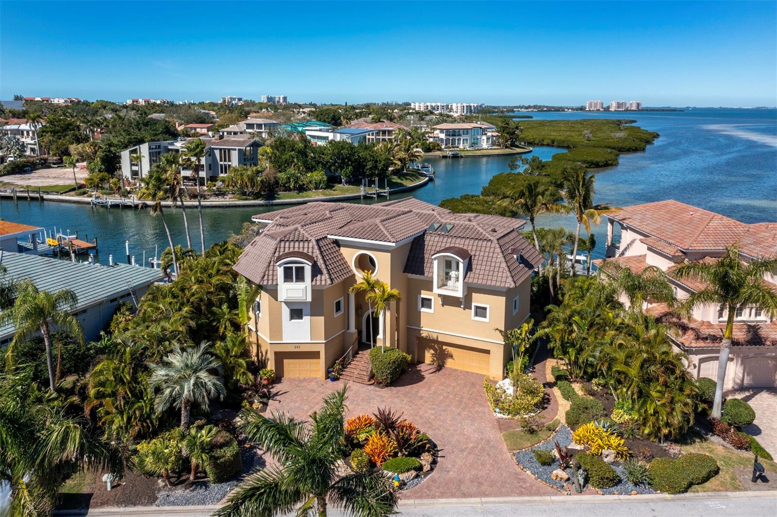 Discover a realm of unparalleled luxury as you arrive at this majestic 4BR +Office, Den, and Fitness Room/5.5BA, 5,300+/- sq. ft. property on coveted Putter Lane, a sought-after gem within the prestigious Country Club Shores on Longboat Key. The stately paver drive, adorned by lush, meticulously manicured landscaping, sets the stage for the grandeur that awaits in this 3-story haven. Elevated to capture the breathtaking surroundings, the home beckons you to follow the steps to its stately double-door entry, flanked by double garages, with tiled floors, that accommodate up to 6 cars, creating a car collector’s paradise. Upon entrance, the commitment to quality in design and style comes to life, as the architectural details, featuring sleek curves and stately columns, create an opulent ambiance that is further enhanced by walls of glass framing breathtaking views. The highlight of the residence is the soaring 2-story wall of glass that showcases one of the most spectacular views on the Suncoast, where the infinity-edge pool creates a mesmerizing backdrop where manatees and dolphins play. The floor plan is designed for entertaining, with a large circular bar seamlessly connecting the living area to the kitchen, which itself is a culinary delight, boasting stone countertops, rich wood cabinetry, two wine fridges, top-of-the-line stainless-steel appliances, and an adjacent dining area with panoramic views through walls of glass. Two primary suites, one on each floor, offer luxurious retreats with voluminous walk-in closets and spa-like bathrooms featuring dual vanities, spa tubs and separate showers. Guest accommodations are equally lavish, providing ample space and privacy. For boating enthusiasts, this direct bayfront residence is a dream come true, featuring a dock with lift, floating kayak launch, and access to the Gulf of Mexico. The expansive, elevated pool area is a tropical oasis, offering plenty of space for lounging or entertaining, all while enjoying the breathtaking water views. All the world-class boutiques and restaurants of St. Armands Circle are nearby, and the cultural attractions, shopping and dining venues of downtown Sarasota are just a short drive away.