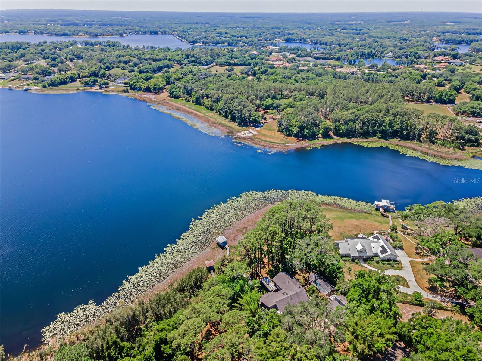 Virtually Staged. This spectacular waterfront manor is nestled on over 4.25 acres on the banks of shimmering Lake Calm. A winding driveway reveals stately wrought iron gates providing entrée to this secluded haven. An architectural masterpiece, this home has been brilliantly renovated, while the property’s design presents private access to the 113-acre lake where you may jet ski and boat to your heart’s content. Contained within this tranquil compound are pickleball/tennis courts, a resort style pool, an endless lap swim spa roofed for all-weather access, and a long pier ending in a covered dock porch with newer wood and railings. Tree-lined, pavered pathways throughout the grounds provide access between amenities; the sunsets are absolute works of art. Enjoy these magnificent twilight vistas from every angle indoors and out. Wonderfully eclectic, this 6,008 SF, 5-bedroom, 5.5 bath residence boasts the perfect blend of luxury contemporary and richly traditional stylings. From the entryway’s stunning stained glass door frame to the splendid grand foyer’s marble floors, to the formal living and dining room’s 20-foot ceilings, the gourmet kitchen shines with walnut cabinetry, quartz countertops, newer faucets, and a dining area. Hardwood bookcases adorn the main floor’s office/library offering access to the commercial grade marble-floored elevator, complete with battery backup. Located just outside this impressive space is a newer side porch. The living room’s soaring ceiling and walls of windows surround a striking fireplace. Multiple sets of glass doors lend entree to the adjacent sunroom/game room. The gorgeous family room’s electric fireplace is mounted on a travertine wall. Newer fans were mounted on the porches; the interior was recently repainted. For even more in sumptuous living, the master suite is a retreat furnished with exquisite fixtures and finishes, a standalone Japanese soaking tub, a spacious shower room, and its own balcony. The detached 3 car garage was outfitted with new door openers and the tracks replaced to maintain a watertight seal. The guest suite above is beautifully appointed and can even alternatively serve as a yoga or sculpture studio. Over 1000 SF of space, it features a bathroom and a powder room, kitchen, and a balcony with lake views. This home’s upgrades include a commercial grade elevator to the second floor, triple water filtration throughout, a newer well, upgraded electrical, two newer A/C systems, and battery backup; underground power coming into the area will eliminate overhead lines. For the best of both worlds, sweet seclusion is surrounded by the finest restaurants and retail, all in the heart of Florida’s Gulf Coast. The word here is: paradise. Also included in the sale is a separate deeded contiguous piece of land (0.13 Acre) Tax ID #U 11 27 17 001 000000 08340.0