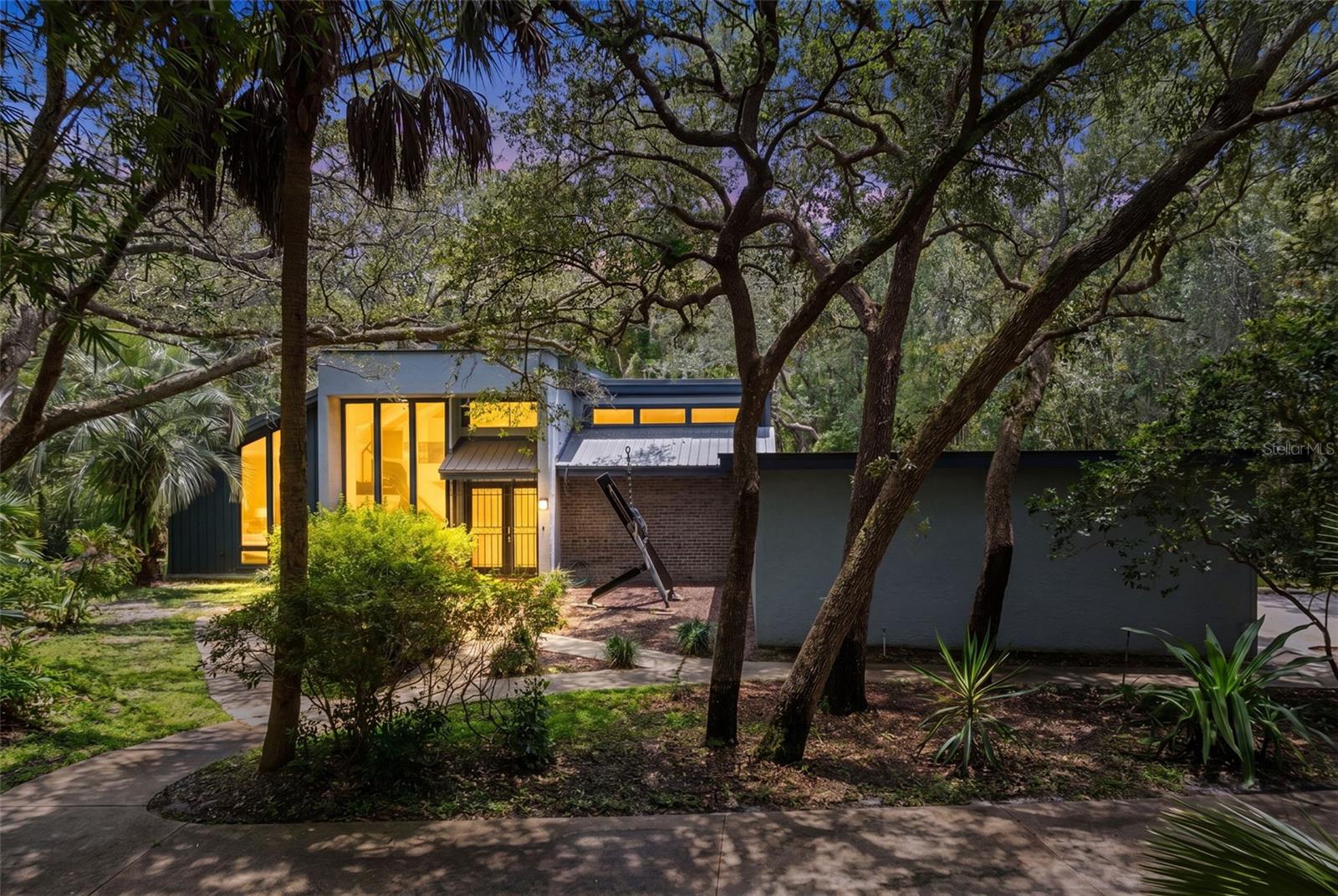 Tucked behind dual steel security gates on more than 1.6 wooded acres in sought after Tuscawilla, this one of a kind gated estate offers exceptional privacy just three blocks from the Tuscawilla Country Club and golf course. Surrounded by mature trees and natural beauty, the property feels like a private park while remaining minutes from shopping, parks, top rated Seminole County schools, major highways, dining, golf, swimming, and tennis.
This custom-built California contemporary home features 3 bedrooms, 2.5 baths, and a loft. The dramatic great room showcases soaring two story vaulted ceilings, expansive windows with tranquil wooded views, a polished granite fireplace with gas logs, built-in bookcases, and a wine rack. The adjoining dining and entertaining area includes granite countertops, a wet bar, and a built-in wine cabinet.
The kitchen is designed for both everyday living and entertaining, offering cherry cabinetry, solid surface countertops with an integrated sink, an oversized breakfast nook, and a large walk-in pantry.
An artistic steel staircase leads to the loft, an ideal space for a home office, studio, or flex room with elevated views of the surrounding landscape. The spacious primary suite features a large walk-in closet and a spa-inspired bath finished in slate with a built-in Jacuzzi tub and waterfall feature, a walk-in shower with fixed glass enclosure, bidet, and updated dual vanity.
Additional upgrades include a tankless water heater, updated HVAC system, upgraded plumbing, a large interior laundry room, oversized two car garage, and a separate workshop. The Florida friendly landscape requires minimal maintenance, and the expansive grounds provide ample room for a future pool, tennis court, guest house, or additional outdoor amenities. New septic 2025, part of roof replaced 2025.
A rare opportunity to own a private estate property in the heart of Tuscawilla with unmatched natural surroundings and modern conveniences close at hand. Zoned PUD!