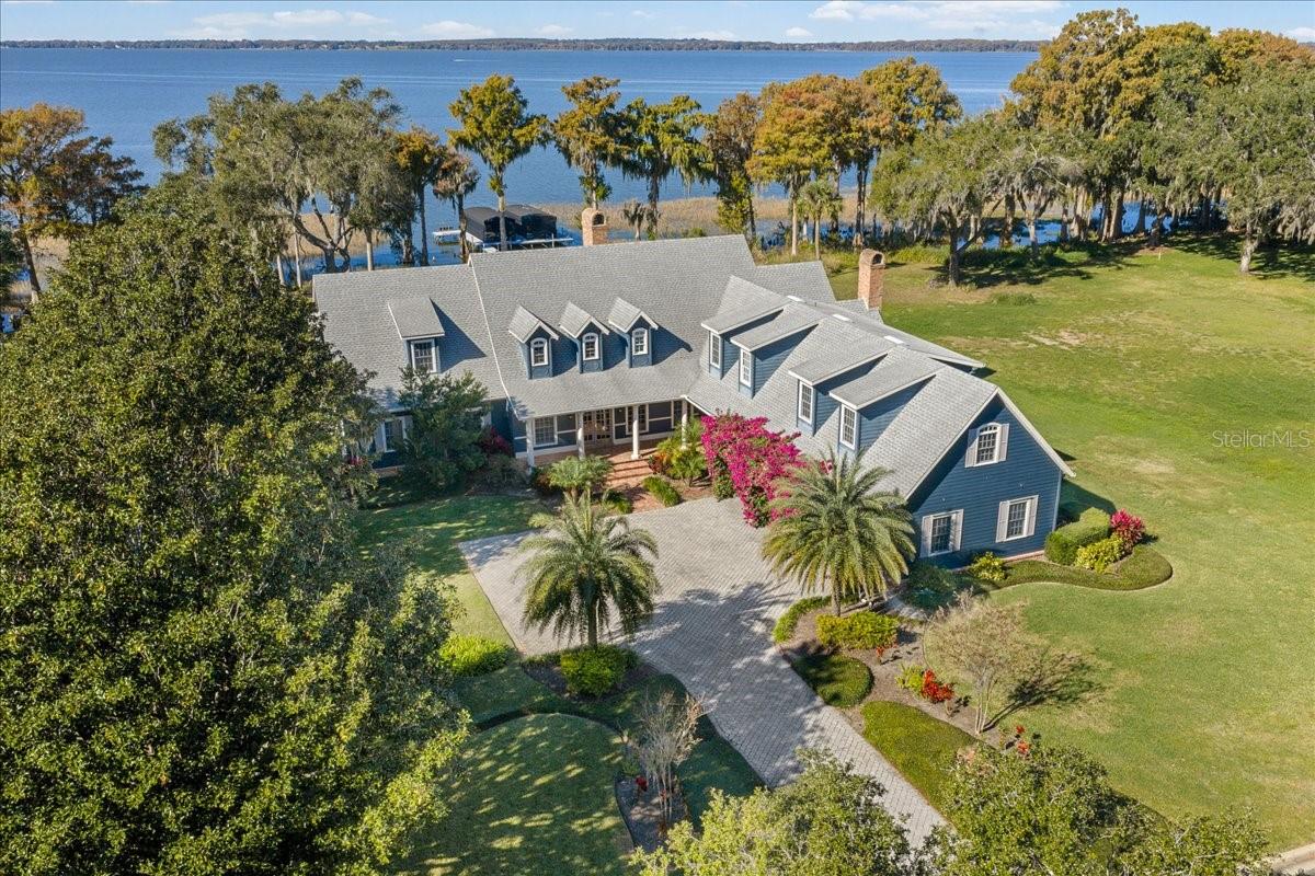 Welcome to an extraordinary lakefront estate in Tavares, gracefully positioned on a private peninsula along the coveted Harris Chain of Lakes. This exclusive enclave of 17 parcels is the most sought after address in Tavares.  Encompassing 6,288 square feet, this timeless Cape Cod-style residence, built in 1997, blends classic architectural charm with expansive living spaces and an unparalleled waterfront lifestyle.  This .9-acre home site sits at the water’s edge dotted with stately cypress trees. The sunsets are spectacular year-round and no two are alike!
Boasting 5 bedrooms, 4 full baths, and 2 half baths, this thoughtfully designed 6,288 square foot  home offers both elegance and functionality. The main level features a spacious primary suite, providing privacy and convenience, while rich wood floors and a stunning double-sided gas fireplace create warmth and sophistication throughout the living areas.
At the heart of the home, an inviting eat-in kitchen flows seamlessly into the family room, where vaulted ceilings with tongue-and-groove detailing and a cozy fireplace create an ideal gathering space.  This open-air kitchen offers a connection to the family room, kitchen dining area, and family room with vast water views of Lake Harris. Upstairs, three additional bedrooms and two full baths provide comfortable accommodations, while a separate oversized bunk room above the garage offers the perfect retreat for small guests. An additional private suite above the garage—complete with its own living room, bedroom, and full bath—adds flexibility for multi-generational living or extended stays.
Designed for effortless indoor-outdoor living, the expansive covered brick lanai is a true showpiece. Complete with a gas firepit, built-in grill station, and dedicated dining area, this space is perfect for entertaining while enjoying serene lake views and unforgettable sunsets. This covered lanai creates an abundant space for luxury dining and entertaining by the water. 
Step outside to a resort-style setting designed for both relaxation and entertaining. A free-form in-ground pool creates a private oasis, perfectly complemented by the expansive covered brick lanai.  Surrounded by lush landscaping and serene water views, this outdoor space captures the essence of Florida luxury living—ideal for hosting or unwinding poolside as the sun sets over the lake.
A lighted paver path leads to the covered boathouse featuring 2 boat slips with automated covers and electric lifts.  This is a premium, ShoreStation dock and boat lift system which enhances the waterfront experience, offering durability, convenience, and immediate access to the Chain. With direct entry to the Harris Chain of Lakes, enjoy world-class boating, fishing, and waterfront dining right from your backyard.
Live like you are on vacation with the 15,088-acre Lake Harris as your backyard or explore the 75,000+ acres of the Harris Chain of Lakes, offering old Florida scenery, waterfront dining options, and quaint, walkable downtowns. In approximately 10 minutes by boat, you can arrive at downtown Tavares, "America's Seaplane City," or the charming historic streets of Mount Dora, celebrated for its exceptional dining, boutique shopping, and year-round festivals. A rare offering where refined design meets relaxed waterfront living—this is lakefront luxury at its finest!  Home to be sold completely furnished (inquire for more details) See you at sunset!