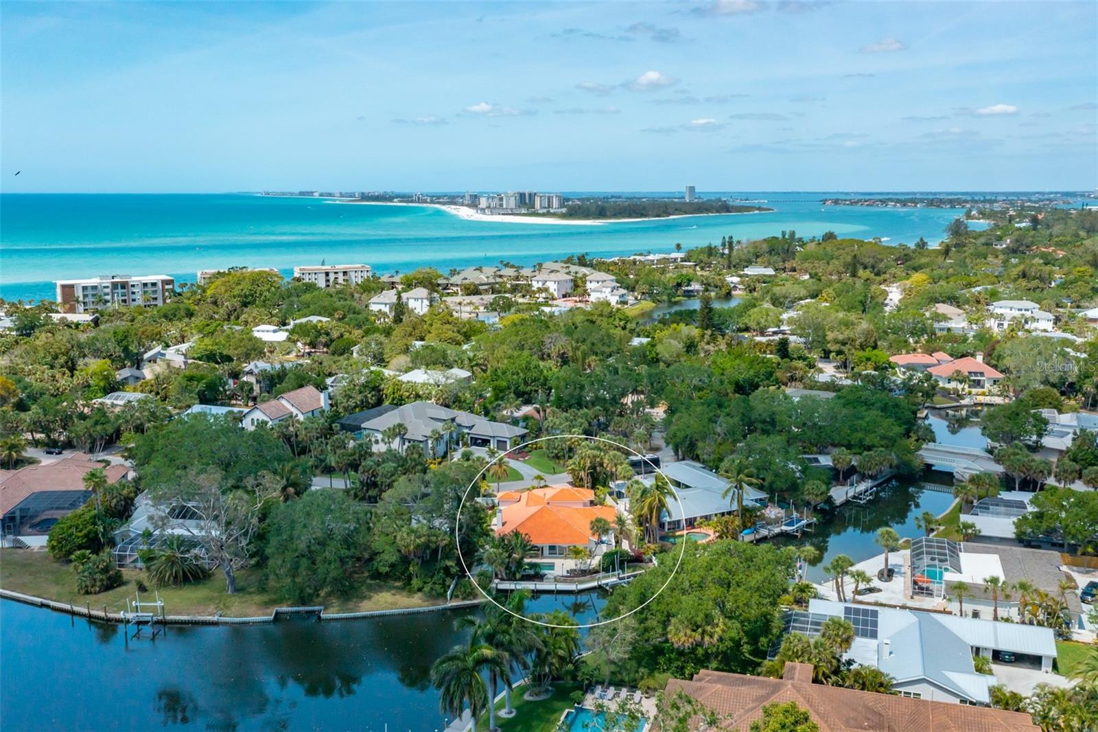 Live the dream in this delightful island home with broad water views along a T-shaped canal and
the tropical splendor of Siesta Key. Exquisite waterfront living envelops this Spanish-influenced home that lures you to enjoy even more water pleasures with a 10,000 lb. boat lift on the east that will never obstruct views. 125 ft of canal frontage creates a tranquil canvas for living. Magazine-worthy renovations means the four-bedroom, four-bath residence lives like new construction. An extensive pavered circular driveway and parking pad for the three-car garage greets your approach as you stroll through the wrought-iron gate past the pineapple fountain in the courtyard. Travertine walkways wrap around the home and lead to the large open portico and pool area. Entering through the Mexican double wooden doors into the foyer, you can see through the expansive open floor plan to the pool and beyond to the canal.  Imbued with a coastal color palette, natural light brightens the open space featuring an eye-catching cathedral ceiling and a carved stone fireplace. The sparkling white kitchen boasts Cambria quartz countertops, stainless Thermador appliances, and a beautifully designed island with seating for four. A separate living room off the main space is perfect for good conversation or family movie night under the vaulted ceiling. Engineered hardwood floors connect and unify all main areas of the home. The outdoors is a cherished feature with one or more sets of sliding glass doors in every main room. The renovated primary bedroom suite offers a large luxury bath with a door to the pool deck and walk-in pass-through closet. Step out through the bedroom’s sliding glass doors onto the portico for a late afternoon swim. The open-air portico feels like a Mediterranean getaway that houses an outdoor living room under roof and seamlessly transitions to the pool deck, pool, outdoor dining, dock, and walkway to the boat lift. Entering from the unique garage foyer, you can step into a lovely private guest suite with full bath as well as the den/office with a vaulted ceiling. Located near what has been named the No. 1 beach in the nation, this home is within walking distance of Siesta Village and its robust restaurant scene and is just over the bridge from the heart of Sarasota – known for its dynamic arts and culture scene, beautiful golf courses, and bustling waterfront downtown.