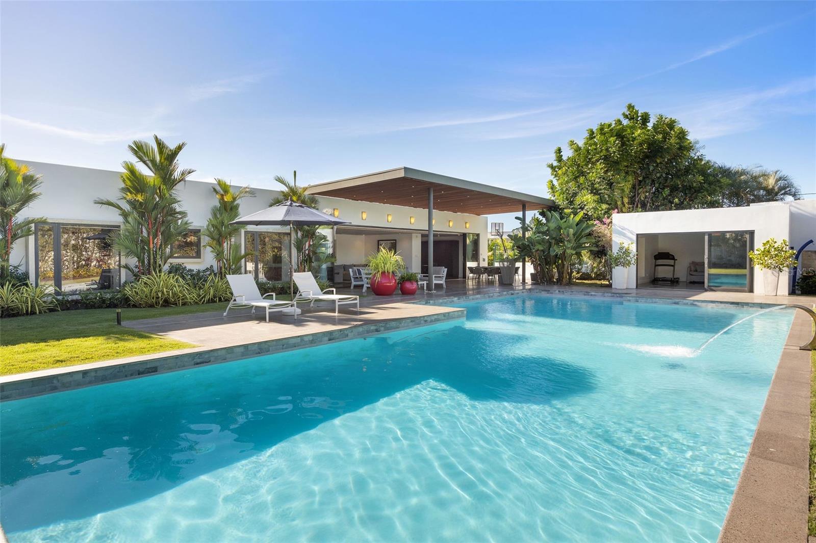 Nestled within the exclusive Santa Maria neighborhood in San Juan, this stunning one-story residence is ready for you to move in and make it your own. Boasting unparalleled privacy, this property offers a serene and peaceful living experience in one of the city's most prestigious enclaves. 
 
This exquisite home features 4 bedrooms and a total of 6.5 bathrooms, making it the perfect space for both family and guests. The basement-flex space is ideal for a man cave, playroom, or wine cellar, and the laundry and maids' room add convenience to daily life. The spacious 3-car garage even comes equipped with an electric charger for added convenience.
 
The 5660 ft.² home sits on a 2034 m² lot and is sold completely furnished, so you can move in and start enjoying your new home right away! The Leicht kitchen from Arkitectura is equipped with top-of-the-line appliances, and the full glass impact-proof windows in each room provide stunning views of the lush greenery outside.
 
As you walk out into the high-ceilinged outdoor terrace, you'll be surrounded by the magnificent landscaping, a big pool with fountain, and lots of green areas. The patio and landscape are equipped with beautiful accent lighting throughout, and a sprinkler system with timers keeps everything looking pristine. Outside, you'll find a guest quarter with a full bath that's ideal for use as an office or gym. And for basketball lovers, there's even a half-basketball court!
 
Residents of this exclusive community have access to San Francisco's Tennis Club, basketball courts, soccer, and baseball fields, providing ample opportunities for sports and recreation. The location is also very accessible, making it easy to get to and from all your favorite destinations. Don't miss out on the opportunity to own this luxurious and stunning home in Santa Maria, San Juan. Schedule your tour today and get ready to start living the life of your dreams!