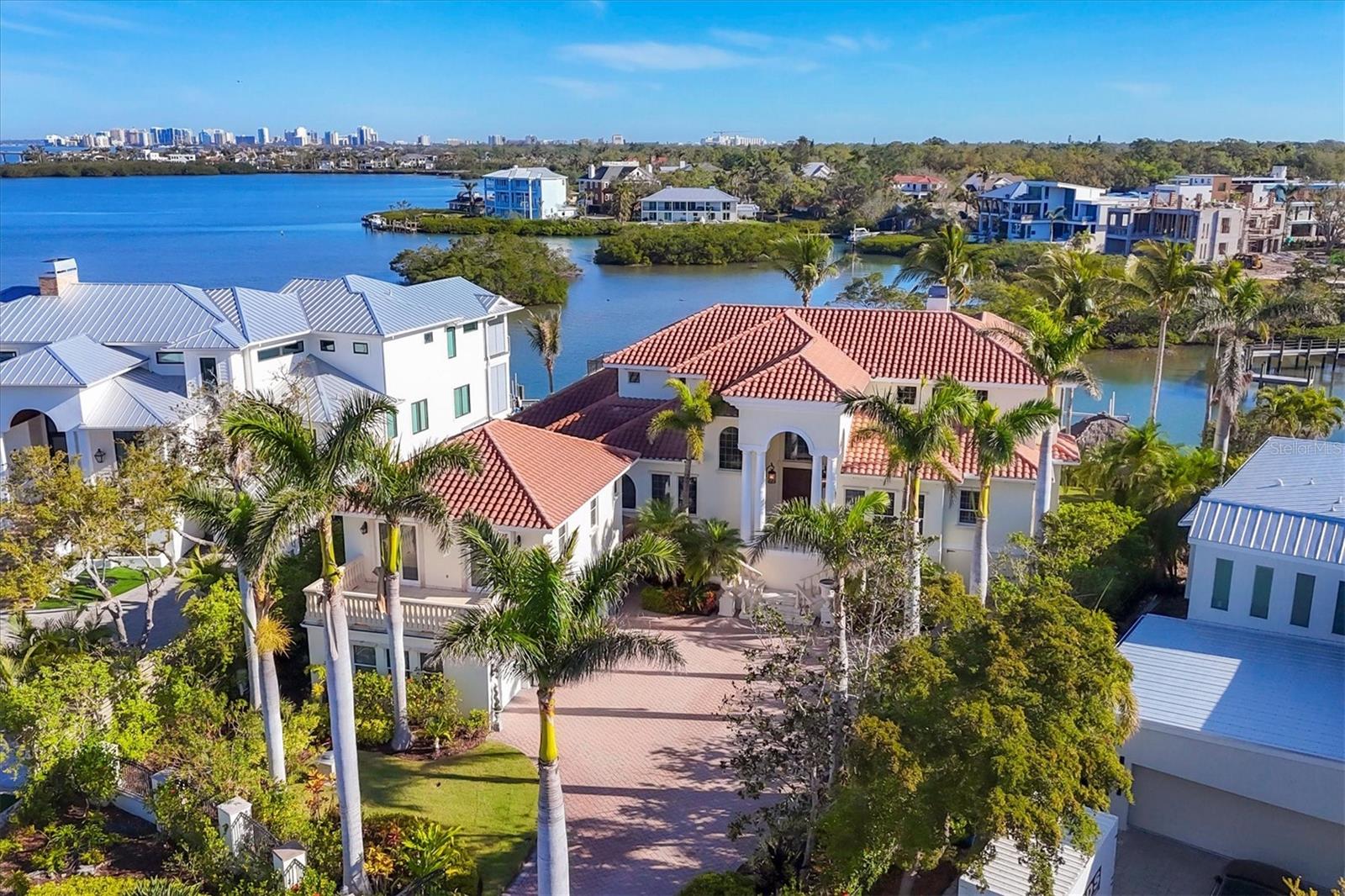 One or more photo(s) has been virtually staged. Panoramic Sarasota Bay views, a gated West of Trail setting in Oyster Bay Estates and an exceptional boating lifestyle define this remarkable waterfront residence overlooking the downtown Sarasota skyline and open waters. Blending timeless architectural details with expansive entertaining spaces and resort-inspired living, the home presents a rare opportunity to experience one of Sarasota’s most sought-after waterfront addresses. Brand-new impact-rated windows and doors are scheduled for installation in August/September 2026, further enhancing the property’s long-term value and storm readiness. A grand arrival sets the tone with travertine stairs leading to stately double entry doors framed by an arched transom window. Inside, expansive living and dining spaces are highlighted by intricate coffered ceilings, artisanal millwork, wainscoting-lined hallways and walls of sliding glass doors designed to maximize natural light while showcasing breathtaking water views. A carved stone gas fireplace anchors the main living area, while seamless indoor-outdoor flow enhances the home’s elevated waterfront atmosphere. Designed for both entertaining and everyday living, the chef’s kitchen features an oversized center island with prep sink, granite countertops, custom wood cabinetry and premium Viking® appliances paired with a Sub-Zero® professional refrigerator. A walk-in pantry with custom organization and an adjoining butler’s pantry with beverage cooler, dishwasher drawers and glass-front cabinetry create exceptional functionality for hosting. Breakfast and casual dining spaces are positioned to capture spectacular waterfront and skyline views from nearly every angle. The great room is surrounded by windows framing Sarasota Bay, lush tropical scenery and the downtown Sarasota skyline, while multiple entertaining bars with beverage coolers, prep sinks, dishwasher drawers and granite countertops provide ideal gathering spaces for family and guests. The primary suite serves as a luxurious private retreat featuring windows overlooking the water, a custom sitting area and a spa-inspired bath with travertine finishes, dual vanities, jetted soaking tub, oversized walk-in shower and custom-designed walk-in closet. A dramatic wood staircase leads to four additional en-suite guest bedrooms, each with access to an enormous balcony showcasing stunning downtown and water views. A three-stop elevator provides convenient access throughout all levels of the residence. The ground-level bonus area seamlessly connects to the resort-style pool deck, creating exceptional flexibility for indoor-outdoor waterfront living. Above the garage, a private guest apartment with separate staircase access offers a living area, kitchenette, spacious bedroom, full bath and private balcony, ideal for extended guests or multigenerational living. Additional highlights include hardwood flooring, plantation shutters, crown molding, custom tray and coffered ceilings, a central vacuum system and extensive architectural detailing throughout. Located minutes from Siesta Key, Southside Village and vibrant downtown Sarasota, this extraordinary Sarasota waterfront estate offers a rare combination of luxury bayfront living, boating access, panoramic sunset views and timeless coastal elegance in one of Sarasota’s premier West of Trail neighborhoods.