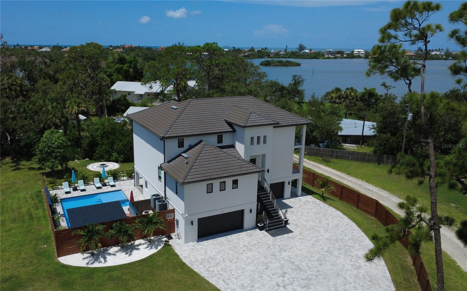 Completed in 2022 and builder/owner-occupied since, this exceptional contemporary home delivers modern Florida living with no HOA restrictions. Designed and built by OMKAL Construction, it reflects the craftsmanship and thoughtful engineering found in the area’s finest new coastal homes. Built to the newest Florida Building Code with impact-rated systems, an elevated stem-wall foundation, and energy-efficient construction, it provides lower insurance costs and greater peace of mind compared to older waterfront properties.
The three-story layout features elevated main-floor living with abundant natural light, enhanced privacy, and upper-level balconies capturing coastal breezes and sunset views. The ground level opens directly to the pool for a private resort-style setting.
Spanning approx. 3,300 sq ft under air and 6,000 sq ft total, the home lives larger with open-concept interior, expansive balconies and lanai, oversized garages, and a fully finished lower level. Highlights include a dramatic two-story great room with massive picture windows and a custom linear fireplace, a chef’s kitchen with sleek modern cabinetry and an oversized island, a main-floor master suite with two additional bedrooms, plus an upper-level loft and second master suite with views toward the Intracoastal Waterway. The finished lower level serves well as a media lounge, fitness area, or multi-use recreation space.
Outdoor living includes a large heated saltwater pool with spa and tanning ledge, fire pit, porcelain accent walls, tiki torches, custom fencing, covered pergola with grilling area, accent lighting, and tropical landscaping. Quality construction details include hurricane-impact windows/doors, flat tile roof, synthetic stucco, large-format porcelain tiles, and Level 5 smooth drywall.
Additional option: An adjacent water-access parcel on Oak Street (offered separately) provides no-fixed-bridge access to the Intracoastal for kayak, jet ski, or small boat usage.
Meticulously maintained and move-in ready, this home delivers the benefits of newer construction without renovation costs or deferred maintenance, minutes from Venice, Sarasota, Casey Key beaches, and the North Jetty.