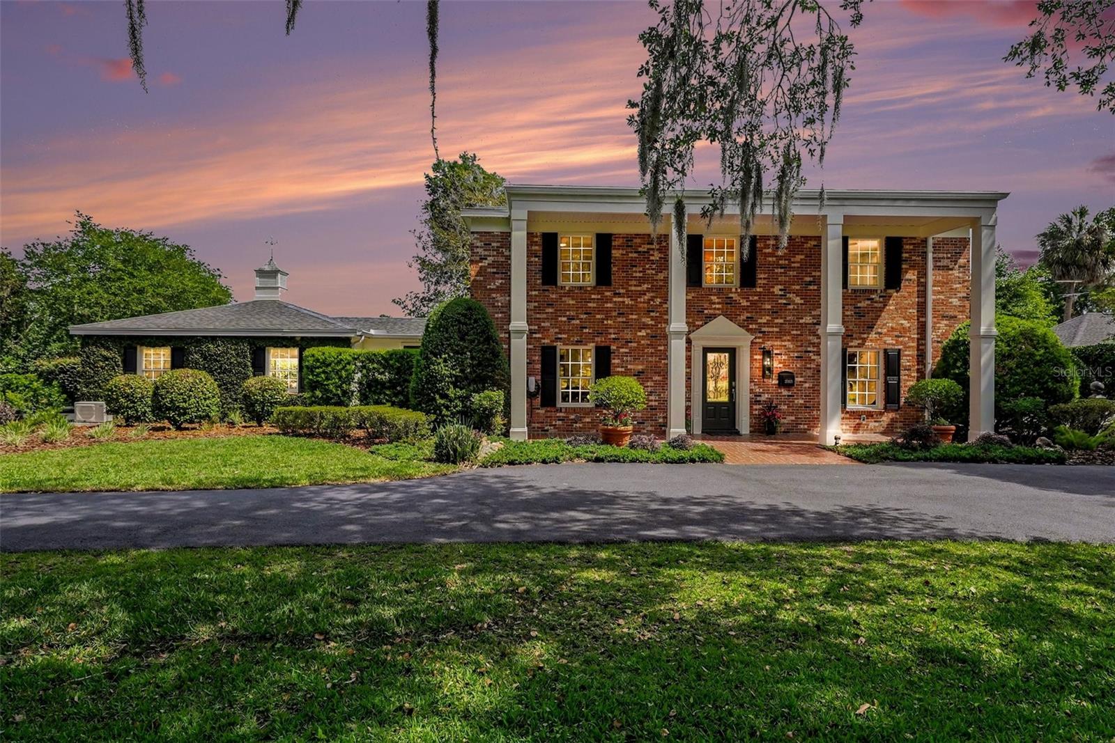 Modern Luxury meets Timeless Elegance.   Majestic Oaks grace the curved drive to soaring two-story columns framing the entrance of this completely reimagined estate.  The foyer sets the tone — bright, welcoming, and purposeful. Veer right into the handsome front office/den, ideal for working from home or quiet reflection. Then follow the natural flow left into the spacious formal dining room and thru the Butler’s Pantry. The kitchen is a showstopper. A commanding center island anchors the space, offering sit-down dining on one side and generous prep counter on the other. A new 5-burner cooktop with pot filler sits beneath a sleek Viking hood plus dual ovens with convection and microwave capability. Sixteen feet of quartz countertops run the length of the room flanked by matching stainless refrigerators. New cabinetry, designer lighting, and flawless finishes round out a kitchen that is as functional as it is stunning. Pause at the breakfast bar — the view tells the story: a crackling fireplace, a private courtyard, and the shimmering pool beyond. Then continue through to the Family Room, where oversized glass doors blur the line between indoors and out. Whether it's game night, movie night, or hosting a crowd, this space delivers. A main-floor bedroom and full bath complete the first level. Ascend the staircase where the warmth of original hardwood floors greets you at a central sitting area — a quiet retreat between the wings. The primary suite is a sanctuary unto itself: two private balconies, a spacious walk-in closet, and a spa-worthy en suite featuring a quartz dual-sink vanity with lighted mirrors, a jetted tub, and walk-in shower. Two Jack & Jill bath configurations serve bedrooms 2 & 3 and bedrooms 4 & 5, each with walk-in closets. Bedroom 5 opens onto the upstairs pool balcony — a coveted perk. Upstairs laundry adds everyday convenience. Back on the main level, step outside to a lush oasis framed by blooming magnolias, established garden beds, and two graceful fountains. With direct access from the Great Room, Family Room, and kitchen, outdoor entertaining flows effortlessly. Completely renovated in 2026 — new electrical, plumbing, fixtures, cabinets, countertops, flooring, and drywall throughout.   Every detail is reimagined. This is rare.  
Historic address. Modern soul. Timeless elegance.