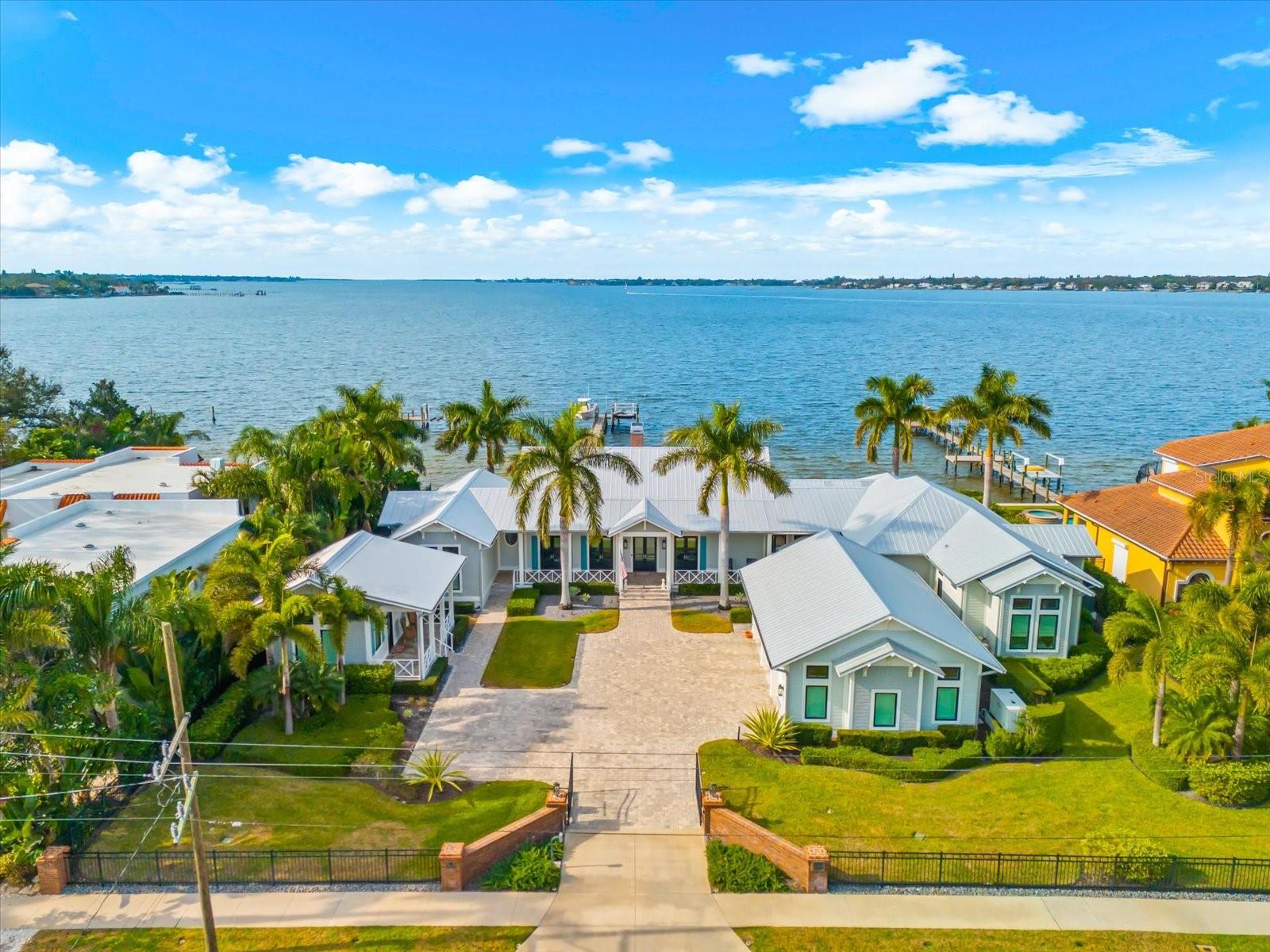 Manatee River Waterfront SHOWSTOPPER! Located in the heart of Downtown Bradenton, this custom-built coastal estate was completed in 2017 by renowned local builder Stephen Carlsen and offers breathtaking panoramic water views along 150 feet of pristine waterfront on an expansive 21,750 sq. ft. double lot. Positioned 8ft. in elevation the property did not flood or take on water during Hurricane Helene in 2024 and includes an assumable flood insurance policy of only $1,394 annually. This 4-bedroom, 4.5-bath coastal masterpiece provides 4,252 sq. ft. of air-conditioned living space and 7,153 sq. ft. total, thoughtfully designed with a timeless Key West–inspired aesthetic. A bonus “Casita” guest house with its own private entrance includes a bedroom, bathroom, and walk-in closet, offering a luxurious and private retreat ideal for guests or extended stays. The home showcases volume ceilings, extensive custom trim detailing, and wide-plank engineered hardwood flooring throughout. Expansive covered patios and porches create an effortless indoor-outdoor living experience while embracing tranquil waterfront views. The home is constructed of concrete block and topped with a striking 5V Galvalume metal roof, blending durability with architectural character. Throughout the residence, Italian Calacatta Gold marble countertops elevate the kitchen and all bathrooms. The chef’s kitchen is outfitted with premium Sub-Zero refrigeration and a full Wolf appliance suite, including one electric oven, two gas ovens, and an integrated warming drawer, making it ideal for entertaining and everyday living. A Generac natural-gas whole-house generator, energy-efficient tankless water heaters, and dual-zone air conditioning in the main residence ensure comfort and peace of mind, while separate mini-split systems independently serve the air-conditioned three-car garage and guest house.

Additional highlights include Marvin Modern hurricane-impact casement windows and doors throughout, all featuring retractable screens, along with motorized retractable screens on the rear porches to seamlessly blend indoor and outdoor living. A private, secured front gate with coded entry enhances privacy, while a comprehensive monitored security system includes cameras and sensors on doors and windows. The home is also equipped with a whole-house water softening system and a private freshwater irrigation well to maintain lush tropical landscaping.
For boating enthusiasts, the property features an impressive 180-foot private dock complete with a 12,500-pound boat lift  and a dedicated dual jet ski lift, offering immediate access to the Manatee River. This extraordinary waterfront estate presents a rare opportunity to own a meticulously designed residence that combines luxury, security, and resort-style boating amenities in one of downtown Bradenton’s most desirable locations. Whether entertaining guests, embarking on a sunset cruise, or relaxing while soaking in serene water views, this exceptional property delivers the ultimate coastal lifestyle.